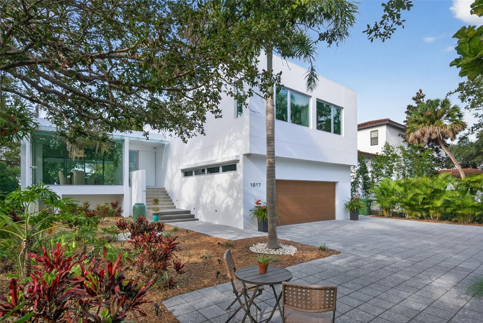 Set within a canopy-covered bayfront neighborhood rapidly emerging as THE place to live, this exceptional modern residence offers a rare blend of architectural distinction and tranquil coastal living. Surrounded by luxury homes along the bay, the property feels delightfully elevated among the trees, with partial bay views unfolding from the rear of the home.
Located just north of Downtown Sarasota, this striking 2015 modern design was masterfully conceived by noted architect Dale Parks, AIA. The home showcases refined contemporary architecture with expansive glass framed in concrete, creating a dramatic yet warm aesthetic throughout.
The open floor plan is anchored by a stunning Great Room with fireplace and a floating glass-wrapped dining area, all bathed in natural light. The chef’s kitchen features stone countertops, a glass-cut tile backsplash, distinctive Zebrawood accents, a Bosch coffee center, high-end stainless appliances, and an oversized eat-in center island ideal for both everyday living and entertaining.
Seamless indoor-outdoor living continues onto a spacious terrace complete with a summer kitchen and TV mount—perfect for hosting gatherings. Polished concrete floors add a sleek, modern touch throughout the main living spaces.
The private primary suite wing offers a peaceful retreat with generous closet space and a spa-inspired bath featuring dual vanities, a soaking tub, and private water closet. Floor-to-ceiling windows and sliding glass doors throughout the home invite abundant natural light and enhance the connection to the surrounding landscape.
A separate stairway leads to two guest bedrooms and a loft-style office, providing privacy and flexibility for guests or work-from-home living. At pool level, expansive covered and open lounging areas surround the large pool, creating a true resort-style setting. Additional highlights include an oversized storage room, a two-car garage, lush landscaping, and exceptional outdoor living spaces.