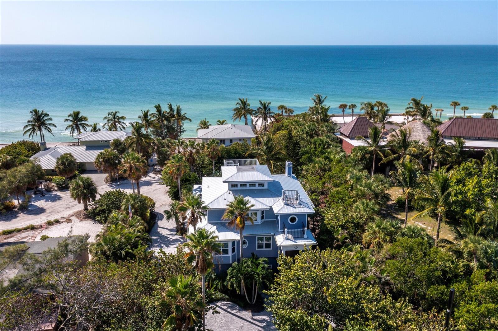 Coastal-inspired elevated pool home. This North Longboat Key 4 bedroom, 4 bath, 4,132sf  home, features beautiful engineered wood floors that flow throughout the open floorplan. The main level is ideal for family gatherings and entertaining with ample seating in the kitchen, living room, dining area and wet bar. All bedrooms have ensuite baths. The Gulf of Mexico facing glass sliders open to an expansive balcony with a gas grill overlooking the pool, spa and lush array of mature tropical trees and landscaping. Enjoy views of the Gulf of Mexico and sunsets from wide covered decks and the third-level widow's walk. Updated with Whirlpool white appliances, custom wood cabinets, quartz counters, built-in desk, wet bar, and a large island and pantry, the property also offers lots of space for parking and storage, including a three-car garage with space for paddleboards, kayaks, and recreational equipment. Other notable highlights include an outdoor shower with a dressing room, Sonos sound system throughout the property, and laundry on all three floors as well as deeded beach access across the cul-de-sac.