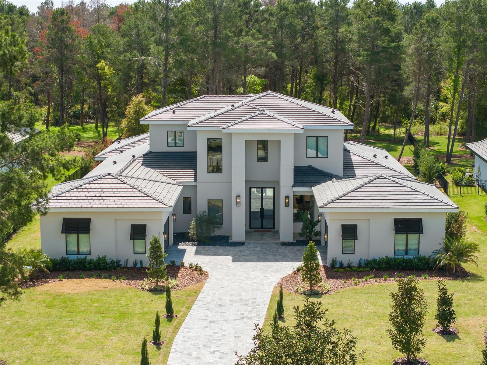 Experience the epitome of luxury living at its finest in the exclusive guard-gated country club community appropriately named Bella Collina, one of Central Florida's most sought-after residential neighborhoods. Nestled on a 1-acre estate preserve lot, this contemporary-crafted Lemans floor plan by Davila Homes boasts an impressive 5,114 square feet of living area and a total of 7,710 square feet under roof.
As you step through the double doors, the open foyer welcomes you, with a well-appointed office on the right. The gourmet kitchen is a chef's dream, featuring top-of-the-line Fisher & Paykel appliances, an 8-burner gas stove, an oversized island, and a custom-built wine wall. Adjacent to the kitchen, you'll find a half bath and a game room with pocket corner sliding doors that offer stunning views of the covered porch and lanai, complete with a custom-built summer kitchen and remote-control screens. A guest suite with a full bathroom provides comfort and privacy for your visitors.
The oversized laundry room features an elevated washer & dryer and an oversized back pantry, making household chores a breeze. The great room exudes tranquility with its natural earth tones and a soothing gas fireplace, while a wall of glass sliders leads to the covered lanai and a resort-like solar pool and spa.
The generous primary suite offers ample space for a sitting area and a spa-like primary bathroom with dual sinks, a soaking tub, and an oversized walk-in shower that leads to a customized walk-in closet. A glass stairway takes you to the second floor, where you'll find a spacious media loft, three generous en-suite bedrooms, and a covered balcony with retractable screens.
This sophisticated home is equipped with state-of-the-art features, including a Crestron electronics system, electronic drapes and shades, a built-in ground-level trampoline, pre-plumbing for a fire pit, and oversized fenced backyard with extensive landscape lighting. As the owners never moved in, you can enjoy all the upgrades without the wait of building from scratch! Enjoy all of the amenities Bella Collina has to offer including two restaurants with outdoor patios, 5-star spa, championship golf course, 5 tennis courts, basketball court, 3 pickle ball courts, fitness center with complimentary fitness classes for residents, a pool complex with bar and cabanas and year-round culinary and social events.