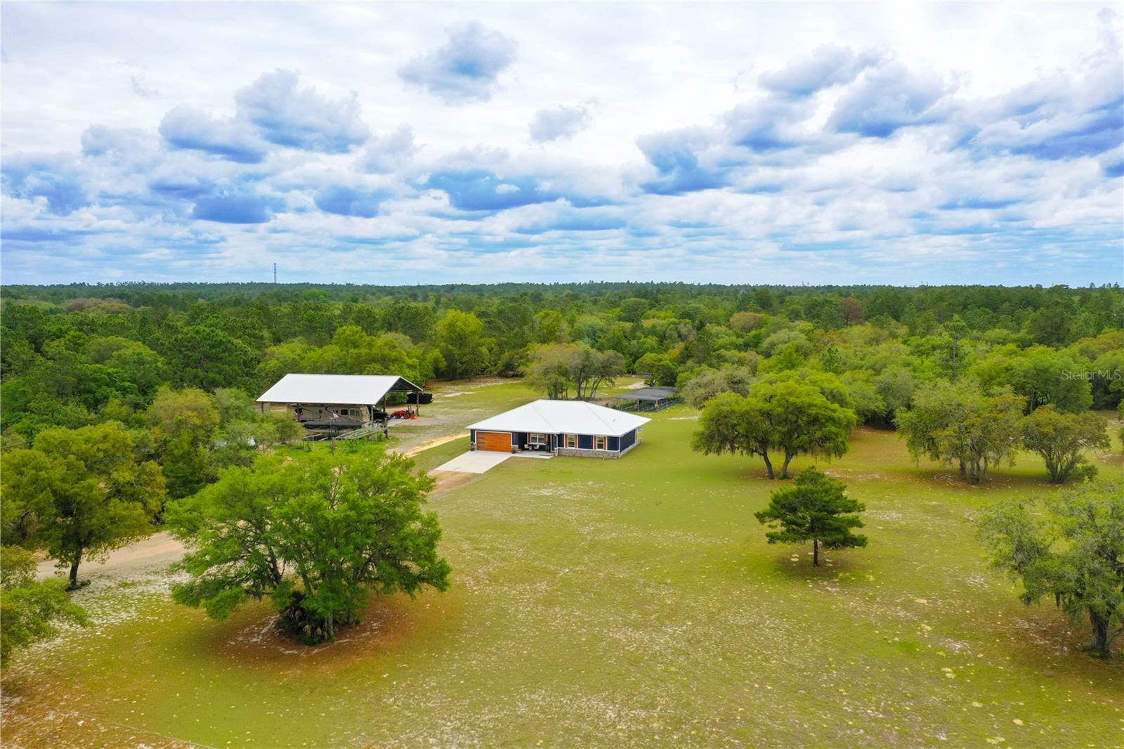 Luxury Homestead on 7.77 Fenced Acres — Custom Home with 3,600-SF Barn, Workshop, RV Storage & Equestrian Potential.

Welcome to a distinguished luxury homestead set on 7.77 fully fenced acres where privacy, refined living, and peaceful country surroundings come together. This exceptional estate offers sweeping pastoral views and an authentic garden-to-table lifestyle, complete with established gardens and fruit-bearing trees just steps from your door.

This brand-new custom home offers 2,751 square feet under roof with an open-concept split floor plan, 4 bedrooms, 2 bathrooms, soaring 10-foot ceilings, and a standing-seam metal roof with gutters. Large-format 24” x 48” porcelain tile flows throughout the home, creating a clean, elevated, and cohesive design. The versatile 4th bedroom, insulated with Safe’n’Sound acoustic insulation, is ideal as a home office, studio, media room, or guest space.

The main living area is designed to impress, featuring tray ceilings, ambient mood lighting, and a dramatic 150-inch custom media wall with a 60-inch linear fireplace and 75-inch television centerpiece. The chef’s kitchen showcases a full Forno espresso appliance suite, ceiling-height cabinetry, under-cabinet lighting, and stunning White Santorini Quartzite that flows from the oversized 117” x 48” island across the full backsplash.

The primary suite offers a private retreat with a custom walk-in closet and a spa-inspired wet-room bath featuring dual rain showerheads, a curbless shower, 65-inch stone resin freestanding soaking tub, his-and-her floating vanities, and a smart toilet bidet. Two additional bedrooms and a beautifully appointed second bath with a curbless walk-in shower and smart toilet bidet complete the interior.

Outdoor living and functionality are just as impressive. Enjoy a covered front porch, covered lanai, 2-car garage with insulated door, 400-amp electrical service, well and septic, no HOA, and Flood Zone X. The 60’ x 60’ engineered pole barn offers 20-foot peak clearance and 3,600 square feet of concrete flooring, with electric outlets at each pole, multiple water spigots, and a 50-amp RV hook-up. This incredible structure is ideal for RVs, boats, tractors, trailers, equipment, agricultural use, or additional garage space, and can be easily configured for horse stalls, a tack room, hobby space, small-business use, or the ultimate man cave.

Additional improvements include a 12’ x 18’ insulated studio shed with A/C, a 20’ x 30’ workshop with electric and concrete floors, and a chicken coop with predator-proof run. The established flock conveys, making this property ready for those seeking a true homestead lifestyle.

Bring your animals, horses, hobbies, equipment, and sense of adventure. Direct trail access for ATVs and horseback riding awaits just beyond the fence line, while the World Equestrian Center in Ocala is approximately 27 miles away. Enjoy the privacy of rural living with convenient access to Rainbow Springs, Crystal River, Kings Bay, Tampa, Orlando, Gainesville, and Ocala.

A property this complete, private, and thoughtfully improved is truly one of a kind.