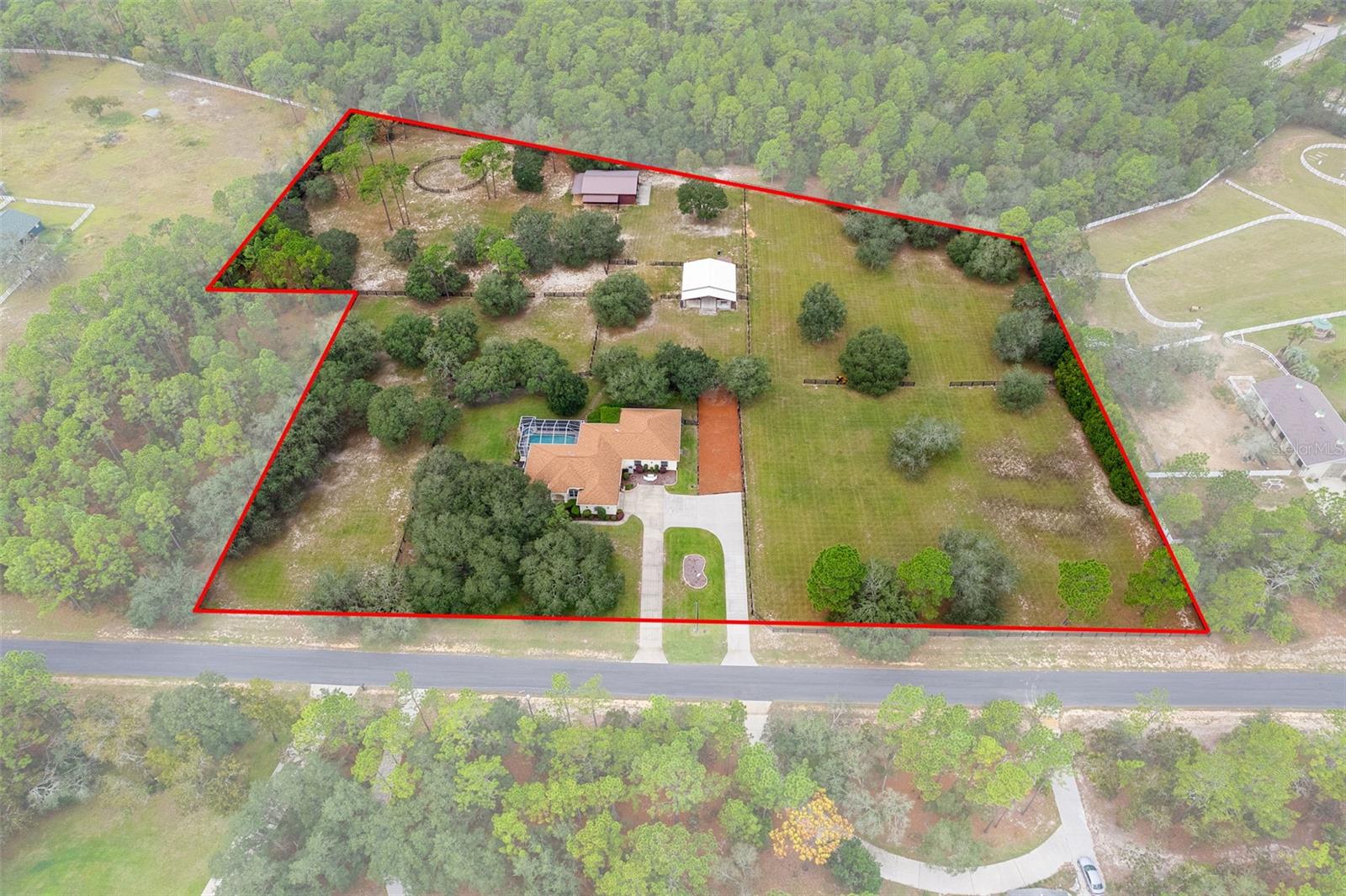 CUSTOM EQUESTRIAN ESTATE ON 7.39 ACRES OF IMPROVED PASTURE - Experience the perfect blend of LUXURY LIVING & EQUESTRIAN FUNCTIONALITY in this CUSTOM 5-BEDROOM (PLUS OFFICE), 3.5-BATH ESTATE designed for comfort, versatility, and connection to the land. With 2 PRIMARY SUITES, this home is ideal for MULTI-GENERATIONAL LIVING or accommodating a TRAINER OR STABLE HAND — the secondary suite features a PRIVATE SIDE ENTRANCE that opens into the main living area with convenient access to the HORSE BARN. Step inside and you’ll find ornate craftmanship and custom finishes throughout — from WOOD-BEAMED CEILINGS in the formal living and dining rooms to the WOOD-LOOK TILE FLOORS that add warmth and elegance. HIGH CEILINGS & ABUNDANT NATURAL LIGHT create an expansive, open, and airy feel throughout the home. The real living areas overloook the SCREENED-IN POOL AND SPA, providing year-round enjoyment and a seamless indoor-outdoor flow. Beyond the pool, the property transitions beautifully into FENCED, IRRIGATED PADDOCKS leading to a 4-STALL CENTER-AISLE BARN equipped with everything a discerning horse owner needs including MULTIPLE WASH RACKS WITH HOT WATER, FEED ROOM & SEPARATE TACK ROOM, ADDITIONAL EQUIPMENT STORAGE, SLIDING CROSS-BUCK STALL DOORS AND FEED DOORS, & BARN DOORS OPENING DIRECTLY TO PADDOCKS for easy turnout. The 7 GRASS PASTURES are irrigated by a private well, making maintenance effortless. For additional training, there’s a ROUND PEN, and behind the barn sits a 2,000 sq. ft. RV AND EQUIPMENT BARN with CONCRETE SLAB & ELECTRIC including 30 AMP & 50 AMP SERVICE. Backing directly to the 28-MILE PRIVATE HORSE TRAIL SYSTEM, this property offers quick trail access to the COMMUNITY EQUESTRIAN TRAINING CENTER featuring a large lighted RIDING ARENA, DRESSAGE ARENA, HUNT COURSE, & TRAIL COURSE. For those who compete or train regularly, it’s a dream setup — and just a short drive from OCALA’S WORLD EQUESTRIAN CENTER and FLORIDA HORSE PARK. Need more land? An ADDITIONAL 6.5-ACRE PARCEL is also available directly behind this property for expanded possibilities. This is a RARE OPPORTUNITY TO OWN A TRUE EQUESTRIAN LIFESTYLE ESTATE where LUXURY, LAND, & LOCATION unite perfectly. Don’t wait too long on this EXCEPTIONAL VALUE — properties offering this level of quality and equestrian infrastructure are few and far between.
