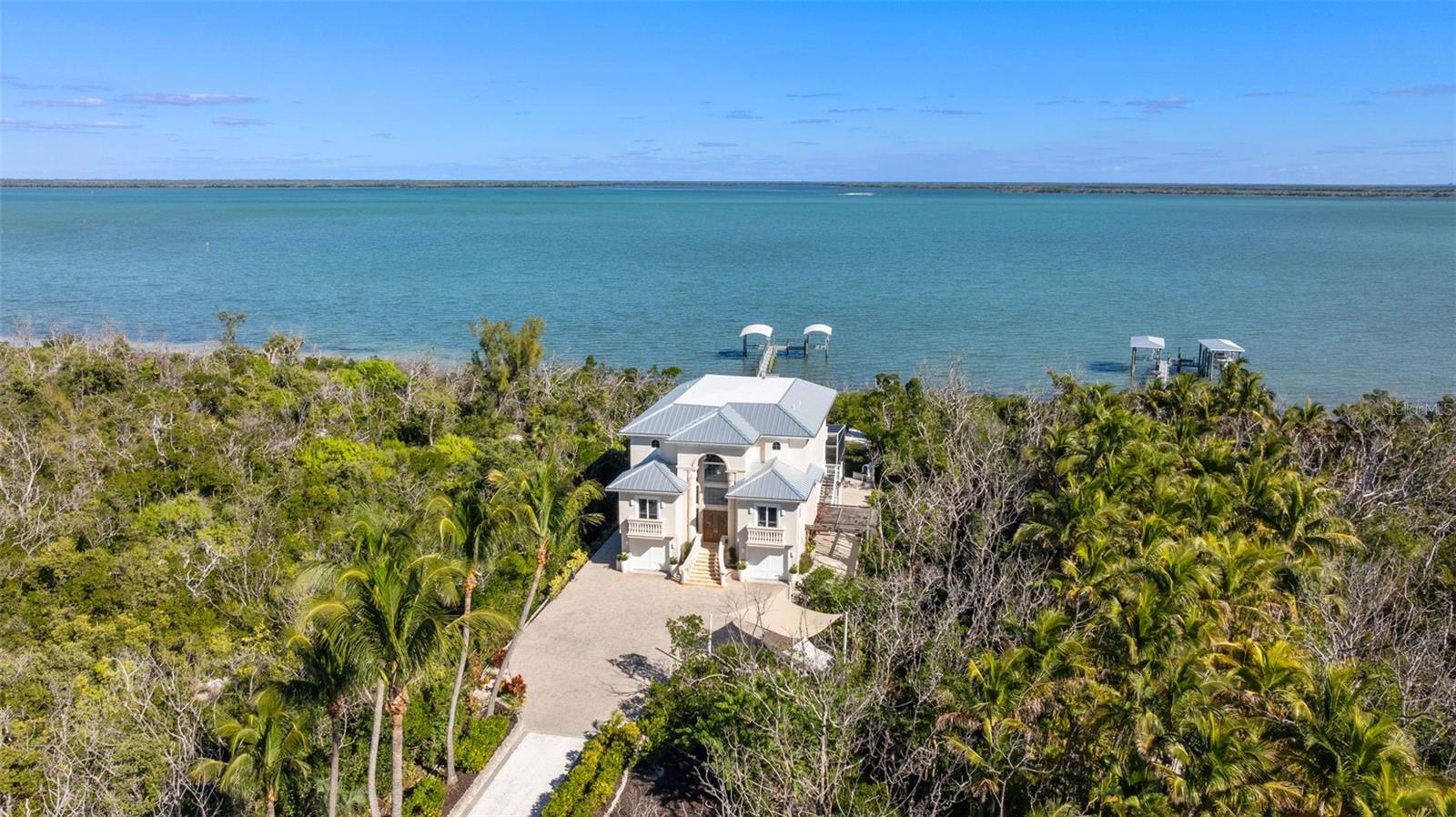 Welcome to 4150 Snail Island Court, a truly one-of-a-kind gated waterfront estate set on 3.57 acres of pristine land and bordered by a protected nature conservatory, offering unmatched privacy and natural beauty. A dramatic, palm-lined driveway with custom lighting creates a grand entrance to this exceptional residence. Built to last, the home is elevated approximately ten steps to the entry and constructed with solid block and concrete, impact-rated windows and doors, and a metal roof. Inside, the home showcases custom solid-wood doors with elegant arched detailing, and a private ELEVATOR servicing all levels for convenience and ease. The main floor is designed for comfortable entertaining and guest accommodations, featuring three guest bedrooms, each with its own ensuite bathroom. The spacious kitchen offers quartz countertops, stainless steel appliances, a breakfast bar, and a cozy dining nook. Adjacent are the formal dining area, living room, and a den with closing doors, ideal for movie nights or flex space. Sliding doors open to a spacious balcony with room for dining, overlooking the pool and surrounding nature. The third floor is dedicated entirely to the owner’s retreat, showcasing a luxurious primary suite with a private balcony, an attached secondary living room with kitchenette, a dedicated office, and two oversized walk-in closets with built-in shelving. The primary bathroom is spacious, has imported Mirano tiles, custom marble countertops, and also features a steam room. Elevated finishes include tray ceilings and decorative wall accents. On the ground floor, a large storage room—easily convertible into a bar or lounge—opens to the outdoor living area. Enjoy a covered lanai, heated pool and spa, and a backyard fire pit, perfect for relaxing or entertaining. Waterfront amenities include a recently rebuilt dock with high-end composite decking and two covered boat lifts. Adding to the uniqueness of this estate, the front yard features a private driving range, making this property as extraordinary as it is luxurious. This rare waterfront offering blends privacy, durability, and resort-style living—an exceptional opportunity on Boca Grande