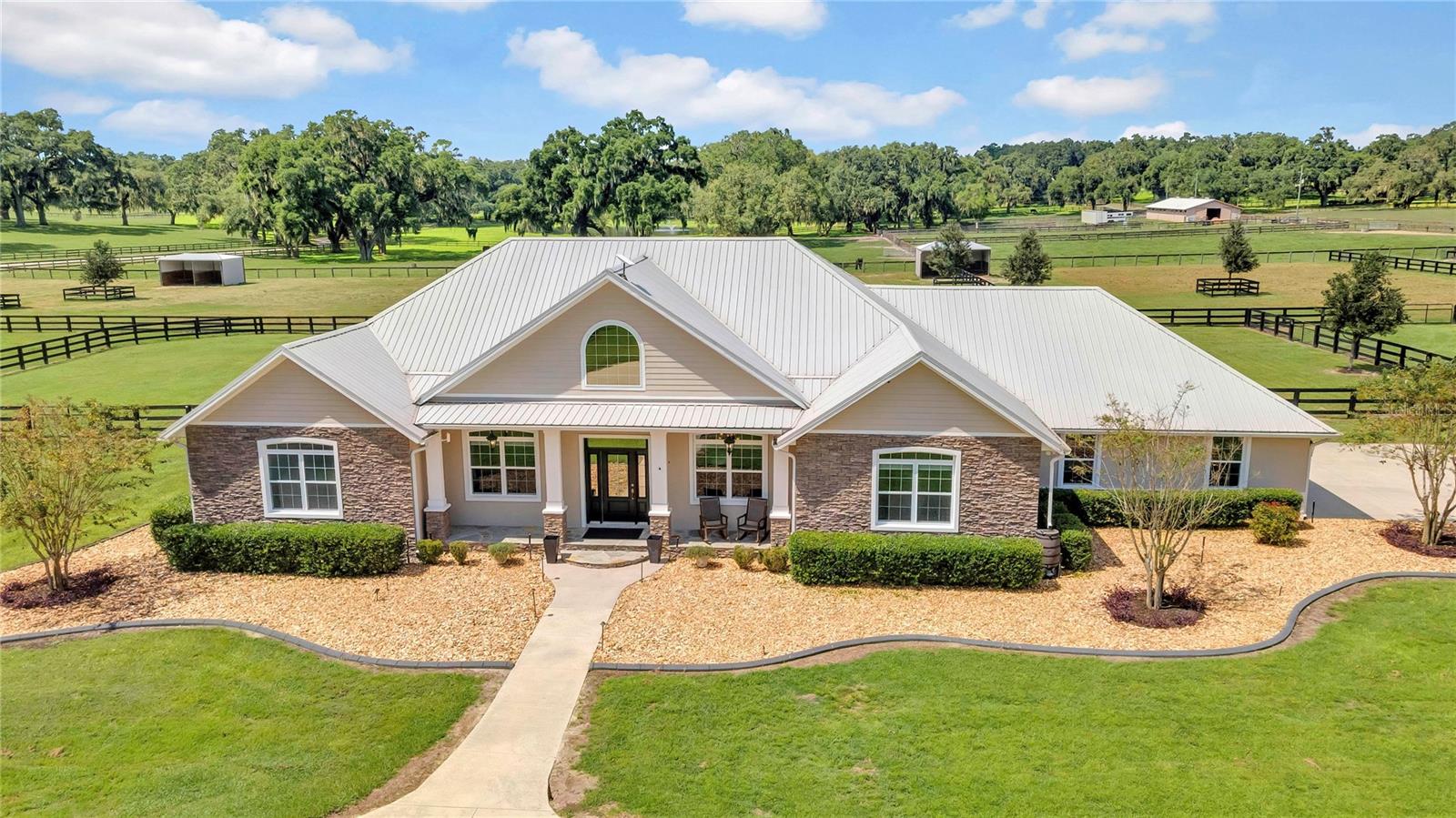 One or more photo(s) has been virtually staged. DEEDED ACCESS TO THE FLORIDA GREENWAYS & TRAILS — Ride directly to the Florida Horse Park from your own backyard! Welcome to over 10 pristine acres in the heart of Ocala’s premier horse country, where luxury living meets exceptional equestrian functionality. Located in Marion County with no HOA and no deed restrictions, this exceptional property offers the freedom and flexibility that are increasingly hard to find. Privately tucked behind a custom electric gate and winding drive, this stunning 2016 custom-built estate offers privacy, beauty, and purpose at every turn. A circular driveway and side-entry 3-car garage create an impressive arrival and provide ample space for vehicles, equipment, or recreational storage. Inside the 4-bedroom, 3.5-bath home (2,804 SF), soaring cathedral ceilings, exposed wood beams, hardwood floors, and a dramatic floor-to-ceiling stacked stone gas fireplace anchor the open split-bedroom floor plan. Expansive windows flood the home with natural light and frame sweeping views of the surrounding countryside.
The chef’s kitchen features stainless steel appliances, custom wood cabinetry, generous counter space, a center island, pantry, and breakfast nook — designed for both entertaining and everyday comfort. The primary suite is a private retreat with two large walk-in closets and a spa-inspired bath offering dual vanities, walk-in shower, and a jetted soaking tub.Outdoor living shines with a covered lanai complete with summer kitchen and built-in fire pit — perfect for gatherings after a day of riding. The heated saltwater pool and spa with waterfall and self-cleaning system (installed 2024) create a true resort-style setting overlooking the farm. Recent Equestrian Improvements: • 100’ x 200’ all-weather arena with perimeter rails and irrigation system (installed 2022) • Two run-in barns with a total of four stalls with corner feeders leading out to the pastures (constructed 2022) • Three separate paddocks/pastures (established 2023) • Three-rail no-climb fencing (installed 2023) • Wash rack with storage barn (installed 2024) With recorded deeded access to the Florida Greenways trail system, enjoy miles of scenic riding and convenient access to the Florida Horse Park — a rare and highly sought-after feature. Additional highlights include a metal roof, Generac whole-house generator, two large buried propane tanks for backup during extended power outages, Starlink internet, Ring security system, well and septic, and thoughtful upgrades throughout.
This exceptional estate offers the perfect balance of privacy, luxury design, and recently enhanced turnkey equestrian infrastructure — ideal for those who want to live, ride, and entertain in one of Ocala’s most desirable equestrian corridors.