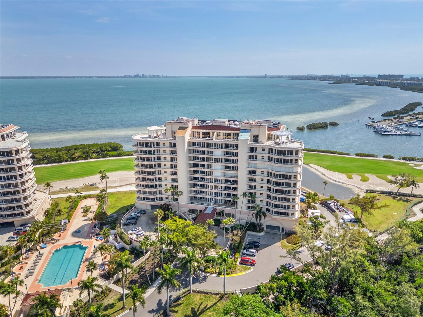 Step into the foyer from your private elevator and through chic double doors into this fully furnished Grand Bay masterpiece where drama meets elegance. Floor-to-ceiling glass sliders reveal a breathtaking panorama of the downtown city skyline, John Ringling Bridge, Harbourside golf course, and Sarasota Bay. The open floor plan seamlessly connects the living and dining areas to a versatile den—perfect as a media room or a third bedroom. Equipped with premium KitchenAid appliances, a Subzero and a central island, the kitchen includes an eating space for casual mornings. Wake up to panoramic bay views in the primary suite featuring private access to a massive wraparound terrace. The spa-like primary bath offers a garden soaking tub, dual vanities, a glass-enclosed shower and walk-in closet. The ensuite guest room ensures privacy and comfort, complete with its own stunning views of the water and greens and terrace access. Located behind the prestigious Longboat Key Club gates, residents enjoy double-gated security, Har-Tru tennis courts, a fitness center, a recently renovated Clubhouse and two heated pools. Grand Bay residents have private access to the Bay Isles Beach Club, all while being minutes away from the world-class shopping of St. Armands Circle and the cultural hub of downtown Sarasota.