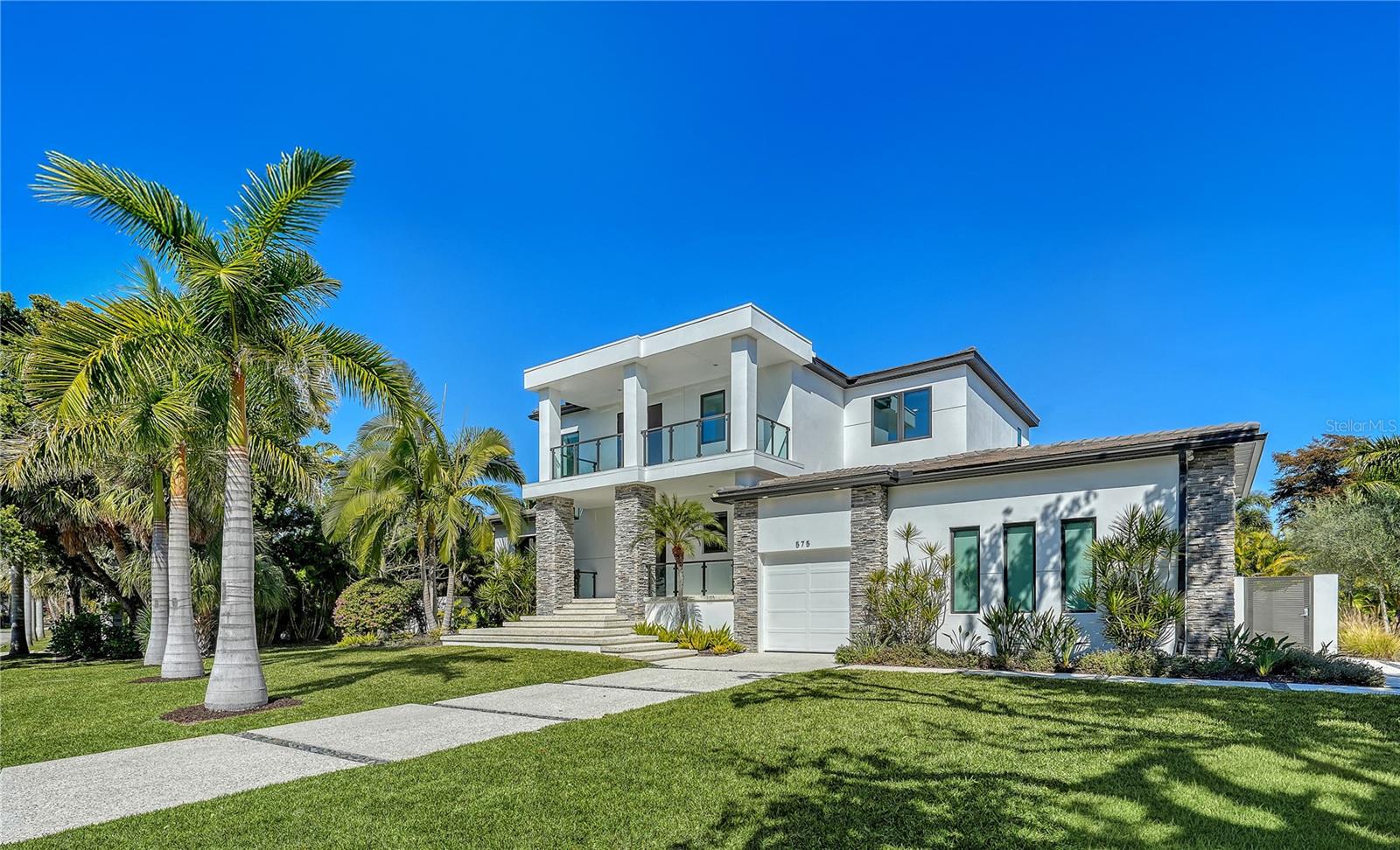 Set within the prestigious island community of Bird Key, this recently completed custom-built residence (2023) delivers refined coastal living just minutes from Sarasota Bay, St. Armands Circle, and downtown Sarasota. Spanning nearly 4,000 square feet of interior space, the thoughtfully designed two-story layout offers four en-suite bedrooms, a library/media room, den, and 5½ baths, with a shaft in place for a future elevator.

The great room serves as the heart of the contemporary home, showcasing European oak hardwood flooring throughout, soaring cathedral ceilings reaching over 21 feet, solid wood beams, and coffered architectural detail. A stone-encased fireplace anchors the space, while walls of impact-rated pocketing glass sliders open directly to the covered patio and outdoor living area, creating a seamless indoor-outdoor flow. Custom built-ins with wainscoting and illuminated display niches provide ideal space for art and decor.

The kitchen is designed for both daily living and entertaining, featuring an oversized quartz waterfall island, custom cabinetry with under-cabinet lighting, tile backsplash, walk-in pantry, pot filler, and Wolf and Sub-Zero appliances. Adjacent dining area includes a built-in buffet and direct patio access for effortless hosting.

The primary suite is located on the main level, offering pool views, extensive built-ins, and a spa-inspired bath with quartz surfaces, soaking tub, and a walk-in shower with multiple showerheads. A second en-suite bedroom on the first floor—currently used as a fitness room—adds flexibility, along with a dedicated den, laundry room, and a library/media room with custom built-ins and en-suite pool bath access.
Upstairs, a spacious loft opens to a private balcony with glass railing, currently used as office space. Two additional guest bedroom suites occupy this level, including one with a walk-in closet.

Outdoor living is complete with a fully equipped summer kitchen, covered dining area, stone accent wall, heated saltwater pool with PebbleTec finish, sun shelf, and raised spa. Additional highlights include EnergyStar insulated impact windows and doors, central vacuum, contemporary lighting, three-car garage with epoxy floors, and insulated garage doors.

Bird Key offers a premier island lifestyle with proximity to marinas, beaches, and optional membership to the Bird Key Yacht Club. Enjoy quick access to Lido Beach, Longboat Key, and Sarasota’s cultural attractions—including The Bay Park, Selby Gardens, world-class dining, and waterfront events—making this a standout opportunity in one of Sarasota’s most sought-after neighborhoods.
