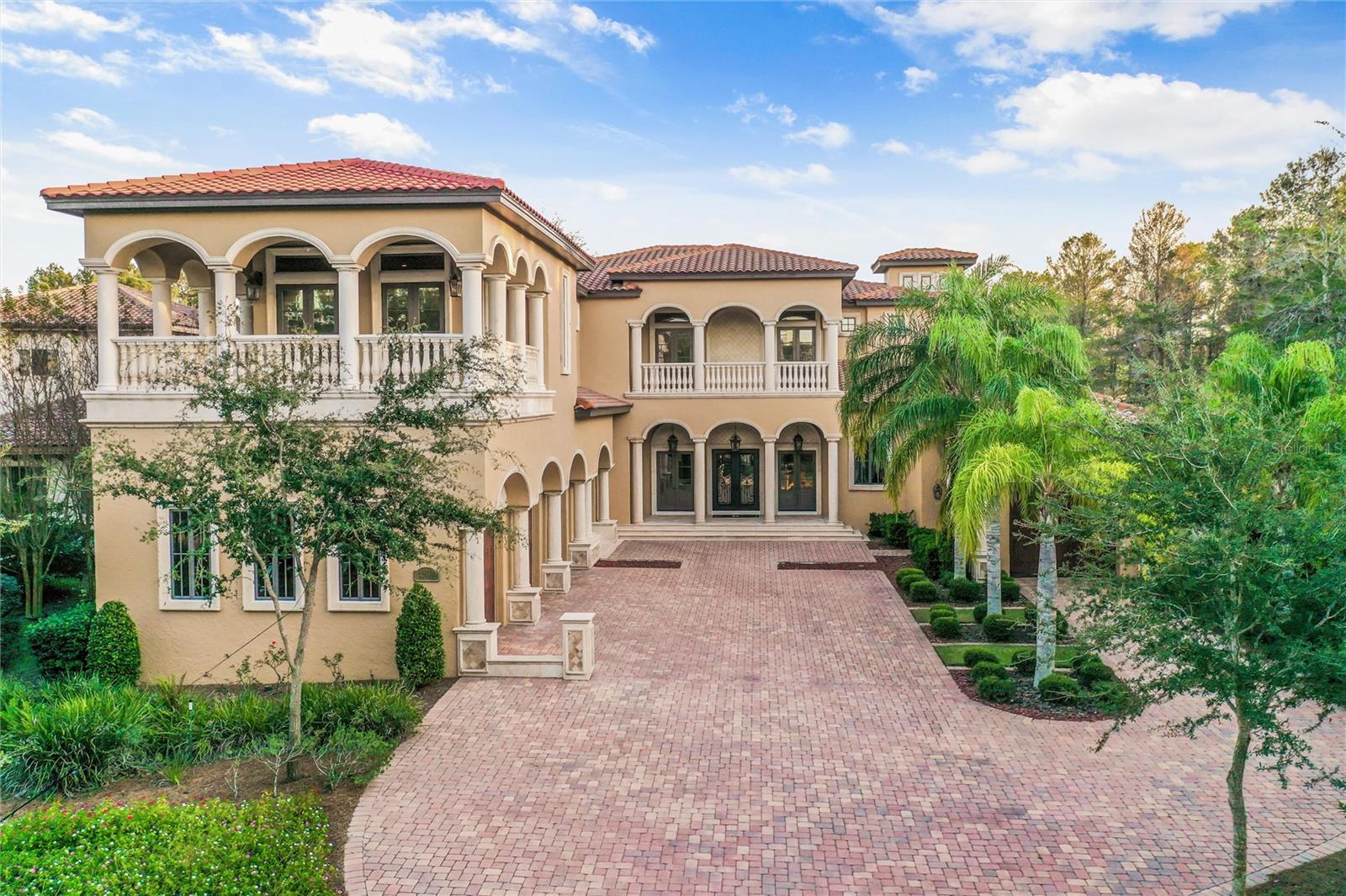 Welcome to this architectural masterpiece nestled in the stunning Bella Collina. This exceptional residence boasts 6 bedrooms and 7.2 baths, embodying the pinnacle of high-end living. The pool area is a haven of tranquility, offering a perfect blend of privacy and natural beauty. A sprawling lanai, adorned with various sitting and dining areas, surrounds the huge pool, complete with a relaxing fire pit and cascading waterfall. The expansive summer kitchen is complemented by a step-down area, perfect for serving cocktails to those seated on built-in stools within the pool. Craftsmanship is evident in every detail of this property, from the exceptionally detailed wood ceilings to the flowing wood floors. The house is strategically set back, featuring 4 front-drive garages and an additional 3 at the rear. Upon crossing the threshold of the double front doors, you are greeted by spectacular barrel ceilings, pillars, and captivating views of the oasis beyond. The open-plan design seamlessly connects the kitchen, dining area, and cathedral-height living room, with sliders opening to the patio. The kitchen is a chef's delight, equipped with top-of-the-line Wolf appliances, including 3 ovens. Custom cabinetry, granite surfaces, and a breakfast bar complete this culinary haven. The office exudes sophistication with maple wood details and an inlaid wood Greek key design flooring. The first-floor master suite is a sanctuary of luxury, featuring double doors that lead to the lanai and expansive windows overlooking the pool. A grand fireplace adds warmth and ambiance, while the spacious bathroom boasts double vanities, a sunken tub, and a large walk-in shower, all with travertine flooring. Custom closets with a central island add practical elegance to this retreat. Another bedroom and bathroom on the first floor complete the ensemble of this exceptional home, where every detail reflects the work of true craftsmen. Ascend in style with a wood-paneled elevator that adds a touch of elegance to this already exquisite residence. Upon reaching the upper floor, a loft space unfolds into a sociable games area with a balcony offering captivating views. Three additional beautiful bedrooms, each uniquely designed, one of which is a lavish master suite. Entertainment reaches new heights with a dedicated cinema room featuring reclining leather seating for a cinematic experience like no other. Adjacent to the cinema room, a vast room is transformed into a gym, complete with a kitchen/bar area and a convenient bathroom. For added convenience, a secret staircase discreetly descends to the garage courtyard, providing a seamless connection to the lower levels. There is the added bonus of three additional garages at the rear. This unique layout sets this property apart as the only one in the community with both front and rear access. These garages can serve as a workshop, equipped for the crafting enthusiast. Above this is an annex providing a living room, a bedroom, and bathroom, creating a self-contained living space within the expansive property.
This truly one-of-a-kind home sits in this beautiful golf community with exceptional Club House with restaurants & great amenities, and close to Mont Verde Academy & Winter Garden shops.