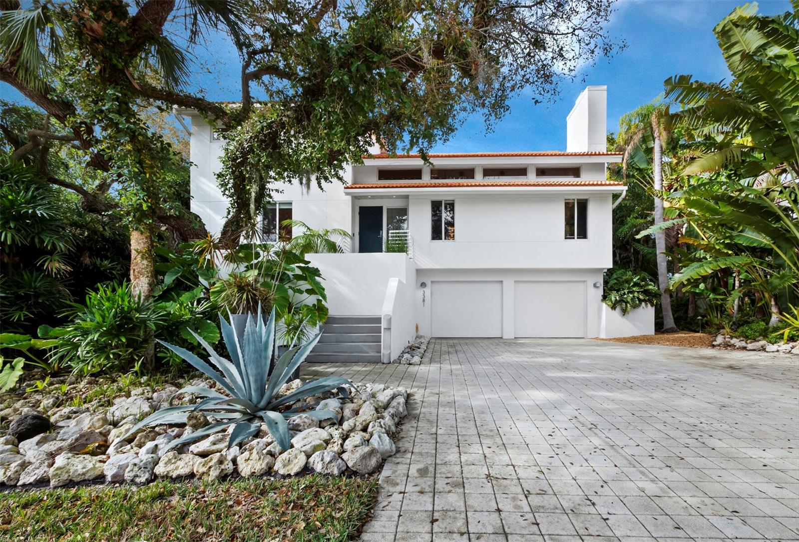 With award winning design and striking contemporary elegance nestled in the lush landscape of Longboat Key, this renovated modern home in a secure, gated community offers three levels of luxury and private access to Cranes Bayou with a fully equipped dock and 80 feet of water frontage. The interior spans more than 3,320 a/c square feet across an open layout with sight lines from the entry to the water, chic minimalist design, and modern architecture that showcases natural light and an ideal indoor/outdoor lifestyle.
On the main level, the elevated entry opens to a massive great room with a vaulted double-height ceiling that creates a dramatic sense of space. The living area flows seamlessly to the kitchen, ingeniously designed in a wraparound layout to promote flow on all sides, opening to the living room, adjacent dining room, and terrace overlooking the water. The kitchen boasts striking exotic wood cabinetry, expansive counter space, dual sinks, and premium stainless steel appliances including gas range, additional wall oven, integrated microwave, and side-by-side refrigerator freezer. Just past the kitchen, a full wall of floor-to-ceiling glass sliding doors open to a terrace that spans the entire width of the home for additional lounge and dining space overlooking the saltwater pool and bayou beyond. On the upper level, dual owners' suites offer luxurious retreats, each with double sliding glass doors that open to private water-facing balconies, large walk-in closets, and generous en suite bathrooms outfitted with chic modern features. Outside of the primary owners’ suite, a mezzanine overlooking the great room offers a private perch for relaxation or workspace. The ground level, currently arranged as a gym and den, is an expansive room with walk-out access to the pool and deck, where additional outdoor lounge space is protected by the three-story cage. Exceptional contemporary finishes, bamboo flooring, recessed lighting, and an elevator that serves three floors add to the luxurious comforts within the home. The landscape design and lighting are noteworthy enhancements that showcase both the home and the setting. Located within the private gated community of Bay Isles, owners also have exclusive access and use of the Bay Isles Beach Club on the Gulf of Mexico. Room Feature: Linen Closet In Bath (Primary Bedroom).