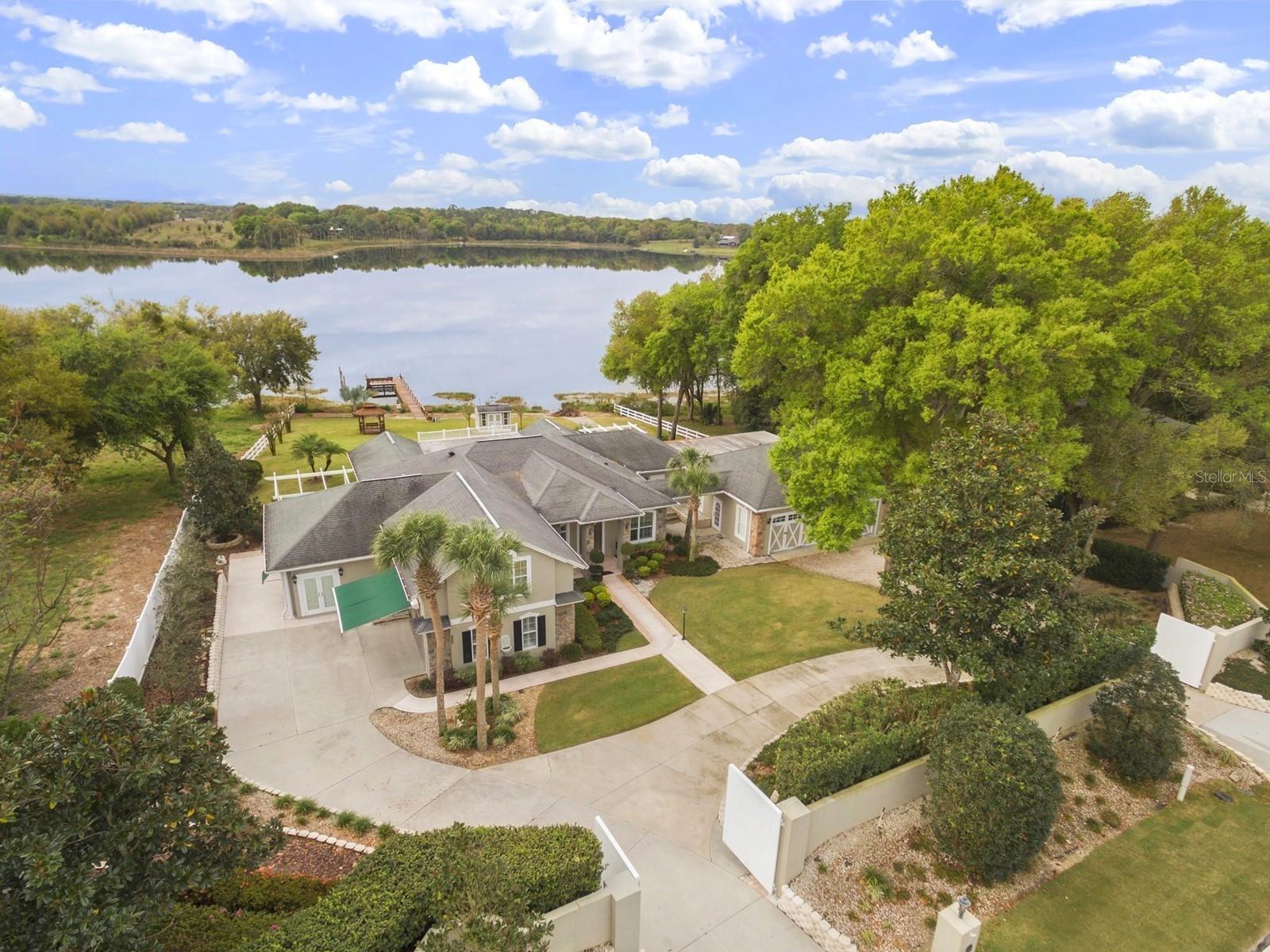 Tucked away in private seclusion, this stylish four bedroom, three bath custom built home sits majestically on 3.03 high and dry acres and 150 feet of direct frontage on 90-acre spring fed East Lake where residents enjoy bass fishing, boating, kayaking and gorgeous lakefront views. Gleaming white vinyl fencing and double gated entry takes you inside where you will be greeted by a circular driveway and a handsome retaining stone wall, exotic landscaping and beautiful curb appeal. The current owner reconstructed this home enlarging some of the existing rooms, adding a new master suite, three car garage, double entry foyer, recreation room, bonus rooms and a fourth bedroom with separate entrance. The views are beautiful from nearly every room of this comfortable, light and airy floor plan which includes a great room, office with gas fireplace, formal dining room, classy kitchen with Butler's pantry, breakfast room and Florida room with abundance of glass to showcase the gorgeous lakefront views. Attention to detail with wood and tile flooring, arched doorways, Plantation shutters, crown molding, double pane windows, radiant heat barriers, Styrofoam insulation and eight-foot French doors. An extensive outdoor lanai with hurricane shutters spans the back of the home and features attractive pergolas, summer kitchen with Jenn-air, gentle breezes and fabulous views. This property is further enhanced by a 34x22 covered shed, attractive free-standing shed with workshop, security cameras, 7500 kw generator, private boat ramp, dock, and lakeside gazebo. Newer updates include a new roof in March ,2023 by Eustis Roofing, brand new 5-ton and 1-ton air conditioner with ten-year warranty, new hot water heater and freshly painted exterior.  City water and Comcast services available featuring internet, cable, burglar and fire alarm. You will be happy here.