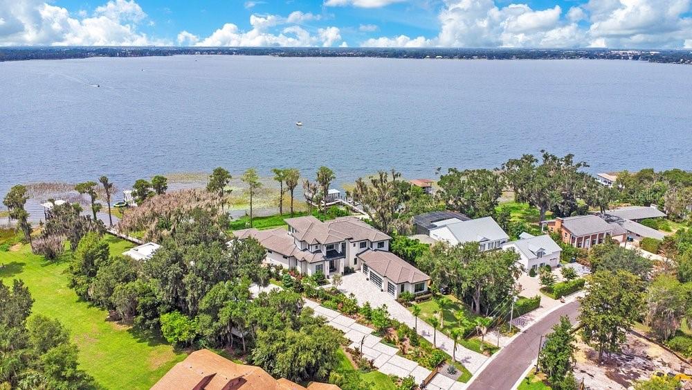 Welcome to an extraordinary lakefront estate on the prestigious shores of Lake Butler with 182 feet of water frontage, where timeless architecture, exceptional craftsmanship, and resort-style amenities come together in one of Windermere's most coveted locations. Built in 2024 and spanning approximately 6,900 square feet under air (10,400 total square feet), this custom residence sits on a rare one-acre homesite along the iconic, paved Second Avenue, renowned for its festive holiday displays, spectacular sunsets, and unmatched charm. Designed for both everyday luxury and grand scale entertaining, this 6 bedroom, 7.5 bathroom home offers en-suite bedrooms with walk-in closets, including a private first floor guest suite. The stunning primary retreat features a spa inspired bathroom and a private balcony overlooking the lake, creating the perfect setting to enjoy breathtaking sunsets and nightly Disney fireworks. The heart of the home is a designer chef's kitchen featuring exquisite Cristallo countertops, premium Miele appliances, and seamless flow into the expansive living and entertaining spaces. A dramatic floating wood staircase with a striking stone accent wall serves as an architectural centerpiece, while an elevator provides effortless access to every level. Additional highlights include a custom onyx sink in the powder bath, elegant 8-foot solid wood core doors throughout, motorized blinds, and laundry rooms on both the first and second floors. Step outside to experience a true private resort. The heated infinity edge saltwater pool features a unique acrylic glass viewing wall, allowing swimmers to enjoy underwater lake views unlike anything else. The expansive summer kitchen is equipped with two oversized Big Green Egg grills, a hibachi grill, and generous entertaining areas perfect for hosting unforgettable gatherings. A spacious game room with a full bar, dedicated fitness room, and professionally designed dog run complete the home's exceptional lifestyle offerings. Boating enthusiasts will appreciate the impressive two story private dock with multiple lifts, providing direct access to the famed Butler Chain of Lakes. Car collectors will love the oversized four car garage with an automotive lift, an additional golf cart garage, and an exceptionally long driveway offering abundant guest parking, a rare luxury on Second Avenue. Constructed with impact-rated windows and doors, spray foam insulation, and energy-efficient systems, this home was thoughtfully built to provide superior comfort, security, and efficiency. Combining impeccable design, world-class amenities, spectacular waterfront views, and one of the finest addresses in Central Florida, this remarkable Lake Butler estate represents a rare opportunity to own a nearly new custom home in one of Windermere's most sought after neighborhoods. Be sure to click on the virtual tour links.
