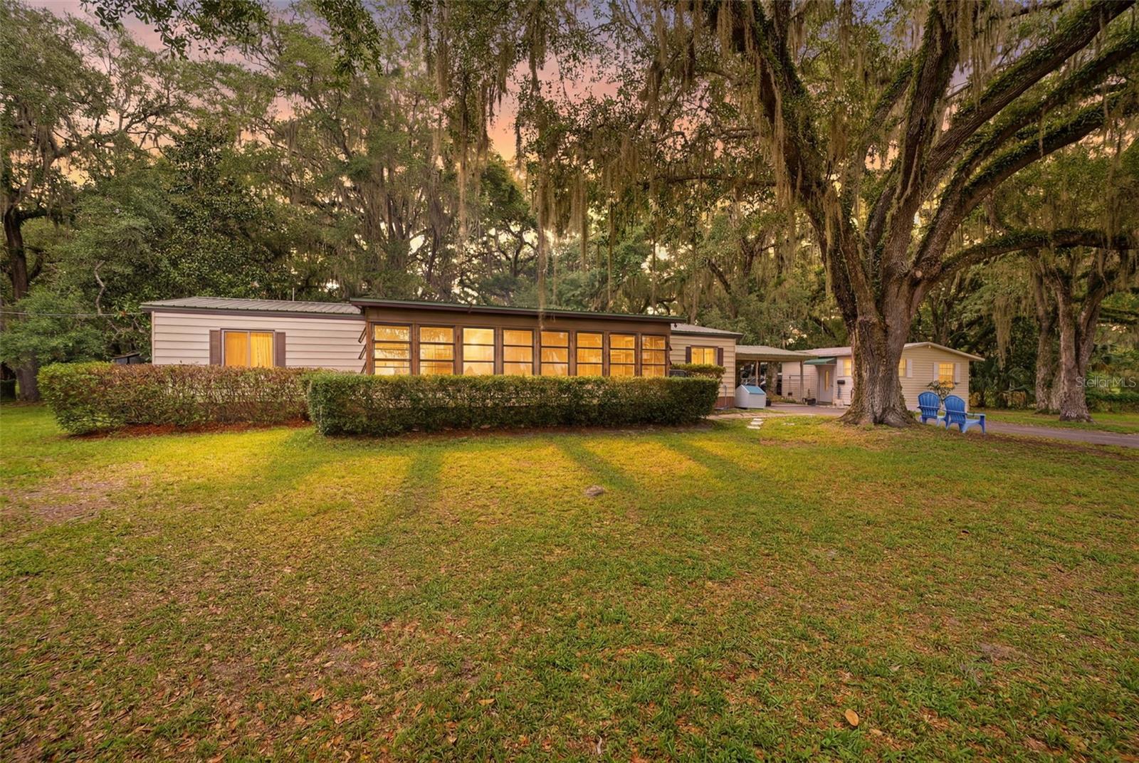 Under contract-accepting backup offers. Set on a fenced 1.85-acre property shaded by mature oak trees, this versatile 3-bedroom, 2-bath modular home offers a peaceful country setting with abundant space and the added benefit of a detached guest house. A gated metal farm-style entrance welcomes you onto the property, leading directly to the residence where a covered carport provides convenient parking. Through the side entry, you are first greeted by a spacious enclosed sunroom featuring well-kept carpeting, open beam ceilings, and walls of windows that showcase views of the front yard while filling the space with natural light. From there, the home opens into the main living area where vinyl flooring flows throughout much of the interior, complemented by vaulted ceilings that enhance the sense of openness. The living room offers a comfortable gathering space with wide windows overlooking the sunroom, abundant built-in shelving, and a built-in storage closet conveniently positioned near the entry. A flex room is also located near the front of the home and features vinyl flooring, built-in cabinetry, and large windows, making it ideal for a home office, hobby room, or additional living space. Continuing through the home, the dining area maintains the same flooring and vaulted ceiling, creating a seamless flow ideal for everyday living and entertaining. To the right, the kitchen combines functionality and storage with ample cabinetry, solid surface countertops, stainless steel appliances, a dual sink positioned beneath a window overlooking the rear Florida room, a walk-in pantry, and a breakfast bar for casual dining. Positioned toward the front of the home, the primary suite features vinyl flooring, natural light from multiple windows, a walk-in closet, and a spacious en-suite bathroom complete with a white pedestal vanity, built-in wall cabinetry, and a step-in shower with sliding glass doors. Bedroom 2 offers carpet flooring, a walk-in closet, windows for natural light, and private access to the shared bathroom. The guest bathroom showcases an updated design with a decorative framed mirror, single vanity, attractive tile accents, and a tub-shower combination with a sliding glass enclosure and grab bar. Bedroom 3 continues the comfortable layout with carpet flooring, a walk-in closet, windows, and direct access to a covered patio area. At the rear of the home, a spacious Florida room with light tile flooring, built-in bookcases, multiple windows, and double sliding glass doors opens to a raised wooden deck overlooking the backyard, creating a bright transition between indoor and outdoor living. Between the home and carport, a covered porch provides space for grilling, entertaining, plants, or relaxing outdoors. Nearby, the detached guest house adds tremendous versatility, offering its own living room, bedroom, and bathroom, making it well suited for visitors for extended stays. Several storage sheds positioned throughout the property provide ample room for tools, equipment, and outdoor necessities, and a recently added 2024 RV dump station enhances the property's functionality. This property is close to Lake Panasoffkee, where boating, fishing, and waterfront recreation can be enjoyed year-round; the Withlacoochee River, popular for kayaking and wildlife viewing; and the Withlacoochee State Forest, offering opportunities for hiking and outdoor recreation. Interstate 75 is also nearby, providing convenient access to shopping, dining, and surrounding communities.