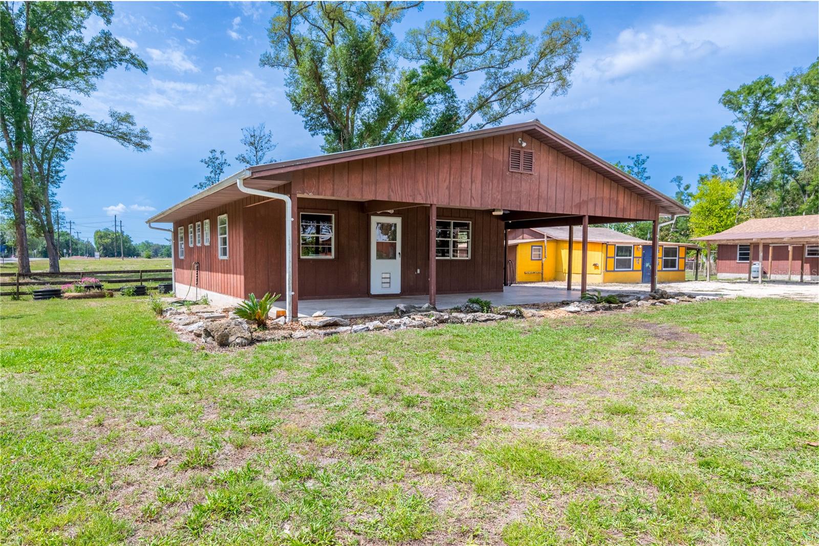 Single-Family Home with Guest House or Multi-Family / Income-Producing Opportunity in Chiefland, Florida. Beautiful country living with income-producing potential! Don’t miss this rare opportunity to own a versatile property featuring two cabin-style homes on approximately one acre ideal for single-family living with a guest house, multi-family use, or rental income. The property is fully fenced and cross-fenced, offering flexibility for livestock or additional use. In total, there are seven structures: two homes, a clubhouse, barn, shop, and two carports. Utilities are well established with three septic systems, one well, and underground electric throughout. Each home has its own 200-amp panel, while the clubhouse and shop have 100-amp panels, and the barn has a 110-amp panel. The well has been recently upgraded with a new pump and tank and provides excellent water. The land adds both beauty and value, featuring mature pecan, orange, and lemon trees, along with young pomegranate and kumquat trees. An electric gate at the entrance enhances both convenience and security. Both homes feature raised concrete foundations with wood framing, reflecting solid construction and durability. The front home offers a two-bedroom, one-bath layout with a utility room, functional kitchen, and comfortable living area, along with spacious front and side porches. Totaling 1,554 sq ft (984 sq ft H/C), it includes an efficient gas fireplace for heating and a wall A/C unit for cooling. While central air was previously installed, the ductwork remains, allowing for easy reinstallation if desired. The back home includes two bedrooms, one bath, a kitchen, and combined living/dining area, with both front and back porches. Totaling 856 sq ft (656 sq ft H/C), it is equipped with a wall A/C and electric heater for reliable comfort. A new roof installed in January 2026 adds peace of mind. High-speed Wi-Fiber internet in both homes. The approximately 1,000 sq ft clubhouse, originally a deer camp on the Suwannee River and relocated to the property, includes a shower, sink, and toilet, along with its own septic system and 100-amp panel. While it could use some TLC, it remains functional and offers potential for additional living space or other uses. Enjoy peaceful Levy County living just minutes from the Suwannee River, approximately 20 minutes to the Gulf, and only 6 miles to Chiefland for shopping and everyday needs. Located within a rural commercial node, this property could present future rezoning potential, further enhancing its investment value. Whether you’re looking for a primary residence with a guest home, a multi-family setup, or an income-producing investment, this unique property delivers flexibility, functionality, and long-term potential.
Agent Comments: Dimensions, square footage and other property details were obtained from DCPA and should be verified to satisfy buyer. It is buyer's responsibility to verify, by survey, exact dimensions, acreage, corner markers and elevation. Buyer should also complete their due diligence to check zoning and allowable uses of property with local governing authorities. Red boundary lines are estimates only. Total heated/cooled and living square footage reflects the combined total of both residences on the property.