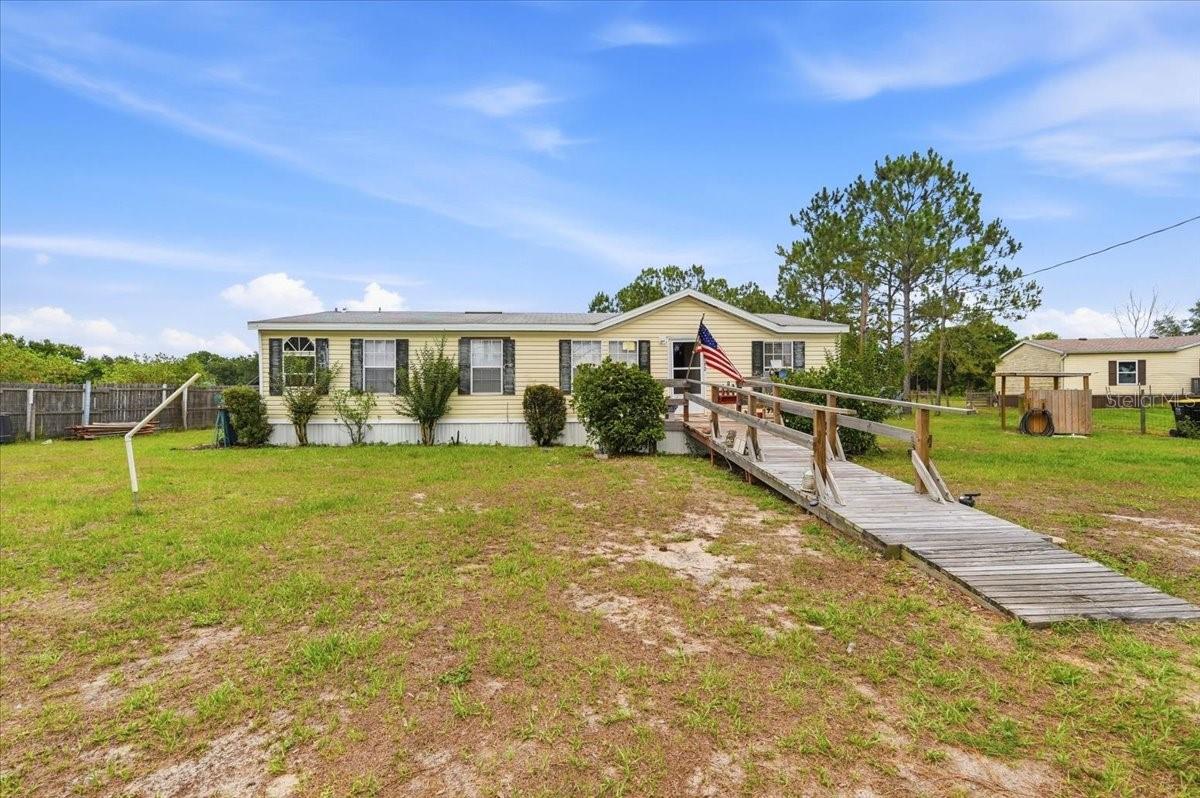 This 3 bedroom/2 bath manufactured home offering approximately 1,296 sq. ft. of living space on a 1 acre corner cul-de-sac lot. The home features a kitchen with wood cabinets, laminate countertops, and SVL flooring, followed by a spacious living room, dining area, and an open breakfast nook/mudroom just off the back entrance. All bedrooms are carpeted and include built-in storage, while the primary suite offers a large soaking tub, separate shower, and vanity with a wood cabinet. A dedicated laundry room adds everyday convenience.
Outside, the property features a detached carport, wide front yard with an accessibility ramp, and a fenced backyard with an above-ground pool, open patio, and barbecue area. Additional improvements include a rebuilt rear deck with double staircase, a newer heavy-duty front ramp, a 10x12 storage shed, and a pole barn. A 5-year-old roof and HVAC system, recently replaced well pump, and a water softener installed less than a year ago. Located in a cul-de-sac setting, this property offers space, functionality, and value.
