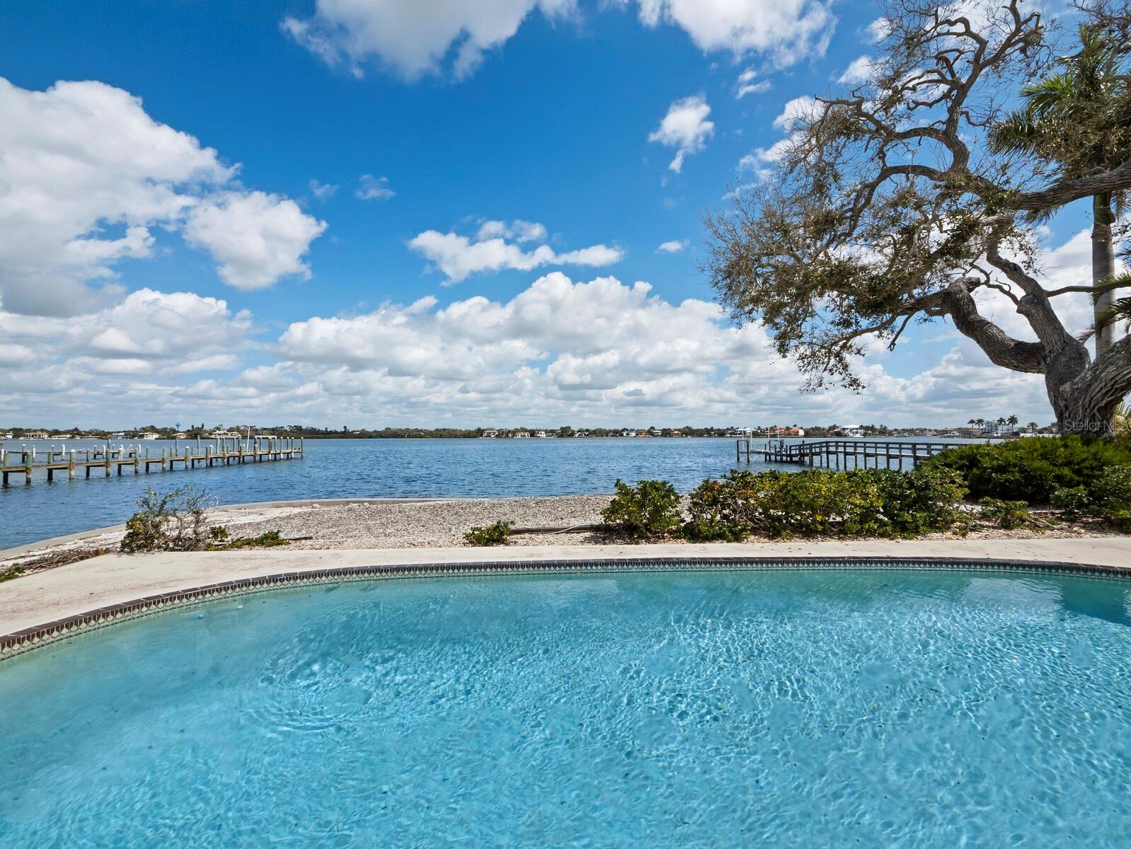 Under contract-accepting backup offers. A rare opportunity on Siesta Key’s Little Sarasota Bay. Positioned at the end of a quiet street in the established Midnight Harbor neighborhood, this 0.45-acre bayfront lot offers 287 feet of water frontage, approximately 92 feet along the bay and 195 feet along a protected saltwater canal, creating water on two sides and expansive open water views. The property is being offered for land value and presents an exceptional canvas for a new custom bayfront estate. The existing structure is not being marketed for renovation, allowing a buyer or builder to focus fully on designing a residence that maximizes the site’s orientation, water views and waterfront lifestyle potential. The bayside seawall was replaced in 2014, along with 20 feet of canal seawall. The protected canal frontage provides practical boating access with sailboat water and no fixed bridges, allowing direct navigation to the Intracoastal Waterway and Gulf beyond. The depth of the lot and the dual water exposure create compelling opportunities for architectural design, outdoor living spaces and waterfront amenities. The site is enhanced by mature coastal trees that contribute character and scale, elements often absent in newly created waterfront parcels. With nearly half an acre and substantial waterfront exposure, the property offers the scale required for a significant new coastal residence designed to modern building standards and elevated construction. Just minutes from Siesta Beach and offering convenient access to the mainland via the Stickney Point Bridge, the setting combines island privacy with proximity to Sarasota’s dining, cultural and entertainment districts. Waterfront redevelopment opportunities with this amount of bay and canal frontage on Siesta Key are increasingly limited, making this property a compelling investment for a builder, developer or buyer seeking to create a legacy waterfront home.