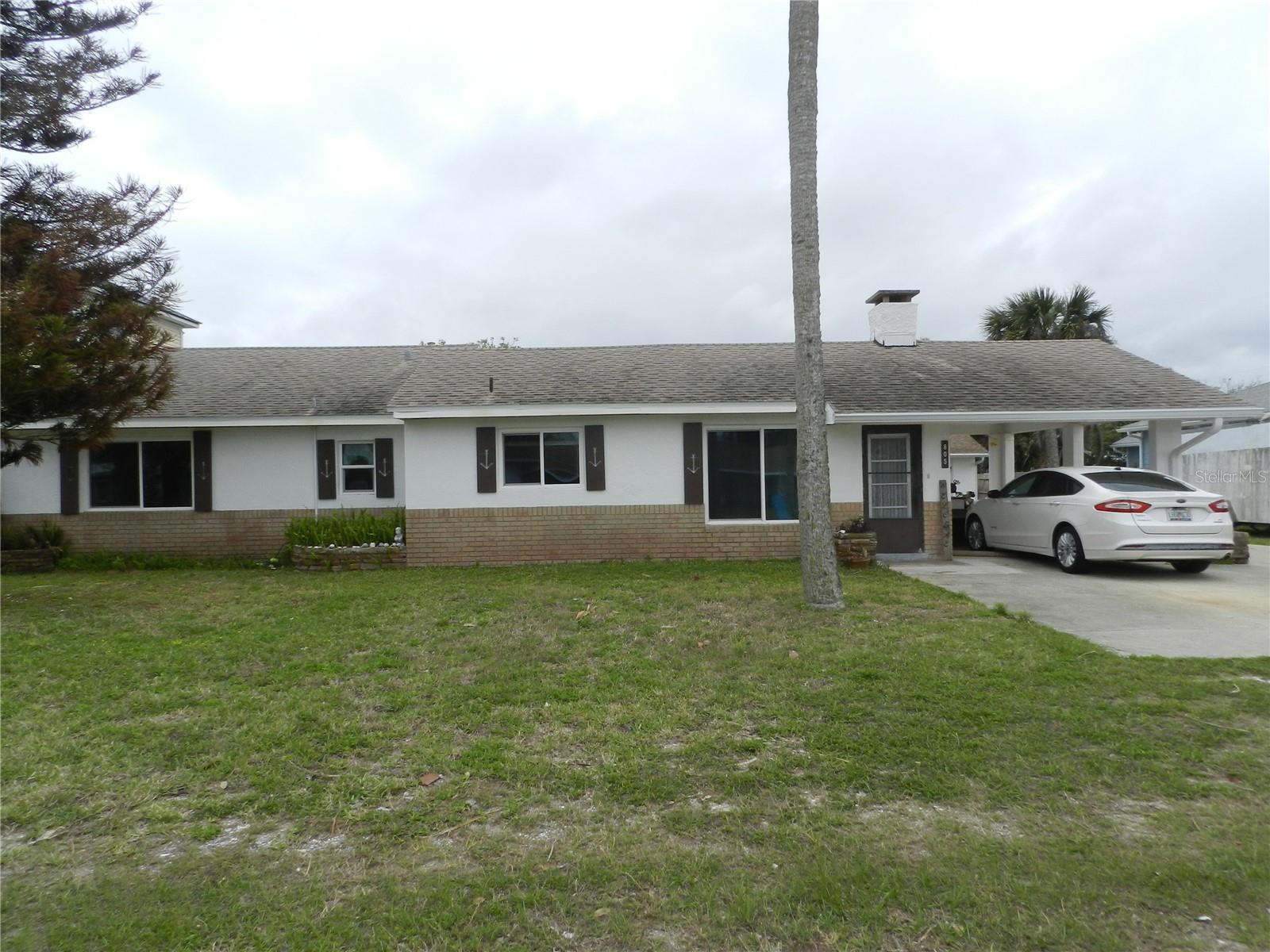 This property offers space and a prime location in the heart of New Smyrna Beach, just a short walk to the beach, Flagler Avenue, shops, restaurants, parks, and a grocery store. It includes two single-family homes. The main home sits on a rare double lot with privacy and parking for five cars. This 4-bedroom, 3-bath home features an enclosed porch, two patios, a carport, and a shed. The spacious eat-in kitchen connects to the dining room, while the living room includes a fireplace and built-in shelves. Three bedrooms have attached bathrooms, and there’s ample space for a pool. The outdoor shower is perfect after beach days, and the large lot offers plenty of room for entertaining, gardening, or relaxing. The second home is a 1-bedroom, 1-bath unit with an attached two-car garage, workshop, and indoor laundry. It can be used as a private retreat, office, guest space, or rental income opportunity.