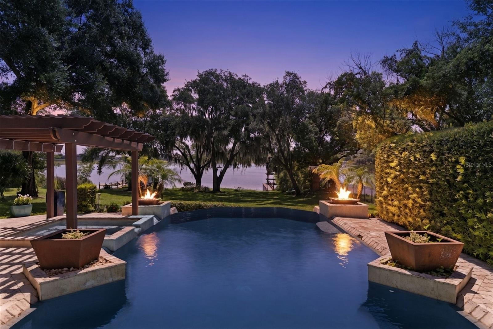 Welcome to 1629 Hempel Avenue, a private lakefront retreat set on more than one gated acre along Lake Olivia, an approximately 88-acre, spring-fed lake with private access. Located in the desirable Gotha/Windermere area, this exceptional property offers rare peace and privacy while remaining convenient to Southwest Orlando’s renowned theme parks, premier shopping, Downtown Orlando, Orlando International Airport, highly regarded schools, and the Florida Turnpike.

Mature trees, lush gardens, and thoughtfully designed outdoor spaces create a setting that feels secluded, established, and distinctly Florida. An antique church door provides a memorable entrance, setting the tone for a residence that blends refined finishes, distinctive character, and comfortable everyday living.

The main residence features four bedrooms, two full bathrooms, and an expansive open-concept living area designed for entertaining while showcasing beautiful lake views. The oversized great room offers multiple gathering spaces, including a billiards area, a large television and game-day space, a generous dining area, and an impressive chef-inspired kitchen.

At the center of the kitchen is an abundant quartz-topped island offering extensive workspace, seating, and a natural gathering place where guests can connect while meals are prepared. High-end flooring throughout the main home includes polished ceramic tile, travertine, and solid wood, while newer energy-efficient windows and doors enhance comfort and efficiency.

The primary suite is a magazine-worthy addition created as a private lakeside sanctuary. Cathedral ceilings, polished ceramic tile flooring, expansive lake views, and a flexible sitting or exercise area create an open and relaxing environment. Two oversized custom closets provide exceptional storage. The luxurious bathroom features floor-to-ceiling ceramic tile, quartz countertops, an oversized porcelain soaking tub, and a spacious walk-in shower room.

Four distinctive outdoor living areas invite you to enjoy the property throughout the year. Gather around the fire in the stone-paver garden area, relax within the private walled courtyard surrounded by potted plants and the soothing sound of a water fountain, or spend the day along the expansive backyard and private boat dock. The recently updated infinity-edge pool and heated spa overlook the lake, creating a resort-style setting for relaxing, entertaining, and enjoying unforgettable sunsets.

A separate guest residence adds tremendous flexibility and privacy. Complete with two bedrooms, two bathrooms, a kitchen, and a living area, it is ideal for multigenerational living, extended guests, or an on-site caretaker.

A private gated driveway and abundant parking accommodate multiple vehicles with ease. Combining two complete residences, more than an acre of lakefront land, exceptional outdoor living, mature landscaping, and private access to Lake Olivia, this one-of-a-kind estate offers a lifestyle rarely available in Central Florida.