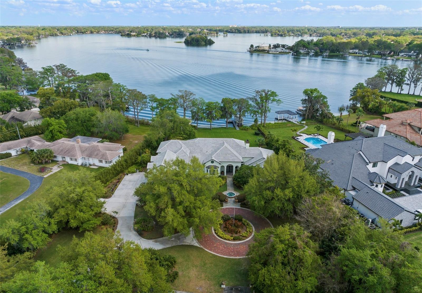 Embrace the epitome of luxury living with this extraordinary lakefront estate located in the heart of Maitland, where endless possibilities await. This expansive custom-built residence, spanning nearly 6,000 square feet, presents the rarest of opportunities. Whether you envision moving right in, updating the existing custom residence, or building anew on this coveted 2-acre high-and-dry lakefront lot, the potential is limitless.
The maturely landscaped driveway meanders to a circular paver roundabout leading you to the custom leaded glass entry doors. The foyer makes way to the expansive light filled formal living room boasting high ceilings, a wall of windows, a gas fireplace, and spectacular views of the lush backyard rolling gently down to unobstructed views of Lake Maitland.  The chef’s kitchen, equipped with custom cabinetry, a stunning copper stove hood, double ovens, and spacious countertops, makes way to the open glass breakfast nook inviting you to create a culinary haven tailored to your every desire. Adjacent to the kitchen, lies the formal dining room, complete with slate tile and majestic front garden vistas!
The first-floor primary bedroom, with its panoramic water views, dual walk-in closets, and spa-inspired bathroom, presents an opportunity to enjoy a luxurious retreat that exceeds your expectations. Just outside the primary bedroom is a stately office with custom wood paneling, a morning bar, and two-story bookshelves complete with a sliding ladder and French doors that lead to the covered porch with stunning lake views.  Downstairs, two additional bedrooms and a Jack and Jill bathroom offers ample space for family and guests, while the upstairs in-law suite, complete with a private balcony overlooking the lake provides a spacious family room area, and full kitchenette, making it the perfect retreat for your most coveted guests, they'll never want to leave their very own sanctuary!  The media and game room is second to none boasting an oversized wet bar with counter seating, an additional full bath and a generous closet behind hidden glass doors.
The oversized 4-car garage with a spacious storage room ensures that your vehicle and hobby needs will all be met. The nearby oversized laundry area and mudroom, complete with an additional full bathroom is beyond practical.  Relish in early morning sunrises and daily duck visits from your massive screened-in rear patio, and private composite dock with a covered boat lift assures you appreciate the extraordinary views of Dog Island, Isle of Sicily, and the Winter Park Racquet Club.  The original regulation-size tennis court, partly shaded by an abundance of Florida citrus trees, has the potential for pickleball courts, basketball or multi-sports court, offering a blank slate for creating your ultimate recreational space.
Situated walking distance from famed Luke's Kitchen and Bar, Antonio’s, and other fine restaurants, and with Winter Park’s--Park Avenue Boutiques and restaurants only 2.5 miles away, this extraordinary lakefront estate presents a once-in-a-lifetime opportunity to build or update your dream home in one of Central Florida’s most sought-after locations. Seize this chance to make your mark on luxury waterfront living and create a legacy that will endure for generations to come!