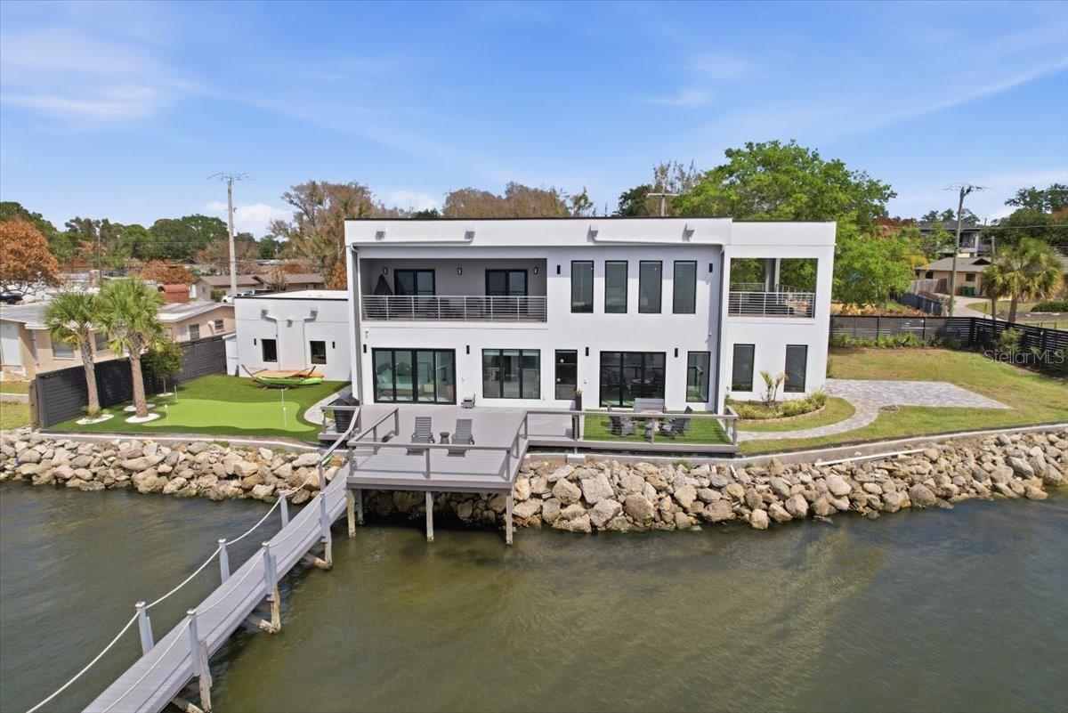 Modern Waterfront Masterpiece on Merritt Island with 142 Feet of Direct Indian River Frontage—this 2024-built, two-story luxury residence offers a rare combination of cutting-edge design, solid construction, and true Florida waterfront living. Built with full concrete block construction on both levels and topped with a commercial-grade roof, this home delivers both style and substance in a way that is virtually unmatched on the island. Featuring 5 bedrooms, 4 full bathrooms, and a 2-car garage, the property comes fully furnished and move-in ready, making it ideal as a primary residence or a high-end vacation retreat. Inside, you’ll find designer finishes throughout, including a sleek modern kitchen, custom built-in closets, high-end lighting, motorized shades, smart home features, and smart toilets in multiple bathrooms. The expansive upstairs primary suite is a true showpiece, offering a private covered terrace overlooking the water, a massive wraparound closet, and a spa-inspired bathroom with a dramatic wall of designer tile and luxury shower. Outdoor living is just as impressive, with a large side yard, putting green, and a covered boat dock with lift plus a jet ski dock—perfect for enjoying deep water access to the Indian River and quick routes to the Atlantic Ocean or cruising toward Cocoa Village. From your west-facing balconies, take in breathtaking sunsets along with daily sightings of dolphins, manatees, and pelicans. Located on prestigious South Tropical Trail, just minutes to Cocoa Village, approximately 45 minutes to Orlando International Airport, and about an hour to Disney World, this home offers a rare blend of privacy, accessibility, and lifestyle. Truly a one-of-a-kind, turnkey modern waterfront property in Central Florida.
