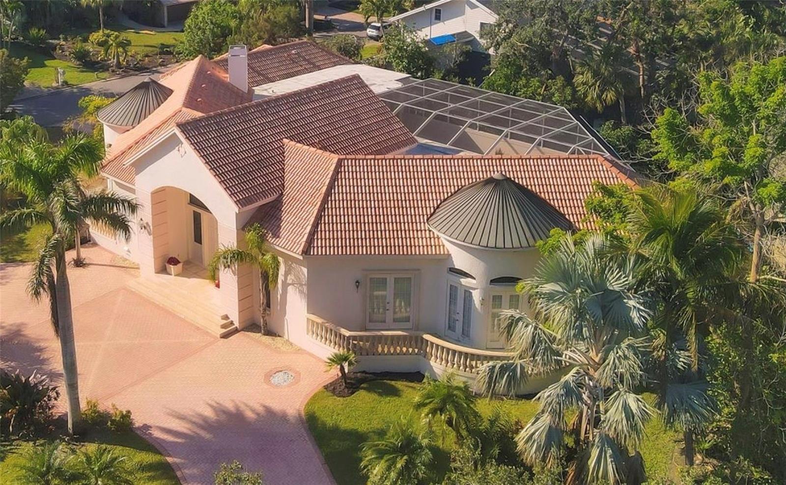 Immerse yourself in the tranquility of 5331 Siesta Cove Drive, a stunning jewel situated on a corner lot in the premier Siesta Key neighborhood. With a Mediterranean architectural aesthetic that radiates finesse, this residence features a stunningly crafted exterior adorned with European copper domes perfectly poised on an impressive 11’ elevation.  Upon entry, one is greeted by an expansive, open concept living space that magnificently fuses the indoors with the surrounding natural beauty. High sweeping ceilings create an enviable sense of space and light, while polished ceramic tile flooring adds a touch of allure.
Thoughtful consideration has been given to the common areas, such as the lavish living room, with an undeniable emphasis on comfort and sophistication. The episodic, broad windows let the glow of sunshine in, accentuating the elegant interior nuances.
The kitchen is a veritable chef’s delight, replete with spacious cabinetry, and granitic countertops that inspire culinary creativity. The generous breakfast nook provides an intimate and cozy venue for smaller gatherings and casual meals.
Outdoors, discover a secluded oasis where the skies, the greens, and the water merge to deliver a serene atmosphere. The sprawling deck, overlooking a large, elevated swimming pool, provides ample room for sun loungers, and al fresco dining setup, with outdoor kitchen.
The residence’s strategic location in Siesta Key, FL, rewards its residents with convenient access to local amenities and landmarks. Enjoy being a stone’s throw away from stunning beaches, upscale shopping destinations, refined dining venues, and outdoor recourses.
5331 Siesta Cove Drive offers an extraordinary amalgamation of luxury living and the calm of a beachside residence. Its matchless design, location, and surrounding serenity make it an idyllic haven for those seeking an unparalleled lifestyle in Siesta Key.