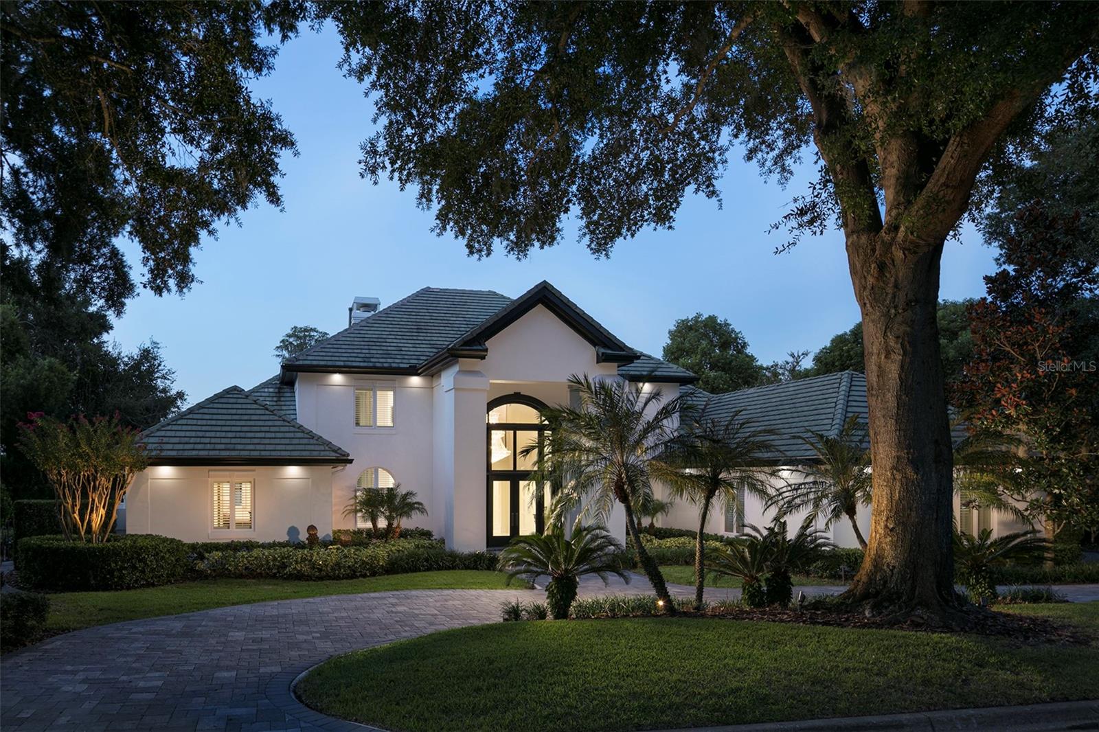 Within the gates of Isleworth Golf & Country Club, along the shores of Lake Chase, this exceptional lakefront offers a refined and contemporary waterfront lifestyle. Ideally positioned near the driving range and just moments from Isleworth’s racquet center, clubhouse, fitness facilities, dining, and pool, the residence combines privacy with convenience.Designed by renowned architect Mark Nasrallah, the home spans more than 7,100 square feet and showcases sophisticated detailing and elevated finishes throughout. A grand foyer introduces the residence with a sweeping floating staircase and dramatic tiered crystal chandelier, leading into the formal living room where soaring ceilings, dual chandeliers, a fireplace, and expansive lake views create an impressive yet inviting setting.Marble flooring transitions seamlessly into the home’s primary living spaces, where rich hardwood floors enhance the warmth of the open-concept kitchen, casual dining area, and family room. The kitchen is both functional and elegant, featuring an oversized island, custom cabinetry, quarried quartz countertops, and professional-grade appliances by Wolf, Sub-Zero, and Bosch. A contemporary, temperature-controlled wine room accommodating over 100 bottles adds a distinctive touch. Architectural millwork in a diamond pattern defines the dining space, while custom media built-ins in the family room enhance the home’s cohesive design. Both areas open effortlessly to the lanai and pool deck.The primary suite serves as a private retreat, complete with a sitting area, designer lighting, and a spa-inspired bath featuring a soaking tub, expansive dual vanities, and a large walk-in shower. Additional interior highlights include a modern office with custom built-ins and private pool access, as well as a spacious game room with a full bar and captivating water views. Outdoors, the covered lanai extends to a resort-style pool and spa, surrounded by generous lounging areas and complemented by the private boat dock - creating an unparalleled setting for boating, entertaining, and year-round enjoyment in Florida's tropical climate.