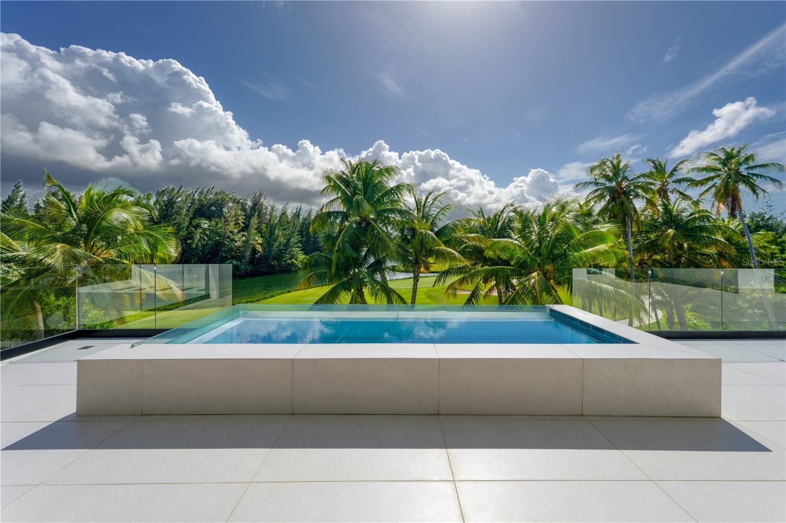 One or more photo(s) has been virtually staged. Set within the exclusive Four Seasons Resort and Residences in Rio Grande, Puerto Rico, this contemporary estate blends refined architecture with expansive interiors and serene lake and golf course views just moments from the Caribbean Sea.  Positioned on approximately 0.7 acres, the residence enjoys a privileged setting within one of Puerto Rico’s most prestigious resort communities. The home is designed around light, scale, and seamless indoor-outdoor living, featuring 10,677 Sq. Ft. of interior living space defined by clean architectural lines. Soaring ceilings, ranging from 10'0" to an impressive 25'2", and expansive glass openings create open living areas that feel both sophisticated and relaxed. The main living and dining areas flow effortlessly toward the terraces and outdoor entertaining areas, capturing beautiful views of the surrounding landscape. The chef’s kitchen features custom cabinetry, elegant natural stone countertops, and a generous island designed for gathering. A well-appointed butler’s pantry offers additional storage and preparation space, ensuring effortless entertaining while maintaining the elegance of the main kitchen. A striking glass wine cellar serves as both a functional and architectural focal point. The residence offers five (5) ensuite bedrooms, each with its own walk-in closet, ensuring comfort and privacy for residents and guests. The primary suite opens to an expansive private terrace featuring a lap pool overlooking the lake and golf course, creating a tranquil retreat. The spacious primary bathroom enjoys the same peaceful views and includes a soaking tub, walk-in shower, and refined spa-inspired finishes. Additional living areas include a separate family room and a home office, offering flexible spaces for relaxation, work, and entertainment. Outdoor living is an integral part of the home’s design, boasting approximately 7,095 Sq. Ft. of covered terraces, balconies, and a rooftop deck. Landscaped gardens and an infinity-edge pool overlook the lake and fairways beyond, creating a peaceful setting surrounded by the natural beauty of Bahia Beach. Adding to the home's impressive scale is a 1,004 Sq. Ft. garage with space for 2 cars plus golf cart. Four Seasons Resort and Residences at Bahia Beach residents enjoy access to the world-class amenities of the Four Seasons Resort at Bahia Beach, a private oceanfront community set across more than 483 acres of preserved natural landscape between the Atlantic Ocean and the Espiritu Santo River. Resort amenities include two miles of secluded beach, the Robert Trent Jones Jr. championship golf course, the Four Seasons Spa and Wellness Center, multiple resort pools and a beach club, fine dining restaurants and lounges, tennis courts, a state-of-the-art fitness center, nature trails, water sports, and access to the nearby marina. With its rare combination of privacy, natural beauty, and legendary Four Seasons service, Bahia Beach offers one of the most exceptional resort lifestyles in the Caribbean. * Photos 21, 23, 24 and 25 are virtually staged and do not reflect the current state of the property. The terrace that connects to the bedroom in Photo 20 has been virtually staged and does not reflect the current state of the property.