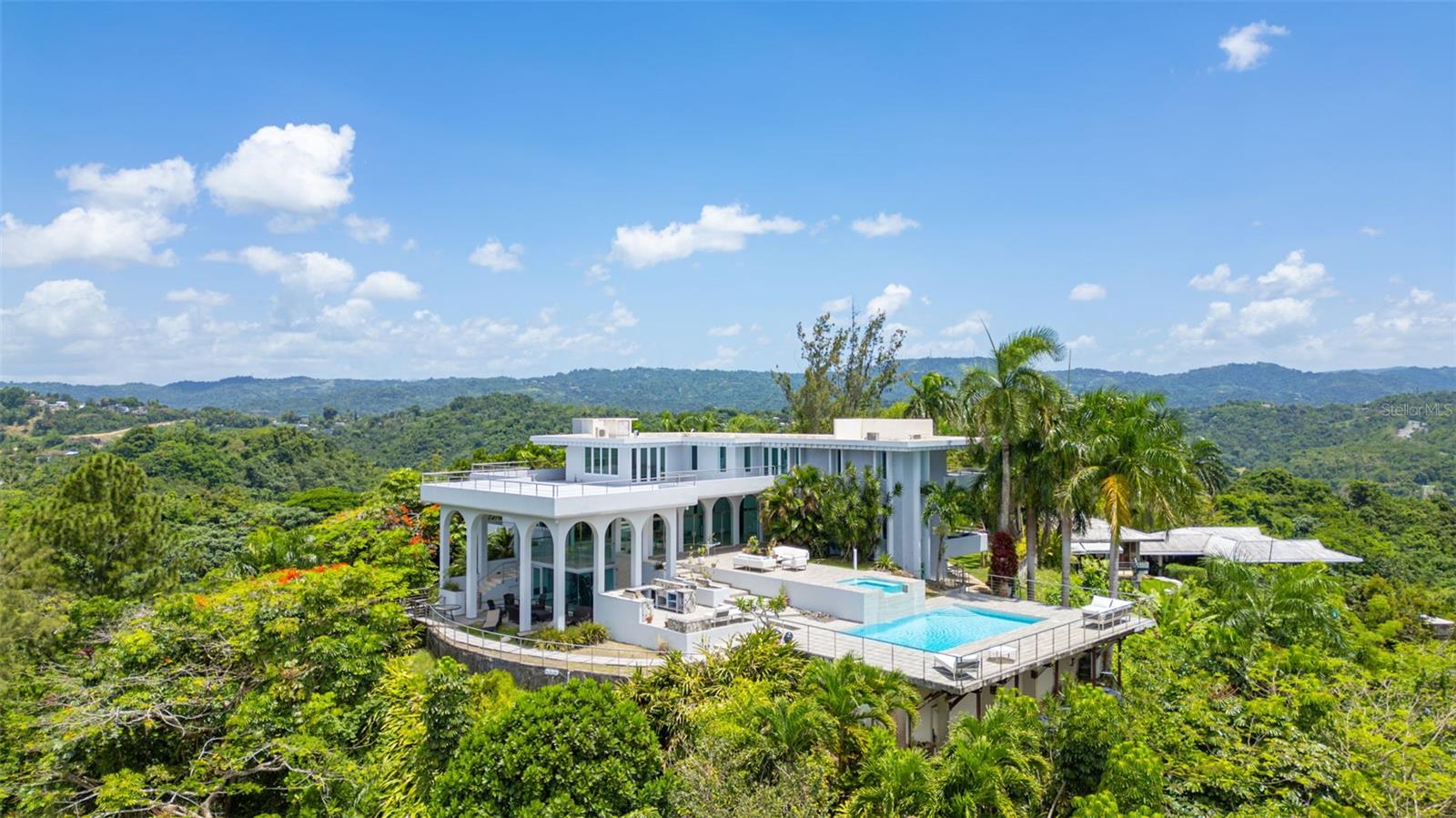 Rising above it all, this is the highest home in Beverly Hills, Guaynabo—with unmatched panoramic vistas in every direction. Set on 1.9 acres and wrapped in greenery, the property offers a rare sense of seclusion and privacy just minutes from the city. The layout is spacious and fluid, designed for both quiet enjoyment and entertaining. The pool and terrace sit at the edge of the hillside, framing the landscape. Floor-to-ceiling views follow you throughout the house, with every room opening to its own balcony or terrace. Downstairs, a large basement awaits your vision—perfect for a wine cellar, gym, or private retreat. With its elevation, size, and natural surroundings, this home delivers a unique blend of openness and intimacy in one of Guaynabo’s most elevated settings.