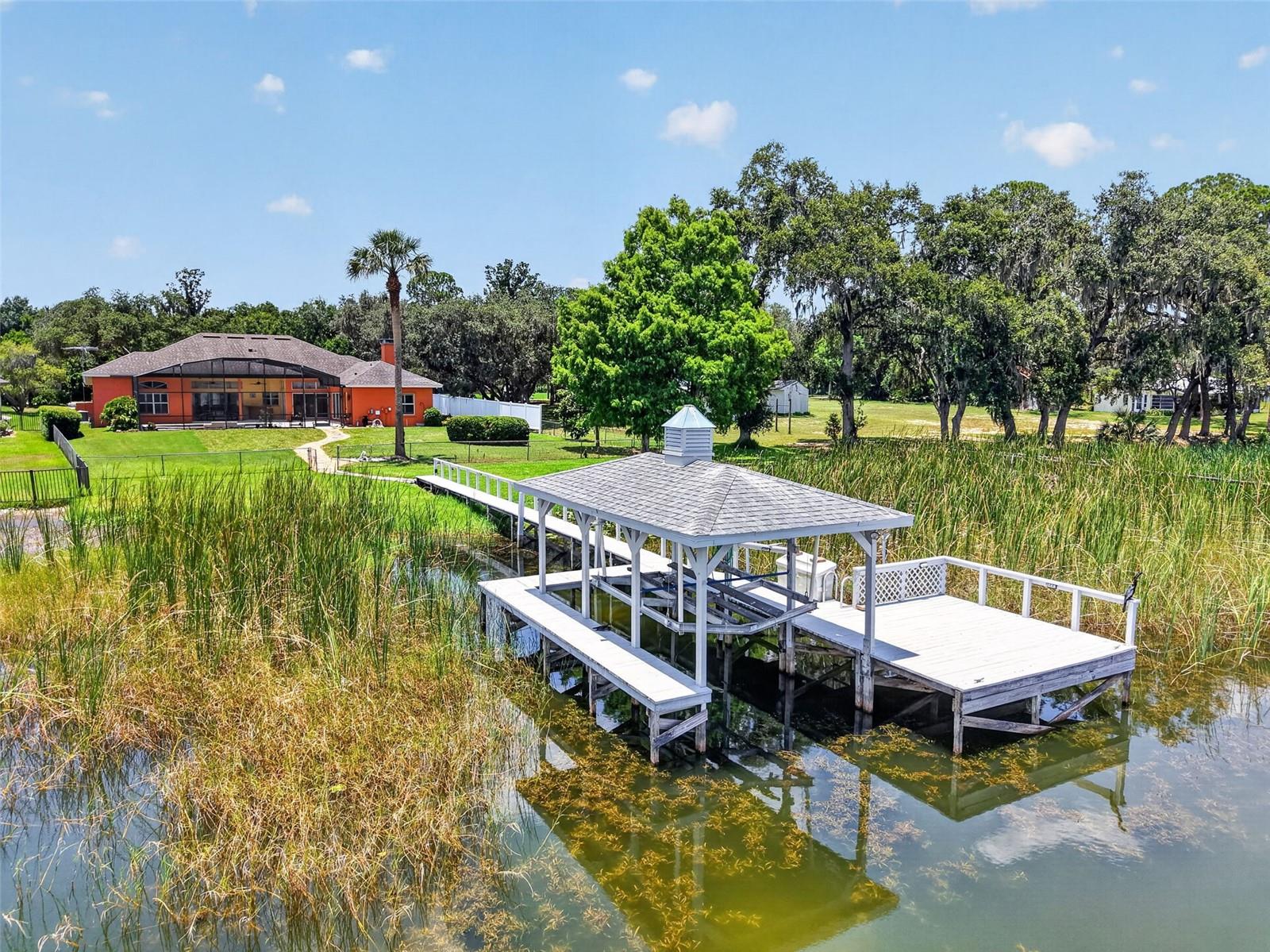 LAKE DORA / HARRIS CHAIN OF LAKES WATERFRONT WITH NO HOA Experience exceptional lakefront living in this stunning waterfront property nestled within the private, peaceful community of Squirrel Point on beautiful Lake Dora, minutes from the Deer Island Golf Club. From the moment you arrive, you'll be captivated by the property's breathtaking setting, where mature trees and lush landscaping create an unforgettable first impression. An expansive paver driveway and oversized three-car garage provide ample parking for family and guests, while the enclosed front porch welcomes you through elegant leaded glass double doors. Enter and be greeted by spectacular panoramic lake views that immediately steal the show. Designed to embrace Florida's indoor-outdoor lifestyle, this home features soaring ceilings, rich hardwood flooring, abundant natural light, and expansive sliding glass doors that seamlessly connect the interior to the outdoor living spaces. Recent updates offer peace of mind and modern convenience, including two HVAC systems (2024), water filtration system (2023), water heater (2024), freshly painted exterior (2023), updated interior and exterior lighting (2025–2026), a new pool pump (2026), a refurbished dock (2022) and recently painted (2026). The thoughtfully designed floor plan offers both elegance and functionality. The living and dining rooms provide inviting spaces for entertaining, with large sliding doors opening directly to the screened pool lanai for effortless indoor-outdoor gatherings. The spacious kitchen is appointed with wood cabinetry, Corian countertops, dual pantries, a center island with prep sink, breakfast bar, and a sunny dining nook overlooking the pool and sparkling Lake. Open to the kitchen, the comfortable family room creates the perfect setting for movie nights or relaxing with loved ones. A dedicated home office provides flexible space for remote work, hobbies, fitness, or art studio. The oversized laundry room includes cabinetry, a utility sink, and direct access to the garage. A desirable triple-split bedroom layout offers privacy for everyone. The primary suite serves as a peaceful retreat, featuring breathtaking lake views, a walk-in closet, and direct access to the pool. The spacious en-suite bath includes dual vanities, tiled shower, deep soaking tub, and convenient shared access to the adjoining office. Bedroom two enjoys easy access to a full hallway bath, while bedrooms three and four share a private pool bath with a tiled shower. Outdoor living is truly extraordinary. The expansive screened lanai features a sparkling pool, covered entertaining areas, ceiling fans, and a convenient wet bar, creating the perfect space for hosting guests or simply relaxing while taking in the incredible waterfront scenery. Beyond the lanai, the fenced backyard leads to your private covered boathouse complete with a boat lift and spacious waterfront deck. Enjoy panoramic views stretching across Lake Dora to the skyline of downtown Mount Dora. Wake to spectacular sunrises, unwind beneath moonlit skies, watch the iconic Dora Queen cruise by, and marvel at rocket launches from NASA and SpaceX visible across Central Florida's eastern horizon. Whether you're boating throughout the renowned Harris Chain of Lakes, paddleboarding, kayaking, fishing, or simply relaxing on your private dock at sunset, this remarkable property offers an unparalleled waterfront lifestyle where every day feels like a vacation.