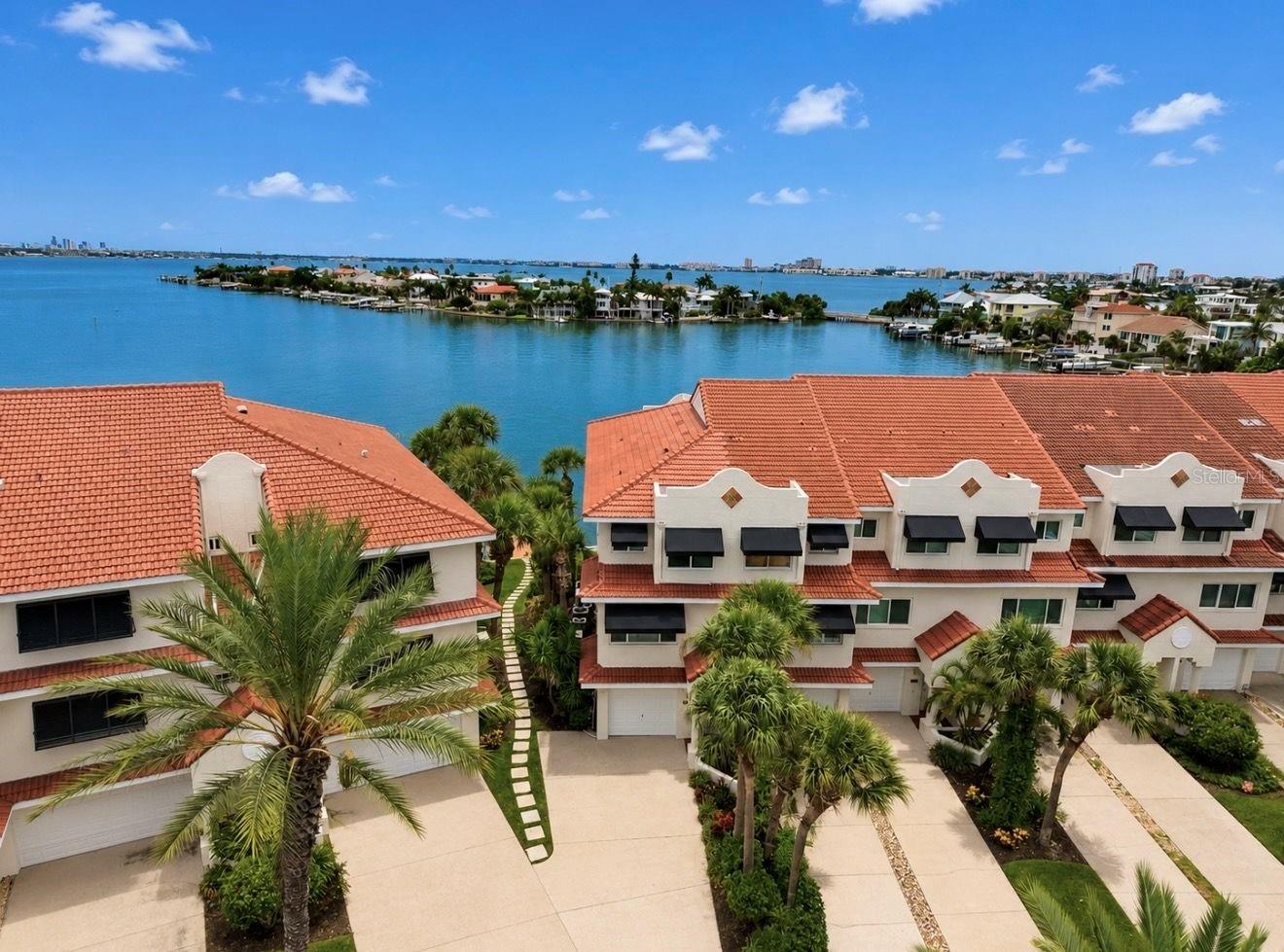 Virtually Staged. Rarely does a waterfront townhome offer this much flexibility, privacy, and value. This beautifully updated end-unit in the highly sought-after Mirabella community features breathtaking Boca Ciega Bay views, major 2025/2026 updates, and owner financing available for qualified buyers.  Wake up to spectacular sunrises and enjoy watching dolphins and manatees from one of three private balconies, offering outdoor living on every level. One of the home's standout features is the private lower-level suite, making it ideal for multi-generational living, long-term guests, or an older child who wants their own space. Complete with a full bath, wet bar, and a queen Murphy bed with built-in closet storage and shelving, plus direct access to the waterfront patio, it offers endless possibilities.  The main living level is designed for everyday living and entertaining, featuring an open floor plan filled with natural light, walls of glass showcasing the water views, and a beautifully updated kitchen with marble countertops, stainless steel appliances, induction cooktop, wine cooler, oversized porcelain farmhouse sink, and abundant cabinetry. The spacious living and dining areas seamlessly connect to the waterfront balcony, creating the perfect setting for morning coffee or evening cocktails.  Upstairs, the spacious primary suite is a true retreat with soaring ceilings, panoramic water views, a sitting area, two walk-in closets, and a beautifully updated ensuite bath. Also on the upper level are an additional bedroom, a full bathroom, and a convenient laundry area, providing privacy and comfort for family or guests.  Enjoy peace of mind knowing the major updates have already been completed, including a new tile roof (2025), new impact windows and sliding glass doors (2025/2026), fresh interior paint, and awnings. The oversized one-car garage and double-wide driveway provide plenty of parking for family and guests—an uncommon convenience for beach living. Storage is abundant with overhead garage storage, additional storage beneath the stairs, and attic storage above the primary bedroom. The home is also generator-ready, with the electrical infrastructure already installed for easy generator hookup.  
Mirabella offers the perfect coastal lifestyle with a heated community pool, fishing pier, kayak launch, day dock, guest parking, beautifully maintained grounds, and a pet-friendly community. The low HOA fee helps simplify ownership by covering water, trash, landscaping, and community maintenance.  Located just a short walk to the sugar-sand beaches of St. Pete Beach, waterfront restaurants, shops, and entertainment, this home combines the relaxed Florida lifestyle with the convenience of deep-water boating and easy access to everything the Gulf Coast has to offer.  Most of the furniture is negotiable, making it even easier to move in and start enjoying the waterfront lifestyle immediately.  Whether you're looking for a full-time waterfront residence, a seasonal retreat, or a home with flexible living space for family and guests, this exceptional property offers the perfect combination of waterfront living, modern updates, and an unbeatable St. Pete Beach location.