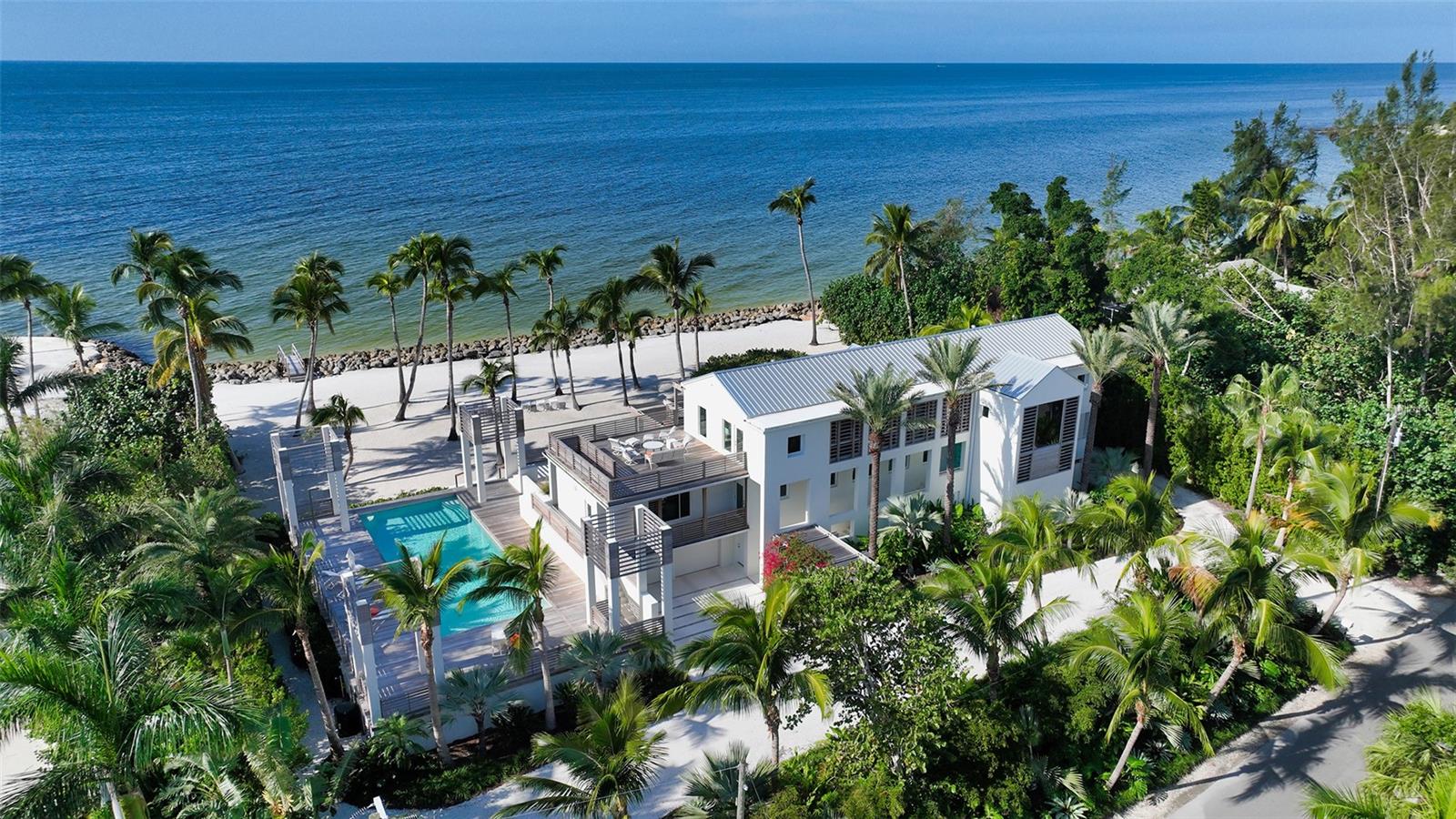 Experience a life like no other at this stunningly updated Siesta Key beachfront residence. Nestled amidst lush, Florida-friendly greenery, this private estate offers a unique and unparalleled living experience. With over an acre of property and an impressive 172’ of beachfront, this property is a true coastal paradise. Situated within the exclusive Sanderling Club, the only guard-gated, single-family neighborhood on Siesta Key, this home is a masterpiece of design and luxury. Originally envisioned by the renowned architect Robert Geddes, this residence was created to showcase the breathtaking beauty of the Gulf. From nearly every room in this four-bedroom, 5,000-square-foot home, you can gaze out over the shimmering Gulf waters and savor awe-inspiring sunsets. The interior is a study in contemporary elegance, with hardwood and Porcelain tile flooring, custom cove and sconce lighting featuring programmable color wheels, a three-stop elevator, and a neutral palette highlighted by natural wood accents. Sound-proofed walls ensure tranquility, while storm impact glass sliders and windows in various sizes enhance the home's distinctive architecture. Privacy is paramount in this beachfront estate, offering uncompromised luxury and tranquility. The current owners embarked on a comprehensive renovation from 2019 to 2022, updating every aspect of the home. Recent improvements include a new metal roof (2020/1), upgraded concrete exterior, state-of-the-art foam insulation, modernized electrical and plumbing systems, newer air-conditioning units, two dehumidifiers, and Hunter Douglas shades controlled remotely. A particular highlight is the sunroom, adjacent to the living room, where walls of glass provide panoramic beach views. With its tray ceiling and multiple access points to outdoor entertaining areas, this space offers an ideal escape. The gourmet kitchen, modernized and adjacent to the dining area and wet bar, features Quartz countertops with a waterfall edge, built-in Miele and Wolf appliances, sleek cabinetry, and a dining nook surrounded by bay windows, this chef's space is a masterpiece. Upstairs, the master suite is a private retreat with a separate sitting room, his and her bathrooms, and multiple closets. The guest suites, arranged in a split plan, enhance privacy and share a morning kitchen in the guest wing. A veranda runs the length of the house, and each bedroom has its own terrace, all connected to an oversized second-floor sundeck. The resort-inspired exterior offers endless options for relaxation and family enjoyment. Durable IPE decking surrounds the home on each level and adds architectural interest to trellises flanking the expansive patio area. The Olympic-sized, saltwater heated swimming pool has been resurfaced, and the inviting lounge and dining areas, along with the grilling station, are perfect for outdoor entertaining. Finally, its the proximity to the pristine beach in your own backyard, creates the ultimate beachfront living experience. This Siesta Key estate epitomizes the essence of luxurious coastal living, where every detail has been meticulously curated to provide a lifestyle of unrivaled beauty and comfort.