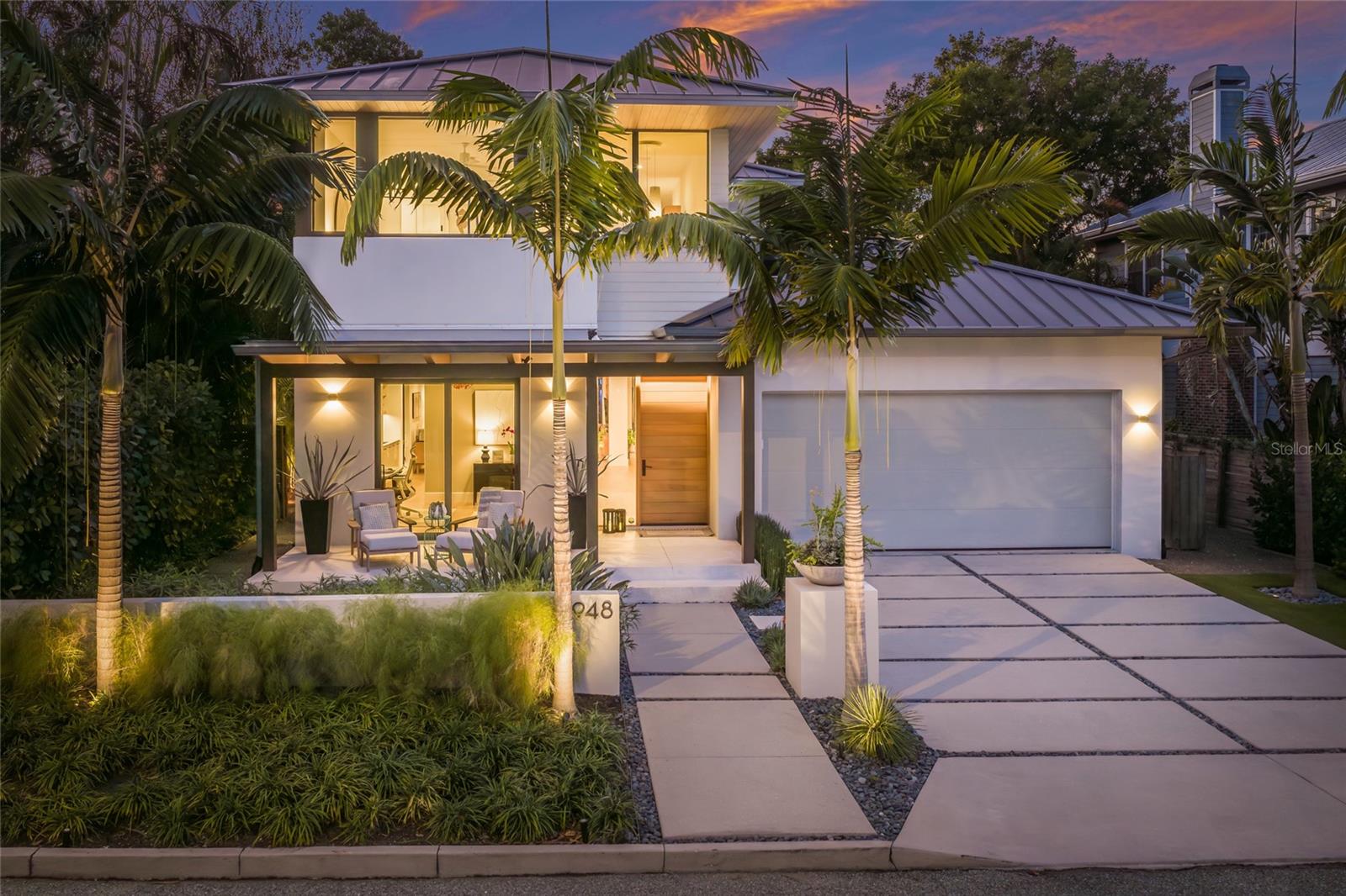 948 Citrus Avenue stands apart in Hudson Bayou by pairing custom-built modern design and Flood Zone X placement with award-winning architecture, dual owner suites, and a private resort-style outdoor living experience rarely found at this scale. Set behind clean modern lines and lush tropical landscaping, this West of Trail residence offers the privacy and livability today’s high-end buyers value most — including two owner suites that both connect directly to the extraordinary, oversized two-story screened lanai, creating a rare indoor-outdoor retreat on multiple levels. With a metal roof, no HOA, a cold plunge, sauna, and exceptional proximity to Selby Gardens, Southside Village, Burns Court, the Bayfront, and downtown Sarasota, the home feels like a private architectural retreat.
Inside, soaring ceilings, expansive glass, wide-plank Spanish White Oak flooring, and warm modern finishes create a refined interior that feels calm, bright, and intentional. The main living areas are open without feeling exposed, offering space for gathering, working, entertaining, and retreating, with strong connections to the pool, gardens, and outdoor living areas.

The kitchen is one of the home’s signature design moments. Recognized with SRQ Magazine Home of the Year Best Kitchen Gold honors, it blends custom cabinetry, quartz surfaces, premium Thermador appliances, an oversized island, generous prep space, and window wall that brings the landscape into the room. It is functional, memorable, and architectural — the kind of kitchen that makes the home feel custom rather than conventional.

The rear of the residence is where 948 Citrus Avenue becomes exceptional. The massive two-story screened lanai expands the way the home lives, creating a private outdoor environment with the feel of a boutique resort. It encloses the saltwater pool, upper balcony, tropical landscaping, and multiple places to relax or entertain year-round. The scale is rare, offering shade, privacy, comfort, and protection from the elements while making the home feel larger than its interior square footage suggests.

The dual owner-suite layout adds flexibility. The main-level owner suite opens to the lanai and pool area, creating an easy daily connection to the home’s best outdoor spaces. The upstairs owner suite provides separation and privacy for guests, family, or a second primary-style retreat. A flexible office/den and wellness-oriented garage area with cold plunge and sauna further support the way buyers want to live now.

Recognized as part of SRQ Magazine’s Home of the Year awards program, 948 Citrus Avenue carries architectural credibility that is felt throughout the home — from the kitchen and materials to the indoor-outdoor flow, privacy, and thoughtful use of space. More than a beautiful Hudson Bayou address, this is a design-recognized Sarasota modern residence with the location, outdoor living, flexibility, and practical advantages to stand out in today’s market.