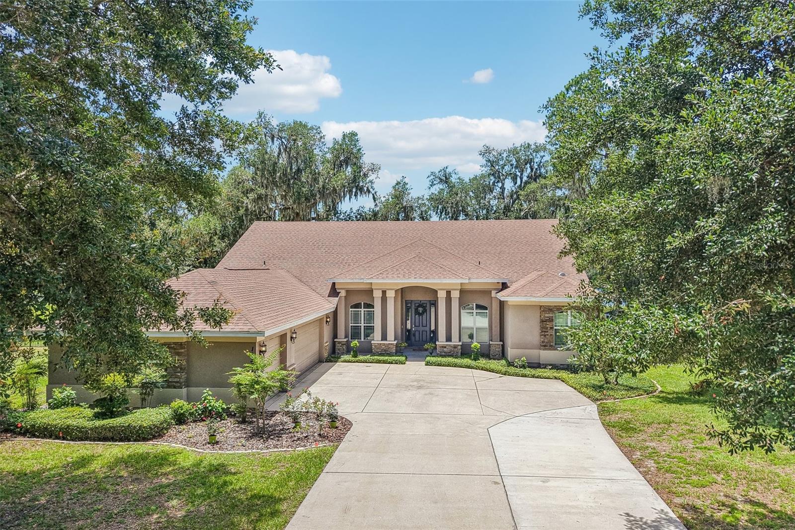 Located in a private gated community on a breathtaking 2.43-acre oversized conservation homesite with direct access and panoramic views of Shadow Lake is this exceptional 2-story residence. Mature oak trees, lush landscaping, and a courtyard-entry 3-car garage with coach lights create striking curb appeal, while the upgraded open deck design (no corner column) and pocket sliding glass doors maximize uninterrupted lake and nature views. The great room showcases a stunning custom wood-burning fireplace built with authentic bricks reclaimed from the historic streets of Ybor City, flanked by large side windows to frame the water views. A custom shiplap mantle with hidden electrical outlet, built-in lighting, and outlets on both sides of the fireplace add both beauty and function. A charming, lighted book nook creates a cozy retreat within the living space. Elegant 5¼" crown molding in the family room, dining room, and foyer, along with upgraded base trim, enhances the home’s architectural detail throughout. Luxury CoreLuxe 5mm waterproof rigid vinyl plank flooring in the San Fernando Hickory finish flows throughout the first floor, with extra material available for the staircase or upstairs bonus room. Storage is abundant with an extended, oversized pantry, spacious laundry room, and well-designed closets featuring swinging doors in the main bedrooms. The gourmet kitchen is a true centerpiece, featuring GE Café appliances, white painted maple shaker-style cabinetry with 42" uppers and crown molding, Level 3 “Alaska Delicatus” White Diamond granite countertops, custom under-cabinet lighting and outlets, a large breakfast bar with generous seating, and a separate breakfast nook. The first-floor primary suite offers tranquil lake views and a spa-inspired bath with a corner 6' garden tub, a fully enclosed shower with a Mr. Steam Thermasol SAA-240 steam unit (unit present, replacement needed for functionality), and a custom double vanity with designer mirrors. Outdoor living is equally impressive with covered and rear porches, an upgraded open deck, fire pit, outdoor kitchen with grill, private irrigated yard, mature oak trees. The spectacular 21’ x 17’ all-cedar Rainbow Clubhouse Package II play set come with a penthouse, monkey bars, rock wall, slide, fort, flower boxes, and hammock swing—professionally installed in November 2024 and backed by a lifetime cedar warranty. A whole-house generator and Energy Star aluminum-framed double-pane windows complete this remarkable lakefront retreat. Don’t miss your chance to make this gem your own—schedule a private tour today!