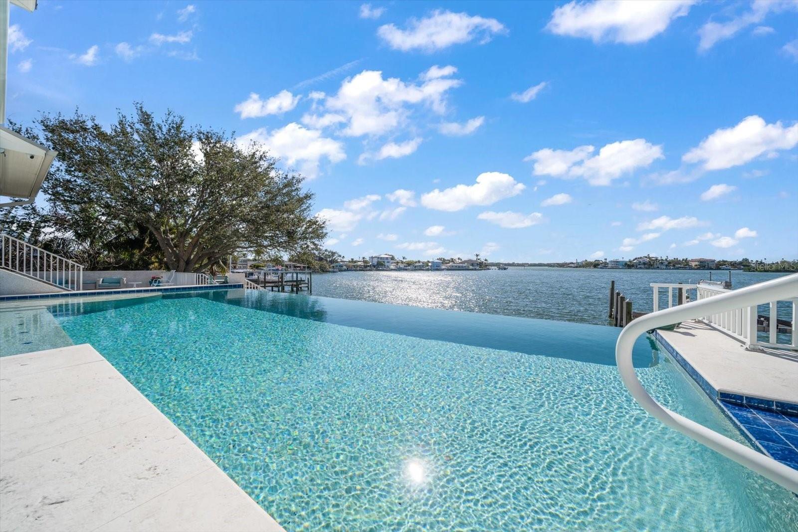 This one-of-a-kind waterfront paradise is perfectly situated on a triple lot. This home offers breathtaking southerly panoramic views of the elevated infinity-edge pool out to the expansive bay.  A true boater's paradise, the property features a custom dock updated in 2020 with a 20,000-lb lift in a protected cove great for wakeboarding, fishing, and paddle boarding. This location provides quick and easy access to the Intracoastal Waterway, Clearwater Pass, and the Gulf of Mexico. Inside this custom-built masterpiece, luxurious interiors and meticulous craftsmanship define every space. Upon entering, you are greeted by soaring 12-foot ceilings and sweeping southerly views that immerse the home in natural light.  The main living area is an entertainer's dream, showcasing 10-foot hurricane-rated sliding glass doors that seamlessly open to a spacious balcony perfect for enjoying sunsets and hosting gatherings.  Custom built-ins and a gas fireplace add elevated elegance, creating a warm yet sophisticated ambiance.  The chef-inspired kitchen is a culinary haven, featuring a large island, custom cabinetry, granite countertops, and premium appliances. This space combines style and functionality, making it ideal for everyday living and entertaining. This level also features a bedroom and pool bath. The bedroom features stunning views and access to the pool. The pool bath features a glass-enclosed shower with custom cabinets and quartz countertops. The third floor is dedicated to relaxation, with a luxurious primary retreat that includes a walk-in custom closet, and a private balcony overlooking the water. The spa-like primary bath is bathed in natural light, offering stunning views from every angle. The bath boasts a dual custom vanity and a glass-enclosed shower with a separate soaking tub.  Three additional spacious bedrooms boast picturesque southerly views, ensuring comfort and privacy for family and guests. Two bedrooms feature full baths and the 3rd bedroom/office has a half bath. The laundry closet is located on this level with an additional laundry room on the second level. The outdoor spaces are spectacular — the elevated infinity pool, fire pit, outdoor kitchen, and grilling area are all set against the backdrop of a beautifully paved pool deck, creating the ultimate outdoor oasis.  This exceptional home offers a unique 2,000-square-foot air-conditioned 6-car garage and a massive 44X14 carport designed to accommodate an RV, providing ample storage and convenience. The beautifully landscaped gardens and custom paver driveway enhance its curb appeal, while its elevated block construction ensures durability and significant protection against hurricanes. For added security and peace of mind, the property is equipped with custom hurricane impact glass, sunshades, a top-of-the-line Generac generator, and two tankless gas water heaters. Both are capable of servicing the entire home.  Experience a lifestyle of unparalleled luxury, privacy, and tranquility in this remarkable waterfront residence.  Schedule a private showing today.