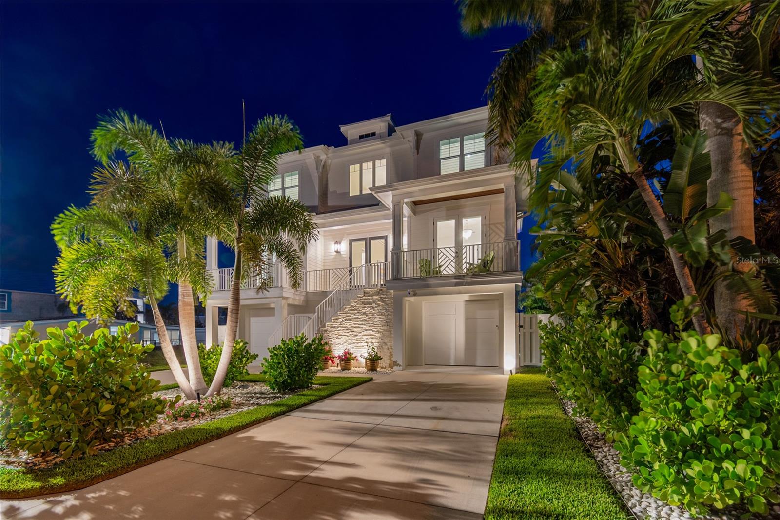 GORGEOUS COASTAL CONTEMPORARY ARCHITECTURE WITH BREATHTAKING WEST-FACING OPEN WATER VIEWS AND UNFORGETTABLE SUNSETS!  Lushly landscaped and fronted by a striking tumbled marble entry facade, this remarkable luxury residence delivers a striking curb appeal with the promise of what's inside.  A soaring 21ft-high foyer sets the tone for an exceptional great room plan, where fine wide-plank oak flooring, designer handrails and rich millwork flow seamlessly through every living area, all framed by fabulous waterfront views.  The spacious living room opens to a splendid covered waterfront balcony complete with wood ceilings, built-in speakers and electronic storm screens - the perfect perch for watching the water change color at dusk.  The sumptuous open chef's kitchen is a showpiece in its own right, boasting high-end appliances, built-in refrigeration, gas cooking and an island bar with seating for four; elegant quartz surfaces and a herringbone designer backsplash are beautifully complemented by coastal-white shaker style cabinetry.  A matching butler's pantry offers extensive storage and a built-in wine chiller, while the sizable dining area turns every meal into a waterfront occasion.  Two guest bedrooms offer tastefully-appointed full baths and their own private covered balconies.  Upstairs, through welcoming double doors, awaits the magnificent owner's suite - an elegant retreat that opens to an impressive private covered balcony with commanding water views and unforgettable western sunsets.  The resplendent owner's bath is an enviable escape from the day, featuring intricate designer porcelain flooring, a large walk-in closet system, lavish dual vanities, a fine stand-alone soaking tub, and a brilliantly-tiled walk-in rainshower.  The upper level also includes a graceful guest bedroom suite with a full luxury bath, plus an additional bedroom with two closets that's ideal as an office or den.  Out back, a huge 400sqft covered deck with wood ceilings, matching fans and built-in speakers sets the stage for effortless poolside dining and lounging.  An expansive pavered deck surrounds a stunning Pebbletec pool and spa with in-pool sunshelf lounging, while beyond it an updated seawall with riprap, a composite dock with pathway lighting, a 350lb manual lift and a 13,000lb boat lift with water and shore power put the entire waterfront at your fingertips.  The lower level features handsome shiplap finishes and extensive open space, ideal for storage, fitness or gaming.  This outstanding residence is further enhanced by a 3-stop elevator, electronic window treatments, plantation shutters, automated landscape lighting, an automated/remote-controlled pool system and so much more.  This extraordinary home makes living the waterfront dream easy, breezy, and unmistakably beautiful.