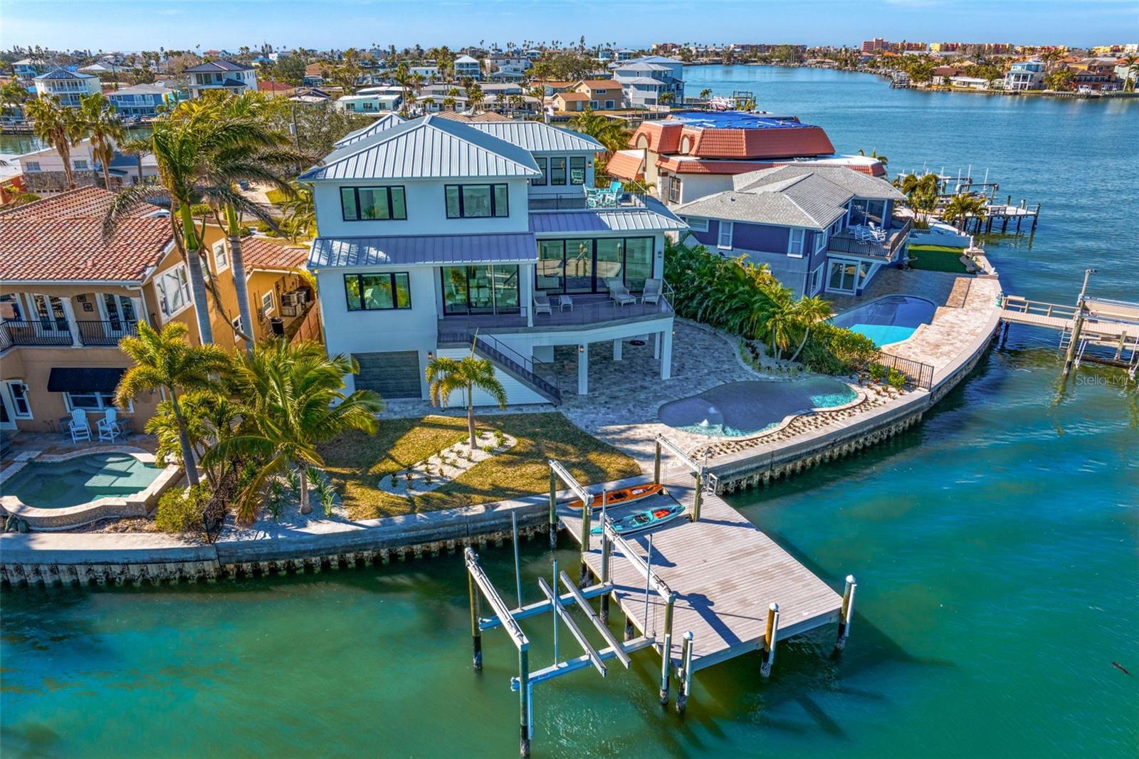 Exquisite Designer Waterfront Home – Experience the pinnacle of luxury waterfront living in this Inspiration Development Signature Home, a designer residence set on an incredible point lot with 103 feet of waterfront. Spanning over 6500 sq. ft. total, with 4180 sq. ft. of A/C living space, this stunning home features two primary suites, two guest bedrooms, five bathrooms, a six-car garage and elevator. This home is move-in ready, blending sophisticated style with exceptional comfort. The great room impresses with soaring ceilings and a 10-ft wall of stacking sliders, framing breathtaking open water views. The chef’s kitchen is a masterpiece. Boasting a stunning Marble prep island, custom white pecky cypress cabinetry, Monogram stainless steel appliances, and an oversized walk-in pantry. The dining area, surrounded by picture windows, offers sweeping water views and creates a unique and elegant dining experience. The main floor primary suite is a luxurious retreat with panoramic water views, his-and-her walk-in closets, and an en-suite bath featuring exquisite Marble details,  dual vanities, an immersive walk-in shower, and a soaking tub. A main-floor guest room serves as a perfect home office or private suite. Take the elevator to the top floor, where a spacious family room with a wet bar opens to an expansive balcony with stunning water views. The second floor primary suite boasts 180 degree water views, an en-suite bath, and a generous walk-in closet, while an additional guest suite offers comfort and privacy. Step outside to your resort-style backyard, featuring a covered lanai, freeform pool, travertine decking, and a composite dock with electric and water hookups. The dock features a 20,000lb boat lift and 10,000lb kayak lift and launch. As a boating enthusiast, you will love being able to walk out of your back door, hop onto your watercraft and live the island life to its fullest. All this and just a short stroll to the white sandy shores of Redington Beach. This home was built with top-tier materials for both elegance and durability, this home includes block construction, impact windows, Icynene insulation, TPO balconies, and a metal roof. Sellers are willing to entertain a sale of furnishings in a separate transaction. This waterfront masterpiece is the epitome of Florida luxury living—schedule your private showing today!