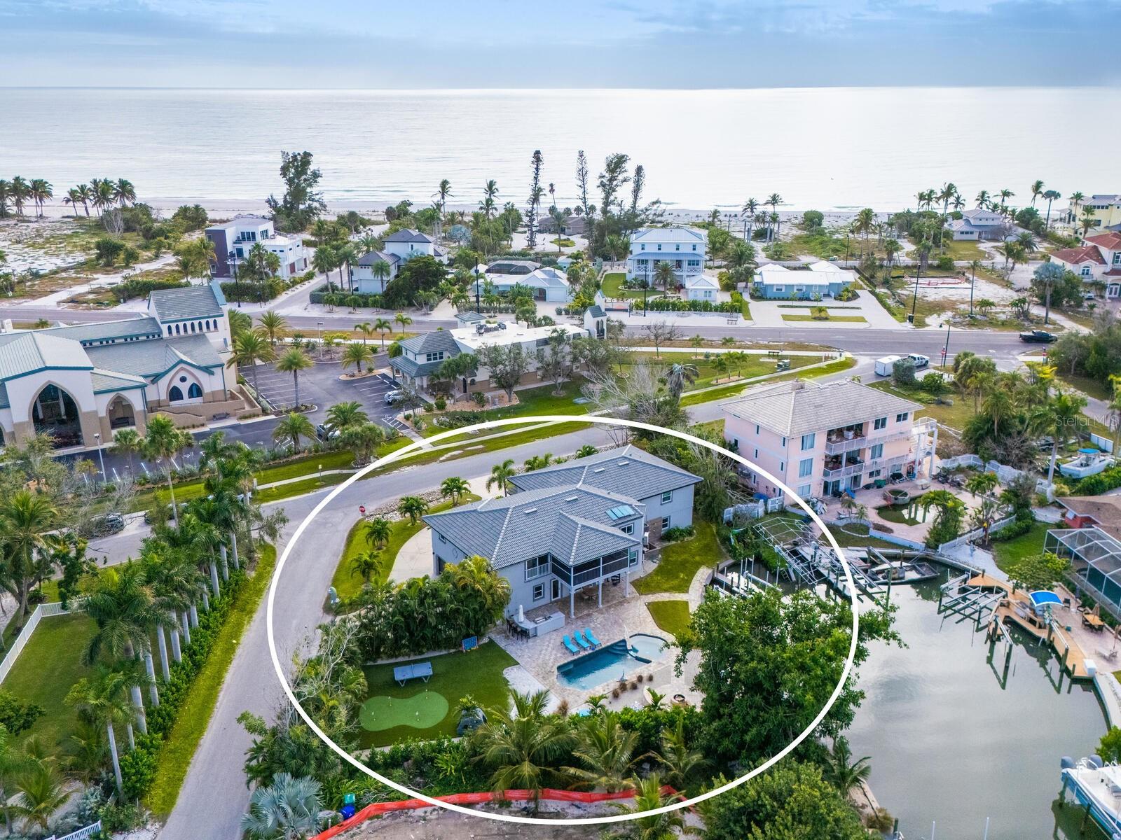 PRICE IMPROVEMENT! In the tranquil north end of Longboat Key, where Gulf breezes drift through the palms and the pace slows to a whisper, this extraordinary beach retreat captures the essence of refined coastal living. Positioned on nearly half an acre of canal front property and encompassing over 3,000 square feet of interior living space (more than 6,000 square feet total), the residence sits just across from the ultra convenient public beach access.  This unique residence offers the rare luxury of both boating and beachside lifestyles in one remarkable setting. Recently transformed through a stunning renovation and offered turnkey furnished, the five bedroom, three bath waterfront home showcases long, picturesque canal views and an effortless indoor outdoor flow.  A NEW ROOF in 2023 and new impact windows were installed in 2022 provide peace of mind. Vaulted ceilings and light-filled spaces that feel both expansive and inviting. At the heart of the home, the chef’s kitchen blends timeless style with modern performance, featuring classic shaker cabinetry, gleaming white quartz countertops, high-end white Café appliances, and generous island seating ideal for gathering. The primary suite is a private sanctuary of nearly 700 square feet, complete with dual walk-in closets and a spa-inspired bath designed for indulgence, including a dramatic double soaking tub with jets, fireplace and TV, a Moen technology-enhanced shower, and electronic Woodbridge toilets that elevate daily living with comfort and innovation. Each of the guest bedrooms offer sizeable walk in closets.  Step from the screened lanai off the living room down to a resort-caliber outdoor environment that rivals the finest destinations, where a heated pool and spa anchor the space alongside a putting green, waterfront fire pit, game area, and a beautifully pavered outdoor kitchen designed for effortless entertaining. For boating enthusiasts, the property is exceptionally equipped with a 10,000-pound boat lift and a second dock for added enjoyment.  Substantial non-conforming enhanced storage beneath the home and a spacious three-car garage provide versatility without compromising luxury, making this a rare waterfront compound where mornings begin at the beach, afternoons unfold on the water, and evenings are spent poolside under the stars.  Located a short distance to the Bridge Street Pier which offers ample dining, shopping and entertainment options, this residence truly is the ultimate beach getaway.