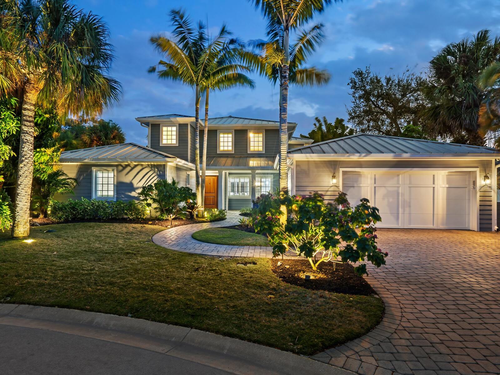 Luxury meets tranquility on the serene shores of Siesta Key. Nestled at the end of a quiet cul-de-sac, this coastal contemporary residence offers a 5-bedroom, 4-bath oasis overlooking 120 feet on the Grand Canal's deep boating water. From the front entry, you're greeted by a beautifully remodeled open-concept floor plan seamlessly connecting the great room, dining area, and chef-inspired kitchen. The kitchen is a haven for culinary enthusiasts with an oversized island, perfect for meal prep and casual dining, white shaker cabinets, quartz counters, and top-of-the-line JennAir stainless steel appliances. Enjoy casual meals in the breakfast nook with banquette seating; a planning desk is ideal for organizing your day in paradise. The main living areas boast floor-to-ceiling sliding glass doors open to the expansive screened lanai, offering breathtaking panoramic waterway views. Whether entertaining guests or enjoying a quiet evening at home, the lanai and waterfront patio provide the perfect setting to relax and dine alfresco while soaking in the balmy island breezes and picturesque sunsets, making it easy to host gatherings with family and friends year-round. provide The first-floor primary suite is a true retreat, featuring serene waterfront views and two walk-in closets. Glass French doors open onto the sparkling pool and spa area, creating a seamless indoor-outdoor living experience. Pamper yourself in style in the spa-like bath, a subway-tiled walk-in shower, and a luxurious Kohler-heated bubble massage air tub. Additionally, there are two quartz-topped vanities, a linen closet, storage, and a private water closet for added convenience. Two additional bedrooms and a full bath with modern fixtures are located on the main floor, providing comfortable accommodations for family and guests. The convenient laundry room offers added functionality and ease of living. Upstairs, a fabulous bonus room awaits, perfect for hosting guests or creating a private retreat for kids and teenagers. Custom built-ins house a media center, while two spacious bedroom suites offer walk-in closets and private baths with elegant quartz counters and designer fixtures. Step out onto the large balcony overlooking the waterway, where you can enjoy peaceful moments of reflection. The spacious outdoor area beckons for fun in the sun and shade. Shell stone pavers surround the south-facing freeform pool, creating an inviting oasis for relaxation and recreation to entertain friends and family. A composite dock and 10,000-pound boat lift are ready for watersport enthusiasts, offering easy access to the open waters of Sarasota Bay and the Gulf of Mexico. The fenced yard offers room for kids and pets to play safely, while lush tropical landscaping enhances the beauty and privacy of the property.
An extensive 2013 renovation includes a new roof, kitchen, baths, flooring, plantation shutters, plumbing, and concrete siding, ensuring modern comfort and style. In the evening, fabulous outdoor lighting illuminates the paver drive and tropical gardens, creating a magical, welcoming ambiance and enhancing the home's curb appeal. Siesta Key's world-famous crystal quartz sands and aqua waters await a few minutes away. Unique Siesta Village awaits with shopping and dining options to suit every taste. Discover the cultural richness of downtown Sarasota, with its array of restaurants, theaters, ballet, opera, museums, galleries, and shopping destinations, all just a short drive away.