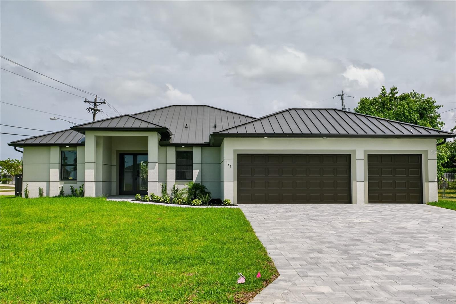 Welcome to elevated COASTAL living! Move-in-ready NEW CONSTRUCTION HOME (2026) complete w/ 2-10 HOME WARRANTY! Located in SW Cape Coral, offers NO FLOOD INSURANCE, durable METAL ROOF, 3-CAR GARAGE & CITY WATER & SEWER! $1,800-$2,400/year homeowners' insurance! Enjoy easy access to SKYLINE BLVD & PINE ISLAND RD, making commuting & daily errands easier! This CONTEMPORARY LUXURY HOME features SCREENED, HEATED POOL & SPA & 4 BEDS (2 primary suites) & 3 full BATHS, layout is ideal for EVERYDAY LIVING & ENTERTAINING! SCREENED LANAI provides PERFECT SETTING TO RELAX in SPA, SWIM in HEATED POOL, or HOST UNFORGETTABLE BBQs while enjoying THE BEST OF SWFL LIVING! Bright, open layout w/ LIGHT NEUTRAL TILE FLOORING throughout. IMPACT-RESISTANT DOUBLE DOORS lead into WELCOMING LIVING ROOM w/ 12-ft VAULTED CEILING & SLIDING DOORS TO LANAI. GORGEOUS CHEF’S KITCHEN showcases sophisticated CUSTOM CABINETRY w/ NATURAL WOOD-GRAIN finish paired w/ sleek WHITE FLAT-PANEL UPPER CABINETS. Warm cabinetry tone features elegant EUROPEAN OAK-style texture w/ organic grain movement. Crisp QUARTZ COUNTERTOPS & matching FULL BACKSPLASH complement modern palette, while UNDER-CABINET LED LIGHTING enhances the bright, open feel. Equipped w/ SS appliances, French-door refrigerator, microwave, smooth-top range & angular EURO-STYLE hood & dishwasher. Oversized ISLAND & minimalist HARDWARE-FREE CABINETRY. Built-in BUTLER’S PANTRY w/ warm WOOD-GRAIN cabinetry, sleek WHITE upper cabinets, QUARTZ countertops, under-cabinet lighting & built-in WINE REFRIGERATOR, ideal for BEVERAGE STATION, COFFEE BAR, or EXTRA STORAGE & PREP SPACE. DINING ROOM w/ bright, modern design, neutral tones & vaulted ceiling w/ recessed lighting that enhances open feel. LARGE PICTURE WINDOW brings in natural light & offers views of screened lanai & pool/spa. LARGE PRIMARY SUITE w/ sliding doors to lanai, WALK-IN CLOSET w/ BUILT-IN SHELVING & HANGING RACKS & LUXURIOUS PRIMARY BATHROOM w/ spacious WALK-IN GLASS SHOWER w/ floor-to-ceiling designer tile, rainfall showerhead, built-in bench & modern matte-black fixtures. Dual sink vanity w/ quartz countertops, sleek white cabinetry & contemporary lighting complements the spa-like design. Private water closet & generous natural light create BRIGHT & SERENE RETREAT! BUILT-IN CUSTOM CLOSET WHITE CABINETRY provides ADDED STORAGE & CLEAN, UPSCALE LOOK. SPLIT LAYOUT offers SECOND PRIMARY SUITE w/ POOL BATHROOM & TWO GUEST BEDROOMS w/ HALL BATHROOM for added privacy. Step outside to SCREENED LANAI w/ HEATED POOL & SPA, landscaped surrounding & FULLY EQUIPED OUTDOOR KITCHEN w/ BUILT-IN stainless steel BBQ GRILL, SINK, BEVERAGE REFRIGERATOR, GRANITE COUNTERTOPS & MODERN BACKSPLASH, ideal for OUTDOOR DINING & ENTERTAINING! PAVER FLOORING & CEILING FAN create COMFORTABLE SPACE for YEAR-ROUND ENJOYMENT. LAUNDRY, 3-CAR GARAGE & long-lasting METAL ROOF complete HOMES' FUNCTIONAL FEATURES. Don’t miss this oversized CORNER LOT w/ PRIME ACCESSIBILITY & unbeatable SWFL convenience!
