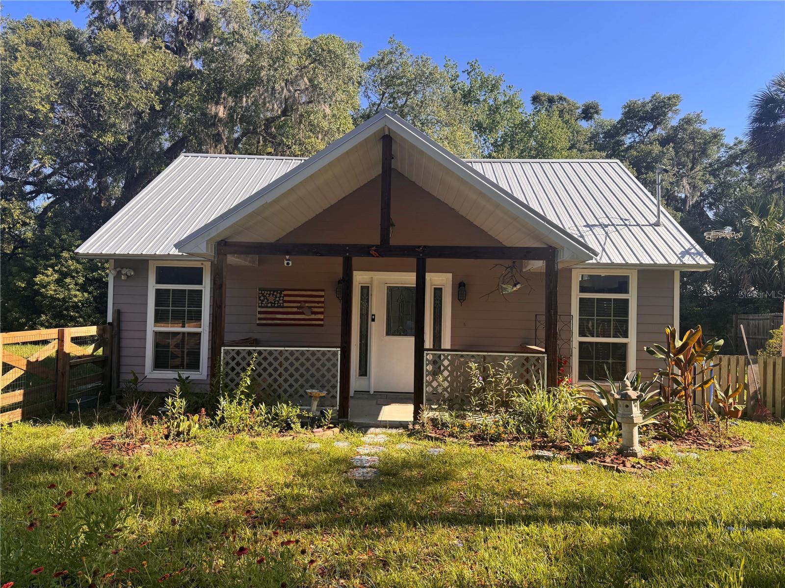 Charming country cottage in the heart of downtown Melrose. This artist inspired, custom-built home features an open floor plan with high ceilings, ceramic tile flooring and lots of natural light!  The kitchen has a gas range, SS Refrigerator, and farm sink. The primary bedroom has a half bath. Washer & dryer and included. The kitchen opens onto a 16x16 ft wood deck with hot tub and pergola and fenced back yard. There is a tool shed and a covered RV carport with concrete pad. Fully Finished 10x16 storage shed with 2 loft spaces and electric was used as artist studio. The corner lot has fruit trees, palms and a wildflower/pollinator garden. High speed cable internet access via Kenetic by Windstream.  LOW Clay Electric Cooperative rates and LOW Putnam County taxes. Plenty of room to add an addition, ADU, or detached dream home while you live onsite.  Rural ambiance, but located only blocks from Heritage Park.  Walk to Mossman Hall, Melrose Bay Art Gallery, Melrose Community Center, and renowned Blue Water bay restaurant. Only 20 miles to Gainesville or Palatka. Melrose offers wonderful Small-town vibes and is well-known for its rich history, and its vibrant music, arts & culture scene. Become a part of this amazing community!
