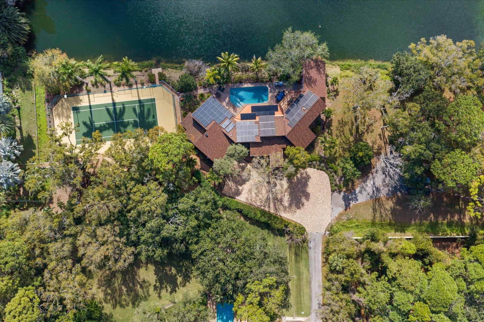 Nestled on a picturesque lake in the heart of Pinellas County, this exceptional home in desirable Kent Place offers the perfect blend of privacy, resilience, and refined Florida living. Thoughtfully designed and meticulously maintained, the residence showcases stunning lake views, a resort-style outdoor setting, and extensive upgrades throughout.

Inside, Brazilian cherry wood floors flow throughout the home, complemented by custom cabinetry in the family room, formal living room, and primary suite. The expansive eat-in kitchen features granite countertops and solid wood cabinetry, while enjoying beautiful lake views and opening seamlessly to the outdoor entertaining areas. A true highlight of the home is the custom, temperature-controlled wine cellar with seating—ideal for collectors and entertainers alike.

The spacious primary suite features vaulted two-story ceilings, a private office, custom built-ins, and a spa-inspired Bain jacuzzi style bath with rain-head shower surrounded by granite walls.The thoughtfully designed split bedroom floor plan provides excellent privacy, with one ensuite bedroom, a separate wing featuring two bedrooms with a Jack-and-Jill bath, and two additional upstairs bedrooms that also share a Jack-and-Jill bath. The upstairs bedrooms open to a shared balcony overlooking the pool and tranquil lake.

Outdoor living truly shines with a porcelain-tiled pool deck, sparkling swimming pool, and a top-of-the-line designer outdoor kitchen featuring a built-in grill and high-energy gas burners designed for wok cooking and other direct-heat preparation, all complemented by a private dock. The lake has been stocked twice with northern striped bass and, importantly, the property has experienced no flooding from the lake. Additional exterior amenities include a lighted tennis court with basketball hoop, creating a truly rare recreational offering.

This home is exceptionally well equipped for peace of mind and efficiency, boasting 100% solar power with battery storage, a solar water heater, two Tesla chargers, and hurricane-impact Miami-Dade rated windows and doors throughout. During recent storms, the home retained power thanks to the impressive solar power system. An oversized two-car garage completes the package.

A rare opportunity to own a lakefront property with unmatched upgrades, energy independence, and an unbeatable Clearwater location—just minutes from everything while feeling worlds away.