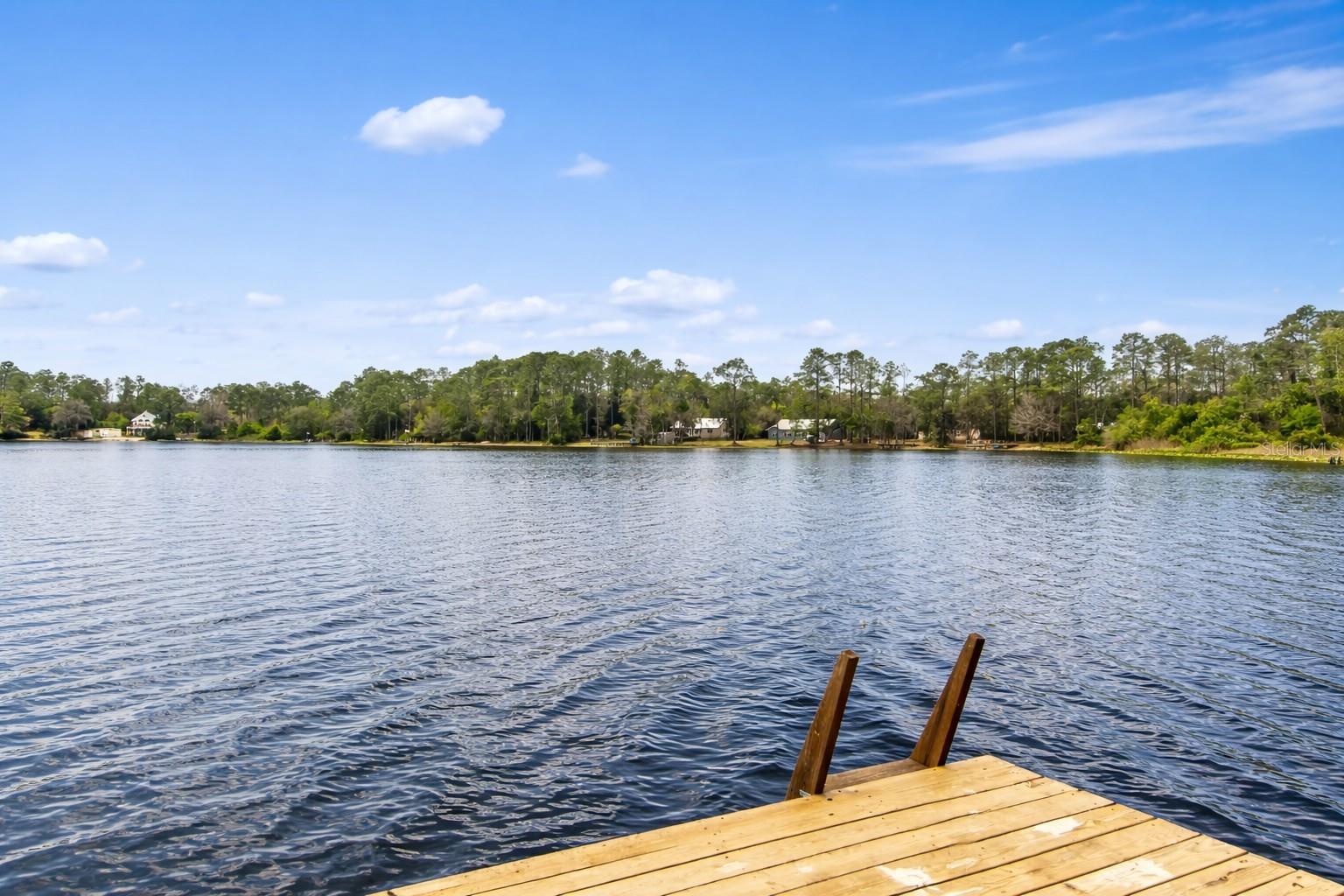 One or more photo(s) has been virtually staged. Welcome home to your architecturally distinct lakefront retreat on Riley Lake. Escape to your own peaceful, secluded setting where everyday living feels like a getaway. This custom 2BR/2.5BA home sits on ¾ of an acre of private, lush grounds with mature landscaping including orange, lime, Meyer lemon, and grapefruit trees, along with Japanese maple, azaleas, butterfly bushes, and a striking bottlebrush tree. Designed in two thoughtfully connected phases, the home is joined by a bright sunroom ideal as additional living space, reading lounge, or future hot tub area. Soaring ceilings and abundant natural light fill the great room, highlighted by a central cupola with clerestory windows, where a gas fireplace and custom built-ins anchor the open layout flowing seamlessly into the kitchen and dining area with stunning lake views. Numerous French doors lead to a screened porch and spacious composite deck, creating effortless indoor-outdoor living and entertaining. Both bedrooms are oversized, including a flexible guest room/office with a Murphy bed, while the primary suite offers beautiful lake views, a walk-in closet, built-ins, fireplace, and private outdoor shower. The remodeled kitchen features granite countertops, wood cabinetry, and excellent flow for gatherings. A new well pump, two tankless water heaters (approx. 2 years old), two HVAC systems, whole-home generator, and durable metal roof add to the home’s appeal. Outdoor amenities include a fully equipped summer kitchen (grill, fridge, sink), half bath, two oversized storage buildings, water treatment system, and fenced dog run. Enjoy ~120 feet of private waterfront with your own dock on spring-fed Riley Lake—one of two multi-purpose lakes (with neighboring Star Lake) ideal for swimming, boating, and fishing—with optional Star Lake access for just $50/year. Perfect as a full-time residence or weekend lake house retreat, this rare waterfront property offers privacy, flexibility, and the kind of serene Florida lakefront living that’s hard to find, all just minutes from Gainesville and Ocala.