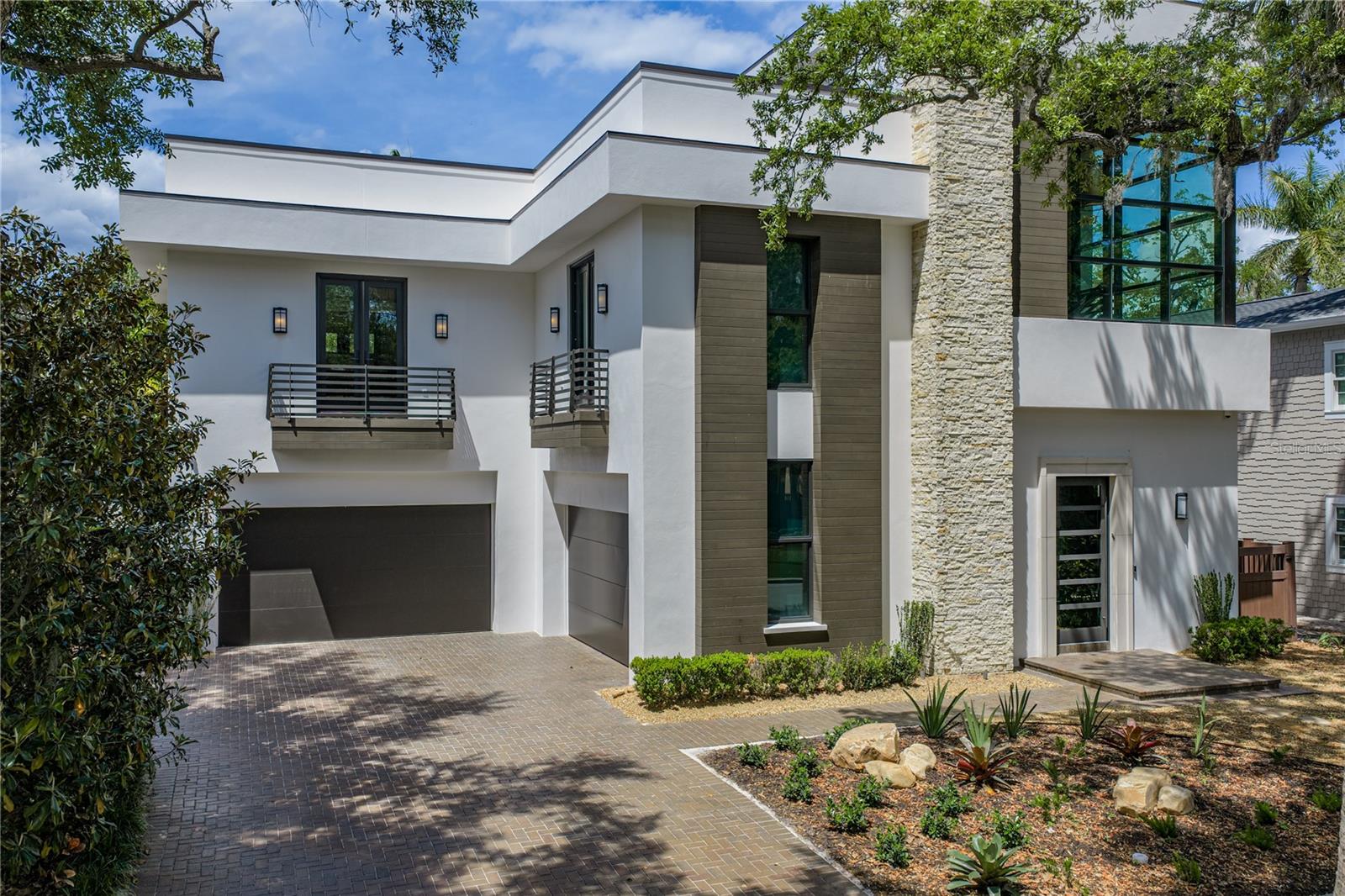 Set along a picturesque, oak-lined street in the highly coveted Villa Rosa Park, steps from the iconic Bayshore Boulevard sits an extraordinary, award-winning contemporary residence. A masterclass in architectural design, luxury, and effortless living. Custom built by Windstar Homes this home offers both striking curb appeal and a sense of serene privacy. The home makes an unforgettable impression. A dramatic 42-inch custom pivoting steel door opens to a breathtaking three-story foyer, where a soaring stacked stone feature wall, custom designer pendants, and a floating walnut staircase create a stunning architectural centerpiece. Every detail has been thoughtfully curated for both grand entertaining and refined everyday living. Spanning three spacious levels, the residence showcases all block construction, hurricane-rated windows and doors, a private elevator servicing all floors, and a suite of high-performance systems including a whole-house Generac generator,  tankless gas water heater, whole-house water filtration, integrated CATV wiring, and a Savant home automation system, and security. The main living level is designed to blur the line between indoors and out. Expansive EuroWall stacking glass doors open to a lush, manicured backyard retreat featuring a resort-style pool and spa with outdoor speakers, custom landscape lighting, and a gas fire pit—creating an intimate, private setting for both relaxed evenings and elevated entertaining. Inside, whitewashed wide-plank oak floors run throughout, enhancing the modern elegance. At the heart of the home, the chef’s kitchen is both functional and inspiring, featuring a full suite of Thermador appliances, custom Busby cabinetry, and leathered quartzite countertops. Adjacent, a show-stopping cocktail bar—complete with dual 84-inch wine towers and ice maker—creates the ultimate setting for entertaining at any level. For the automotive enthusiast, the property offers a rare and remarkable feature: two climate-controlled garages. Space for up to five vehicles, both garages are equipped with a slimline Mitsubishi split system. Designed with exceptional versatility in mind, the secondary garage transforms seamlessly into an extension of the home’s living space—fully equipped with a gas fireplace, television, and a retractable screen enclosure when opening  to the backyard, this unique space functions as a stylish indoor-outdoor lounge, perfect for entertaining, relaxing, or showcasing prized vehicles in a gallery-like setting. Upstairs, a one-of-a-kind private cinema elevates the experience of home living, featuring CinemaTech seating for eight with a 120-inch screen. The second level also hosts a serene, hotel-inspired primary suite along with an additional two bedrooms, all designed with comfort and sophistication in mind. Crowning the home is the spectacular third-floor sky deck—an entertainer’s dream and a true sanctuary in the sky. Designed for both vibrant gatherings and quiet moments, this expansive rooftop retreat features a covered bar, sound system, and ltelevisions, all set against the backdrop of breathtaking Florida sunsets. With flexible living options, including convertible bedroom configurations, this home adapts effortlessly to your lifestyle. It presents a rare opportunity to step into a turnkey luxury experience. Resort-style, low-maintenance living meets architectural excellence. This is more than a home—it is a statement, a sanctuary, and an experience unlike any other.