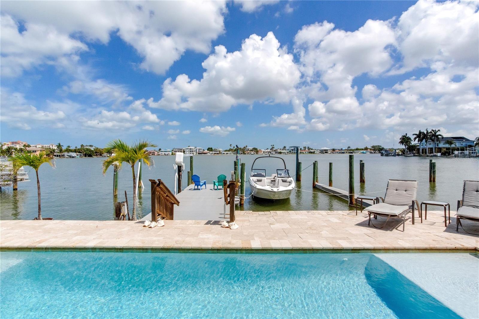 WELCOME TO YOUR WATERFRONT PARADISE IN NORTH REDINGTON BEACH WITH A LIFT AND WET SLIP!  This beautiful 3-bedroom, 2.5-bath coastal retreat offers the perfect blend of luxury, comfort, and effortless Florida living. Elevated construction, lush tropical landscaping, and striking curb appeal welcome you home as you step inside to soaring ceilings, abundant natural light, and breathtaking water views that immediately capture your attention.  Designed with both everyday living and entertaining in mind, the spacious open floor plan flows seamlessly from room to room. The inviting living spaces feature elegant finishes, custom details, and expansive windows that showcase the tranquil waterfront setting. The beautifully appointed kitchen offers generous cabinetry, ample counter space, breakfast bar seating, and opens directly into the main living and dining areas, creating the ideal atmosphere for gatherings with family and friends.  The newly renovated primary suite, conveniently located on the first floor, is a true private oasis. This luxurious retreat features spacious accommodations, beautiful flooring, and a stunning spa-inspired ensuite bathroom complete with modern finishes, dual vanities, soaking tub, and oversized walk-in shower. Upstairs, the additional guest bedrooms provide comfortable accommodations for family and visitors alike.  Step outside into your own tropical resort-style backyard where waterfront living truly comes to life. The expansive travertine pool deck surrounds the sparkling pool and jacuzzi, both equipped with a heater and chiller for year-round enjoyment. Relax in the sun, entertain under the stars, or simply take in the wide-open water views and coastal breezes. The dock offers quick access to the Intracoastal and Gulf waters, making this property ideal for boating enthusiasts.  Additional highlights include paid-off solar panels that greatly enhance the home’s energy efficiency, turf landscaping for low-maintenance living, a spacious laundry room, oversized 2-car garage, and multiple indoor and outdoor entertaining spaces. From the peaceful waterfront setting to the thoughtful upgrades throughout, this home embodies the very best of luxury coastal living in the heart of North Redington Beach.