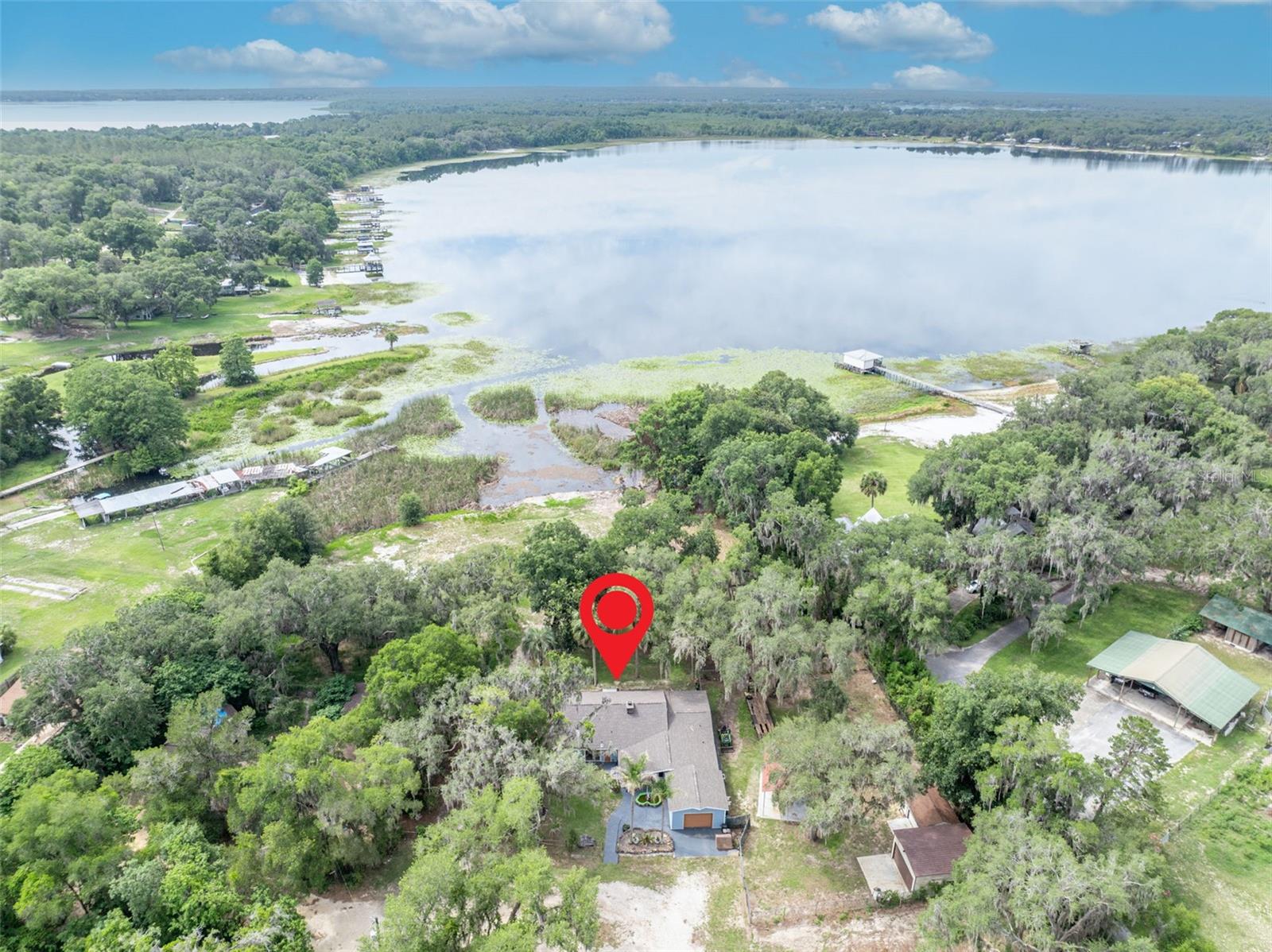 PRICE IMPROVEMENT! Don't miss this newly repositioned gem. You have been looking for a place where the day actually slows down. Where the only thing on the schedule is the sunset, and the only sound at the end of the day is the water. This is that place. That version of your life lives at the end of a quiet cul-de-sac on Little Lake Weir. Walk through the front door and the home opens up the way good homes do. A floor-to-ceiling stone fireplace anchors the great room, double-sided, the kind that has hosted a thousand quiet evenings and is ready for a thousand more. Above it, soaring tongue-and-groove wood ceilings and exposed beams stretch across the main living areas, warm and unmistakably Florida. The sightlines pull you forward, through the kitchen, through the dining space, all the way to the water glinting through the oaks beyond. Then you step into the Florida room and you understand why this house exists. Glass on three sides. That same wood plank ceiling overhead. The lake out front, the breeze moving through, the oaks dripping Spanish moss on every side. This is the room where coffee turns into conversation and conversation turns into afternoon. This is where you will be when someone asks where you have been lately. The kitchen keeps pace with the rest of the home, opening cleanly into the living and dining spaces with stone backsplash, generous wood cabinetry, and a flow built for the way real life happens that makes hosting feel effortless and weeknights feel easy. Four bedrooms and two bathrooms give everyone room to land. The seller has already done the hard part with $150k in premium updates, including Brand new roof. New exterior siding. A Culligan water treatment system-2024, new high efficiency AC-2024, new Well-2020. Fresh interior paint throughout. Wood look tile and new plush carpet-2024. And here is where the story gets better. Two parcels convey together. Behind the home, a 1 acre-deeded access boasts 230 feet of private beachfront with a secluded cove nestled next to a peninsula, complete with its own boat ramp and a nearby sandbar leading out to direct access on Little Lake Weir. Just down the street, Carney Island Recreation and Conservation Area waits with its public ramp into the main 5,600-acre Lake Weir. Quiet water out your back door. Big water when you want it. The kind of setup that does not exist anymore, except here. Outside, the property is built for the way Florida is meant to be lived. The attached garage takes care of the everyday with room for your car and ample storage with existing shelves. A detached two-bay garage and a separate one-bay garage are the true craftsman dream, featuring multiple 110V & 220V electrical hookups, including a generator back-feed breaker-ensuring you don't go without when hurricane season comes! The detached garage also features floor to ceiling shelving and work benches, and one of them even has air conditioning. A large covered concrete boat and RV pad with electricity means the toys come home with you. Mature live oaks shade the grounds, and the additional vacant parcel-bringing the total acreage to just under an acre at .83- handing you privacy, room to roam, and whatever you want to dream up next. This is lakeside Ocala the way it used to be. Big skies. Lily pads on the shoreline. Seaplanes on the water. Bass under the brush piles. Are you ready to start your next chapter?