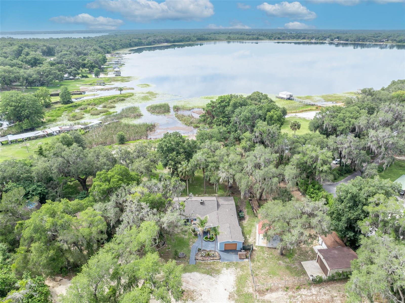 PRICE IMPROVEMENT! Your ultimate family Lake destination is now more affordable than ever! If you've been looking for a place where the day actually slows down. Where the only thing on the schedule is the sunset, and the only sound at the end of the day is the water. This is that place. That version of your life lives at the end of a quiet cul-de-sac on Little Lake Weir. Walk through the front door and the home opens up the way good homes do. A floor-to-ceiling stone fireplace anchors the great room, double-sided, the kind that has hosted a thousand quiet evenings and is ready for a thousand more. Above it, soaring tongue-and-groove wood ceilings and exposed beams stretch across the main living areas, warm and unmistakably Florida. The sightlines pull you forward, through the kitchen, through the dining space, all the way to the water glinting through the oaks beyond. Then you step into the Florida room and you understand why this house exists. Glass on three sides. That same wood plank ceiling overhead. The lake out front, the breeze moving through, the oaks dripping Spanish moss on every side. This is where you will be when someone asks where you have been lately. The kitchen keeps pace with the rest of the home, opening cleanly into the living and dining spaces with stone backsplash, generous wood cabinetry, and a flow built for the way real life happens that makes hosting feel effortless and weeknights feel easy. Four bedrooms and two bathrooms give everyone room to land. The seller has already done the hard part with $150k in premium updates, including Brand new roof. New exterior siding. A Culligan water treatment system-2024, new high efficiency AC-2024, new Well-2020. Fresh interior paint throughout. Wood look tile and new plush carpet-2024. And here is where the story gets better. Two parcels convey together. Leverage the bonus parcel to build rental income or expand into a truly multigenerational lakeside compound. Behind the home, a 1.21 acre-deeded access boasts 230 feet of private beachfront with a secluded cove nestled next to a peninsula, complete with its own boat ramp and a nearby sandbar leading out to direct access on Little Lake Weir. Just down the street, Carney Island Recreation and Conservation Area waits with its public ramp into the main 5,600-acre Lake Weir. Quiet water out your back door. Big water when you want it. The kind of setup that does not exist anymore, except here. Outside, the property is built for the way Florida is meant to be lived. The attached garage takes care of the everyday with room for your car and ample storage with existing shelves. A detached two-bay garage and a separate one-bay garage are the true craftsman dream, featuring multiple 110V & 220V electrical hookups, including a generator back-feed breaker-ensuring you don't go without when hurricane season comes! The detached garage also features floor to ceiling shelving and work benches, and one of them even has air conditioning. A large covered concrete boat and RV pad with electricity means the toys come home with you. Mature live oaks shade the grounds, and the additional vacant parcel-bringing the total acreage to just under an acre at .83- handing you privacy, room to roam, and whatever you want to dream up next. This is lakeside Ocala the way it used to be. Big skies. Lily pads on the shoreline. Seaplanes on the water. Bass under the brush piles. Are you ready to start your next chapter?