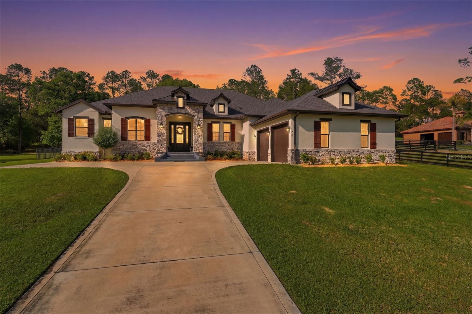 Luxury, space, and timeless design come together in this stunning custom residence located in the highly sought-after acreage community of Lakewood Ranches. Situated on 3.25 private acres, this exceptional 4-bedroom, 3.5-bath home offers the perfect blend of upscale living, thoughtful design, and peaceful surroundings, highlighted by striking copper roof accents that reflect the quality found throughout.
From the moment you enter, the home impresses with vaulted ceilings, crown molding, and an open, light-filled layout designed for both everyday living and effortless entertaining. Three expansive sliding glass doors create a seamless connection between the interior living spaces and the outdoor entertaining area, filling the home with natural light and beautiful views of the property. The gourmet kitchen serves as the heart of the home and is designed to impress, featuring granite countertops, high-end soft-close cabinetry, an oversized island, premium appliances, wine cooler, double oven range with designer hood, and a spacious butler’s pantry offering exceptional storage and prep space.
The expansive primary suite provides a private retreat with bay windows overlooking the property. The spa-inspired ensuite bath features dual vanities with a dedicated vanity area, a large walk-in shower, and multiple storage closets, while the oversized walk-in closet provides abundant organization space. Additional interior features include a library or flex room, recessed lighting, custom accent walls, spacious walk-in closets, waterproof luxury vinyl plank flooring, custom blinds, low-E windows, blown-in insulation, and a well-designed laundry room with sink and floor drain. Outdoor living is equally impressive. The large covered patio with ceiling fans creates the perfect setting for relaxing or entertaining while enjoying the expansive acreage and peaceful surroundings. The property also includes an oversized two-car garage plus an additional side-entry garage, ideal for storage, recreational equipment, or a golf cart. An XL well system efficiently services the home and offers capacity for future additions such as a detached structure or additional amenities. Located in East Lake County, Lakewood Ranches offers the appeal of spacious acreage living while remaining convenient to nearby shopping, dining, and major roadways connecting to the greater Orlando area. The surrounding area is also known for its abundance of equestrian amenities and outdoor recreation opportunities, with nearby riding trails, training facilities, and horse-friendly parks providing opportunities for trail riding and equestrian activities throughout the region. Combined with the area’s scenic landscapes and open spaces, this location offers a unique opportunity to enjoy both luxury living and a lifestyle connected to the outdoors. A rare opportunity to own a beautifully designed luxury home on acreage in one of East Lake County’s most desirable communities.