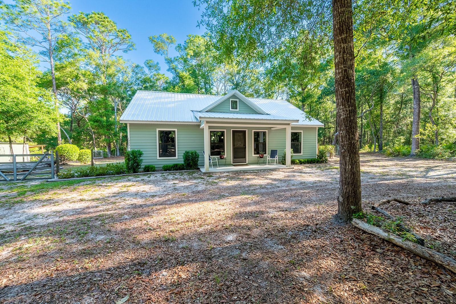 Tucked away on 4.5 beautiful acres in Chiefland, this charming 2 bedroom, 2 bathroom home offers the perfect blend of comfort, privacy, and outdoor living. Step inside to an inviting open-concept layout featuring high ceilings that create a bright and spacious feel throughout the home. The thoughtfully designed interior also includes a large pantry and oversized laundry room, providing plenty of storage and convenience for everyday living. Outside, this property is set up to fully enjoy the Florida lifestyle. Relax and entertain in the outdoor cooking area, gather around the fire pit on cool evenings, or explore the peaceful nature trails that wind throughout the property. The back portion of the property is fenced, offering added functionality while still maintaining the natural beauty of the land. Additional improvements include a 10x20 storage building with an attached carport and an 8x10 workshop with its own attached carport, offering ample space for hobbies, equipment, or recreational vehicles. Located in the heart of Chiefland, you’ll enjoy the quiet beauty of North Central Florida while still being close to shopping, dining, schools, and everyday conveniences. The area is known for its nearby natural springs, boating, fishing, and outdoor recreation opportunities along the Suwannee River and the Nature Coast State Trail. Whether you’re looking for a peaceful homestead, weekend retreat, or full-time country living, this property offers the space and setting to make it your own.