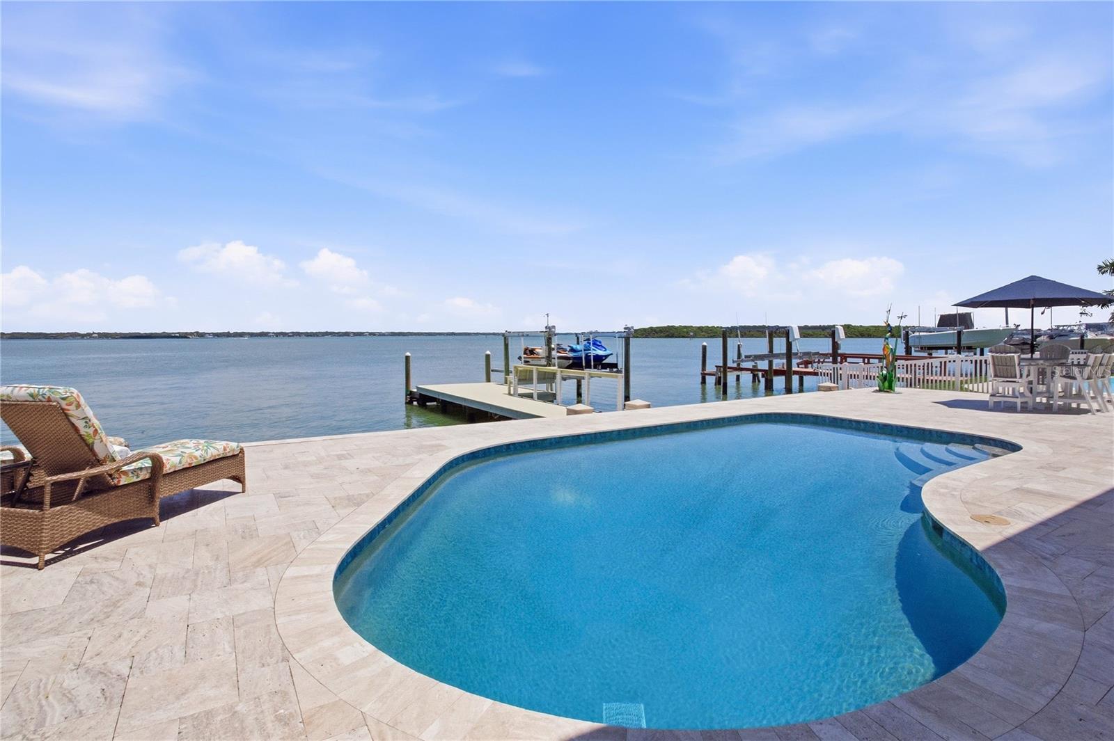 WELCOME TO 547 JOHNS PASS AVENUE A RARE OPEN WATER ESTATE FEATURING TWO PRIMARY SUITES, BREATHTAKING PANORAMIC VIEWS, AND THE ULTIMATE FLORIDA WATERFRONT LIFESTYLE. Perfectly positioned on an expansive stretch of wide-open water, this extraordinary coastal retreat was thoughtfully designed to capture spectacular views from nearly every room while blending luxurious indoor-outdoor living seamlessly throughout the home. From the moment you arrive, the circular paver driveway, lush tropical landscaping, and striking coastal architecture create an unforgettable first impression. Step through the grand entryway into a light-filled open-concept floorplan where soaring ceilings, oversized windows, and endless water views immediately steal the show.  Designed for both elegant everyday living and effortless entertaining, the expansive living and dining spaces flow beautifully into the gourmet chef’s kitchen featuring custom cabinetry, stunning quartz countertops, oversized center island, premium Bosch appliances, designer backsplash, abundant storage, and an impressive wet bar with beverage refrigeration. Every detail has been thoughtfully curated to complement the home’s coastal aesthetic.  One of the home’s most exceptional features is the presence of TWO PRIVATE PRIMARY SUITES offering incredible flexibility for multigenerational living, guests, or creating the ultimate private retreat experience. The first-floor primary suite features a spacious walk-in closet, ensuite bath, and convenient access to the main living areas, while two additional well-appointed guest bedrooms share a beautifully updated guest bathroom. A spacious laundry room is also conveniently located on the first floor.  The entire second floor is dedicated to the luxurious grand primary retreat a true sanctuary of peace and tranquility. Wake up each morning to breathtaking sunrises and sweeping open water views through oversized windows designed to showcase the incredible scenery. This remarkable suite offers a spa-inspired ensuite bath, expansive walk-in closet space, private waterfront balcony, and a loft/office area ideal for working remotely while overlooking one of the most spectacular waterfront settings on the Gulf Coast. The upstairs retreat feels like a private penthouse oasis suspended above the water.  Step outside into your private waterfront paradise where resort-style living awaits. The expansive travertine pool deck surrounds the sparkling saltwater pool and creates multiple areas for lounging, dining, and entertaining while overlooking the stunning open water backdrop. The covered balcony provides the perfect setting for morning coffee, evening cocktails, and unforgettable sunsets. Boating enthusiasts will appreciate the private dock and lift with direct access to open water.  Every detail of this exceptional residence has been carefully designed to embrace the beauty of waterfront living while offering luxury, comfort, and functionality. With its rare dual primary suite layout, breathtaking views, and seamless indoor-outdoor design, this is more than just a home it is a private coastal sanctuary designed to experience the very best of luxury waterfront living.