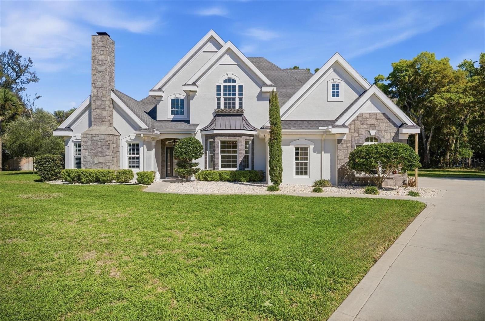 A storybook home tucked behind private gates on a coveted cul-de-sac, offering a rare sense of elegance and timeless charm. Desired Halifax Plantation Phase 1, on fully fenced property. Better than new, this beautifully appointed 4-bedroom, 3.5-bath residence offers 3,324 square feet of refined living space, thoughtfully designed to blend timeless elegance with elevated Florida living. Set on an expansive and private homesite in Ormond Beach, the home showcases sophisticated interiors with soaring ceilings, rich wood flooring, custom millwork, and a seamless, open-concept layout ideal for both everyday living and upscale entertaining. The main living areas are enhanced by architectural detailing and flow effortlessly to the outdoor living space, while the chef’s kitchen features granite countertops, custom cabinetry, stainless steel appliances, and a sunlit breakfast area overlooking the grounds. The primary suite serves as a serene retreat with direct access to the lanai and a spa-inspired bath complete with dual vanities, a walk-in shower, and a generously sized custom closet. Additional bedrooms and versatile living spaces offer comfort and flexibility for guests, a private office, or secondary lounge areas. Outdoors, a resort-style setting awaits with a sparkling pool and sun shelf, expansive patio space, a covered lanai, and a fully equipped outdoor kitchen designed for effortless entertaining, all framed by lush, mature landscaping and a large fenced lawn. A stately exterior with stone accents, manicured grounds, and an expansive driveway further enhances the home’s presence, creating a polished and private estate feel. This exceptional property delivers a sophisticated yet relaxed lifestyle in one of Ormond Beach’s most desirable settings. To further elevate the Halifax lifestyle, residents enjoy access to community amenities through the HOA, including swimming, tennis, fitness, the clubhouse, and fine dining, while golf remains available separately at Halifax Plantation’s public course. With no CDD fees and a peaceful golf-course setting, this community offers a relaxed and enjoyable Florida lifestyle.