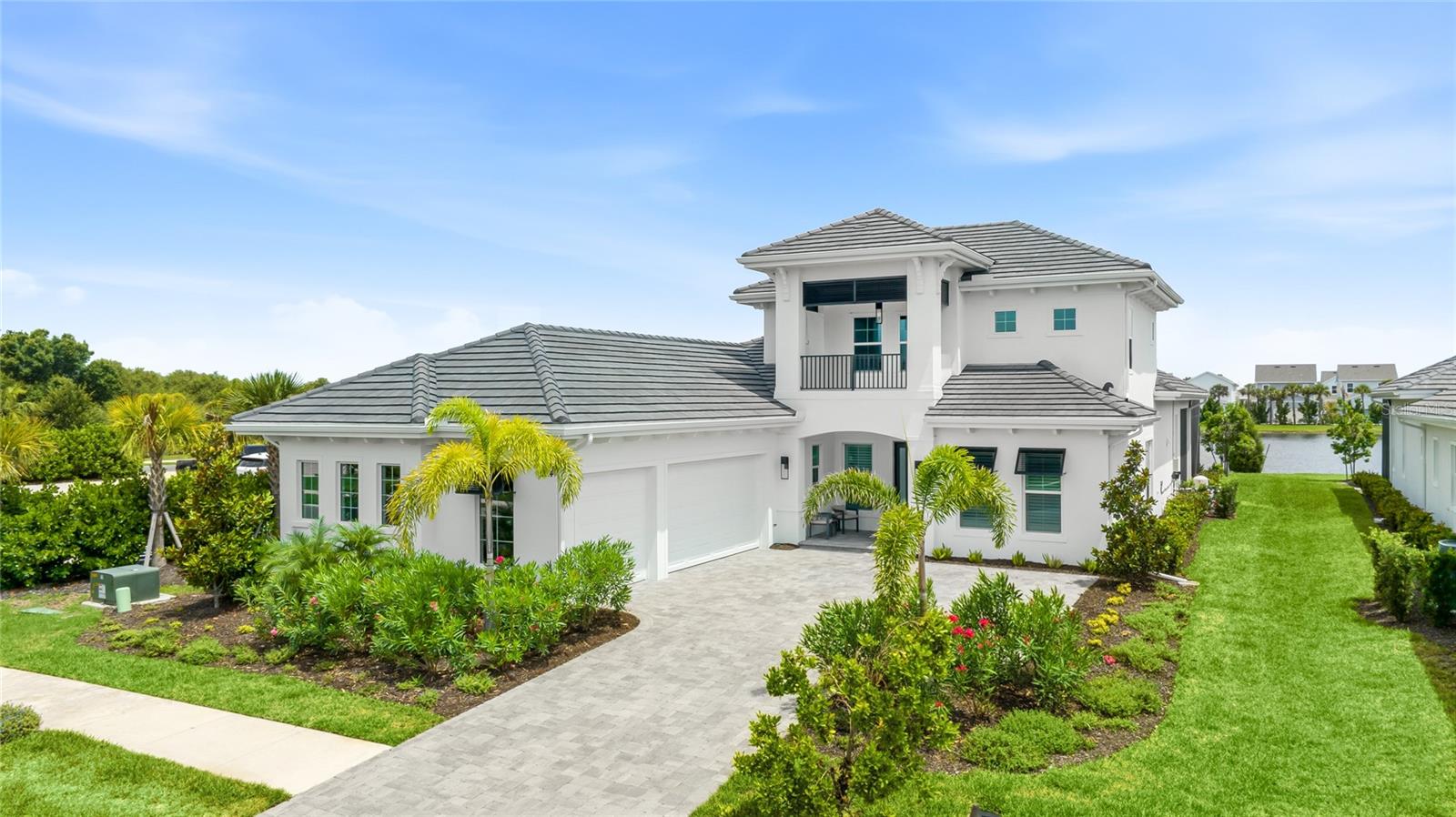 Welcome to Wild Blue at Waterside, where this 2024-built residence rests on a premier lakefront homesite in Lakewood Ranch's top resort community. Offering five bedrooms and four and a half baths across an expansive single-story footprint with a private upstairs retreat, it presents a rare opportunity to own a home already finished to an exacting standard, available now without the long wait and decisions of building from the ground up. The coastal-contemporary elevation sets the tone, with a crisp white facade, charcoal tile roof, a two-story tower balcony, and lush tropical landscaping framing the paver drive and three-car garage. Inside, natural light pours across wide-plank tile floors beneath soaring ceilings dressed with white oak faux beams, custom crown molding, and statement designer lighting throughout. The great room is the heart of the home, anchored by a shiplap feature wall with built-in display niches and crowned by a dramatic two-tier chandelier. A wall of pocketing glass sliders dissolves the line between indoors and out, carrying your eye across the pool to the water beyond. The kitchen is built for gathering, with a large island topped in marbled Cambria quartz, white shaker cabinetry, a custom range hood, a designer subway backsplash, and professional stainless appliances that include a gas cooktop, double wall oven, and built-in refrigerator. Nearby, a formal dining room dressed in crown molding and plantation shutters and a dedicated study with custom built-ins and a sliding barn door bring everyday function together with polish. The owner's retreat is a private sanctuary finished with a tray ceiling, a crystal chandelier, French door access to the lanai, and two custom walk-in closets. Its spa-inspired bath showcases dual vanities, a freestanding soaking tub, and an oversized glass shower with two-tone mosaic detail. Three additional bedrooms and well-appointed baths anchor the main level, while a generous upstairs loft with its own bedroom and full bath makes an ideal guest or bonus suite. Outdoor living is where this home truly shines. Beneath a panoramic screen enclosure, the custom pool and raised spillover spa glow amid twin water bowls, joined by a sun shelf, an expansive paver deck, and covered lounge and dining areas that all overlook the lake and its fountain. Designed for comfort and longevity, the home adds a whole-house water treatment system, a tankless water heater, and a fully outfitted three-car garage. Residents of Wild Blue enjoy a 25,000-square-foot clubhouse with resort and lap pools, indoor and outdoor dining, a fitness studio, golf simulator, private theater, and putting course. Just moments from Waterside Place, the shops and restaurants of UTC, and the Gulf beaches that define the Sarasota coast, this is Florida living at its most refined. Come experience it for yourself. **THIS PROPERTY QUALIFIES FOR A 1% LENDER INCENTIVE IF USING PREFERRED LENDER. INQUIRE FOR MORE DETAILS.**