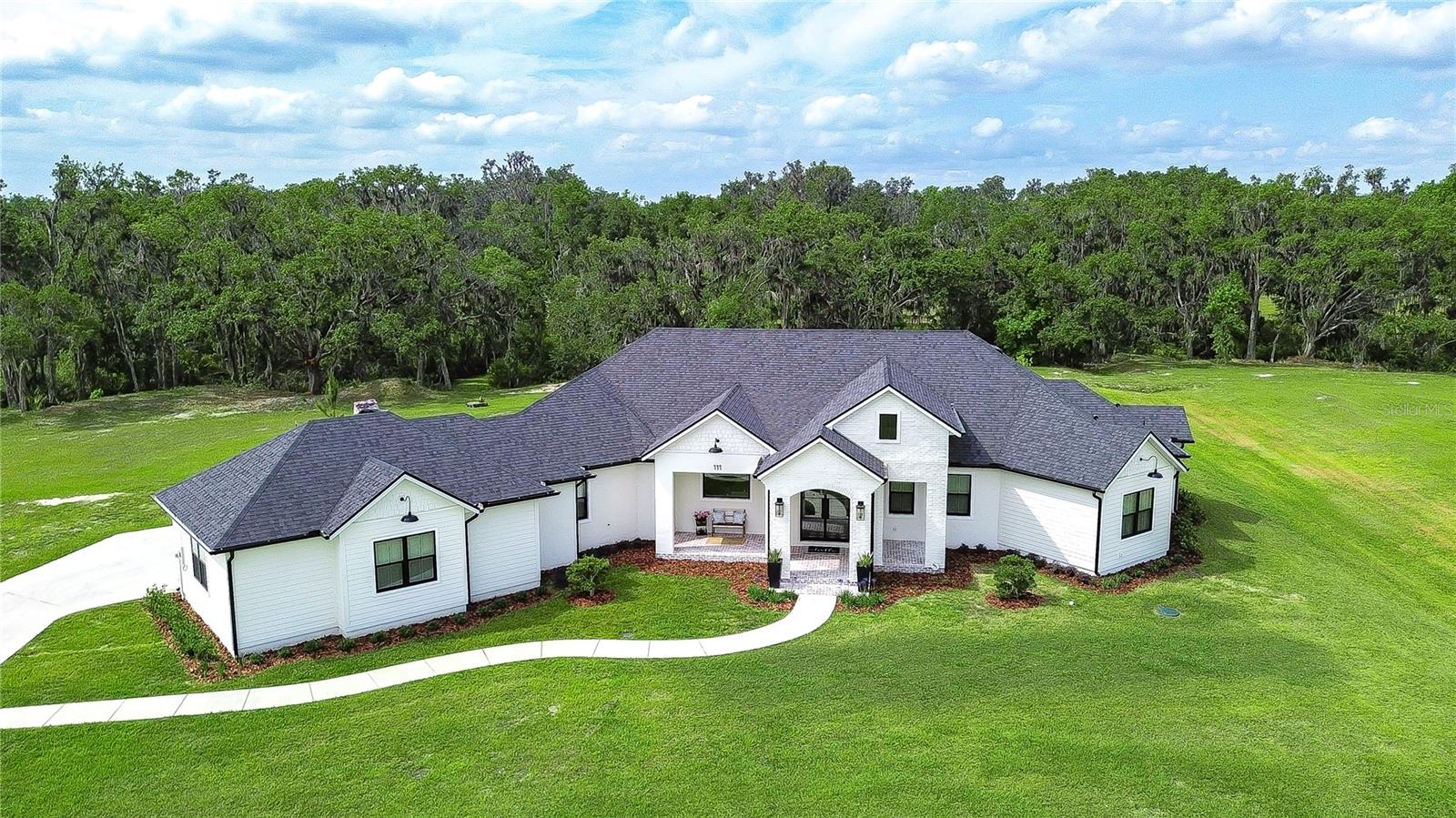 Welcome to the lifestyle you've been waiting for. Set on 5.11 stunning acres, this custom-built Southern Tradition estate is a rare blend of refined elegance, modern luxury, and peaceful, nature-filled surroundings. Whether you crave open space, love to entertain, or simply enjoy the outdoors, this one-of-a-kind property is ready to impress. From the moment you arrive, the white brick front porch and elegant glass French doors welcome you into a home filled with warmth and style. Inside, you'll find 8-foot doorways, soaring ceilings, and rich wood beam accents, all grounded by beautiful wood-look tile flooring that flows throughout the main living areas, including the office and primary suite—offering durability and timeless charm. The kitchen is a true showstopper—straight from the pages of a design magazine. Anchored by a massive center island with quartz countertops, it features top-of-the-line stainless appliances, including a Thermador gas cooktop with electric oven, built-in appliances, custom lighting, and a butler’s pantry that makes entertaining effortless. The great room is equally inviting, with a bold accent wall and pocket sliding doors that open to a sprawling brick-paver lanai—designed for your dream outdoor kitchen and pool. A spacious office sits at the front of the home and features a hidden Murphy door leading directly into the luxurious primary suite—adding both convenience and a touch of intrigue. The suite itself is a private oasis, complete with dual walk-in closets and an ensuite bath that stuns with marble floors, a soaking tub, and a huge walk-in shower with multiple shower heads, including a rainfall feature. The split floor plan offers ultimate privacy, with two additional bedrooms tucked away on the opposite side—one with its own private ensuite and walk-in closet, and the other adjacent to a full bath—ideal for guests or multigenerational living. Additional highlights include a bright dining room overlooking the backyard, a HUGE custom laundry room that combines beauty and functionality, and generous storage throughout the home. Step outside and you’re surrounded by natural beauty—whether you’re enjoying a quiet morning on the front porch, riding your ATVs across your private acreage, or heading out on a walk to the nearby Alafia River. With over 5 acres to explore, the opportunities are endless. And when you’re ready to venture out, you’re just a short drive from it all—close to major highways, Disney, and Florida’s world-famous beaches. Zoned for top-rated schools and just minutes from everyday conveniences, this home delivers luxury living with room to roam—all without sacrificing location.