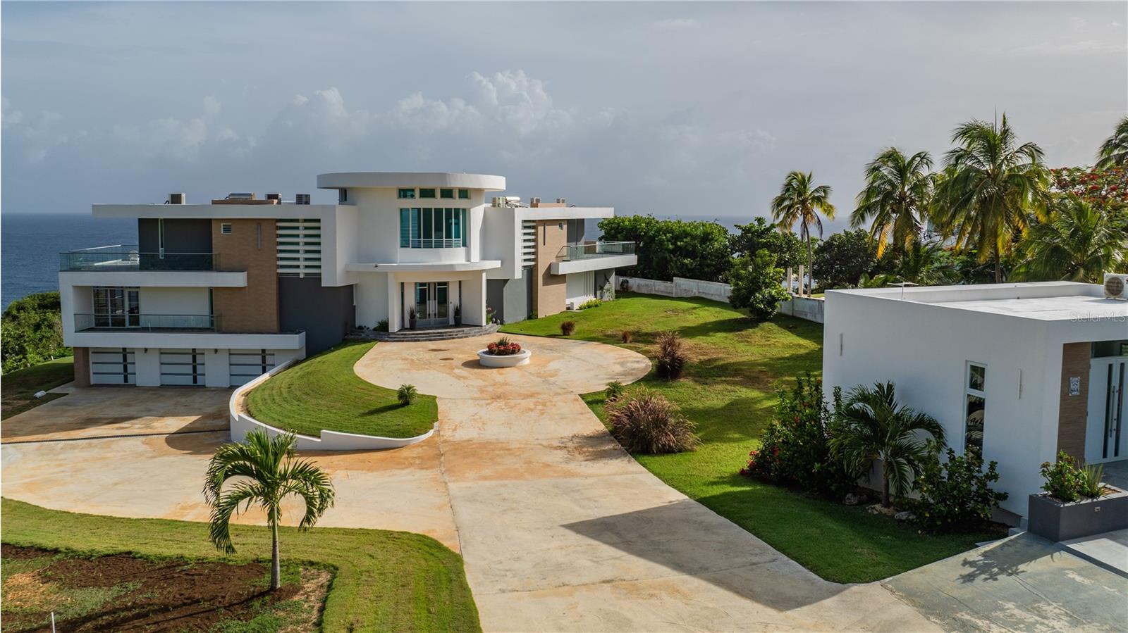 Perched 170 feet above the Atlantic, this modern oceanfront estate in Quebradillas Puerto Rico sits on 1.08 acres of private cliffside land in the Terranova area. Completed in 2024, the property includes a 6,465 sqft main residence and a 1,250 sqft guest house, offering panoramic ocean views from every room across both homes.

The architecture features clean modern lines, expansive glass, and a central spherical design with east and west wings, maximizing views in every direction. The interiors follow a white, gray, and ocean inspired palette with warm tan accents, creating a bright, contemporary coastal feel.

Main residence highlights:

• 3 bedrooms, each with private en suite bathroom
• 4.5 bathrooms total
• 12 ft ceilings throughout main living areas
• open kitchen with island and walk in pantry
• living room, office, and dining areas facing the ocean
• screened Florida room used as a dining space
• wraparound balconies with glass railings accessible from every bedroom and living area

The third floor game room serves as a dramatic entertainment space with:

• 20 ft ceilings
• wet bar
• panoramic Atlantic views

The lower level includes:

• 3 car enclosed garage with electric doors
• full laundry room
• full bathroom with backyard access
• storage space

The guest house built in 2023 includes:

• 2 bedrooms and 2 bathrooms
• kitchen, living, and dining areas with ocean views
• independent electric and water meters
• separate septic system

The fully enclosed 1.08 acre property features a 6 ft concrete privacy wall with electric vehicle gate and pedestrian entry. Parking includes the garage, guest house space, and room for 10+ additional vehicles along the driveway and circular motor court.

Outdoor highlights:

• dramatic cliff front Atlantic views
• seasonal humpback whale watching from the property (February through April)
• expansive backyard with ample space for an infinity pool overlooking the ocean

Nearby location anchors include:

• steps from Restaurante El Historico Puente Blanco
• hiking distance to Playa El Barco
• 6 minutes to Tunel de Guajataca
• under 1 hour to Rincon beaches and surfing
• approximately 30 km to Aguadilla International Airport

No HOA or community restrictions.

A rare opportunity to own a modern oceanfront estate in Quebradillas Puerto Rico designed for privacy, panoramic views, and multi residence living.